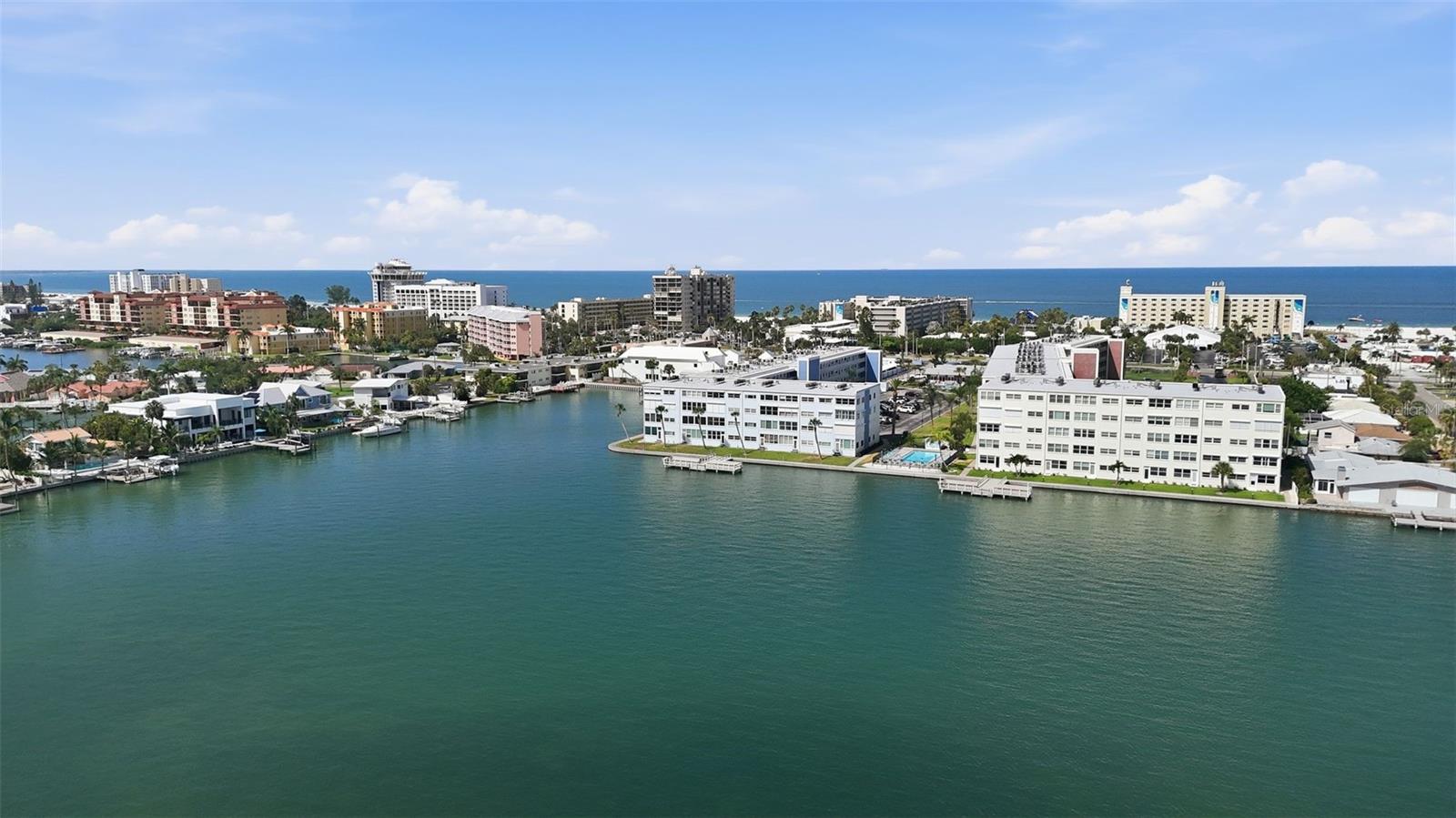 Step through the front door and your eyes go straight to open water — this beautifully renovated and fully furnished 2-bedroom, 2-bath condo at Regency West puts you steps from the sand and squarely on the water. The kitchen is the showstopper: an 11-foot island anchors a custom cabinetry package with a walk-in pantry, spice drawers, and soft-close doors, finished off with high-end Samsung appliances including a double-oven induction range and a beverage-center refrigerator. Both bathrooms have been fully updated tile walk-in showers, and spacious walk-in closets add everyday livability to the open, light-filled floor plan. From the sunroom with custom built in bar, watch the sun rise or the colors change in the sunset sky over the Bay. 
Tucked back from Gulf Blvd for a quiet, private feel, you're still just minutes on foot from the beach and everything St Pete Beach has to offer. Regency West's resort-style amenities include two heated pools, two clubhouses, a fitness center, shuffleboard courts, a common dock with fish-cleaning station, bike/kayak storage, common laundry on each floor and deeded parking right out front. Watch boats cruise the Intracoastal from your own living room — this is easy, elevated coastal living at a price point that's hard to find on the beach.