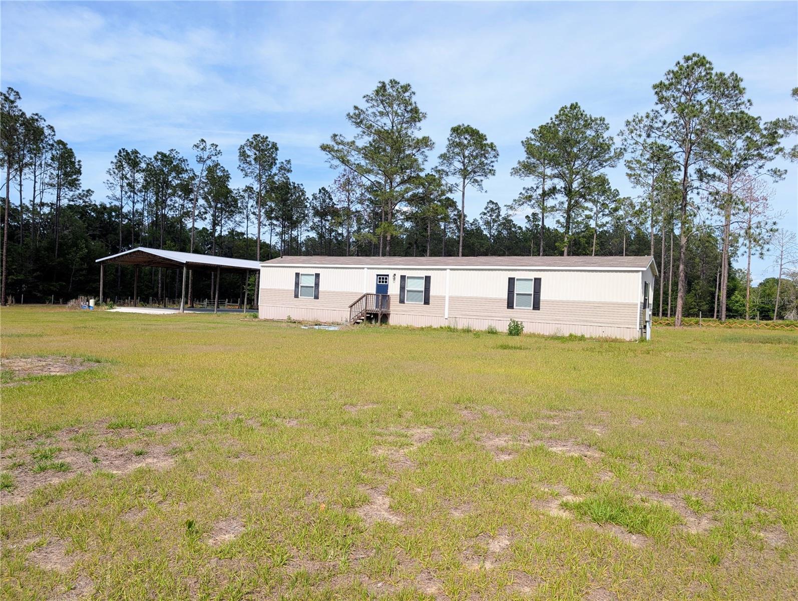 It's hard to beat the location of this attractive fenced and gated 5 acres near High Springs. The drive to it from the town (3.5 mi) is one of the most scenic in the area, a paved live oak-lined shaded avenue. The manufactured home was built in 2022 and has three bedrooms (split plan), two full baths, a laundry/utility area, and an open entry area with the kitchen and living room combined. Of considerable value is the 40' x 60' huge pole barn on a thick concrete pad. The parcel is split into a front and a back section of about the same acreage, defined by a central dividing fence behine the home and pole barn. The parcel is perimeter wire fenced and has black board fencing along the street with a recessed electric entry gate. From this home, one can take a variety of routes for access to Newberry, Alachua, and Gainesville, while remaining in the countryside avoiding more congested highways. The distance to I-75 exit #399 (High Spgs/Alachua) is 6.5 miles from this home. At that exit are Publix, Santa Fe High School, and a variety of restaurants and service businesses. There is no HOA. It's zoned A-agriculture.