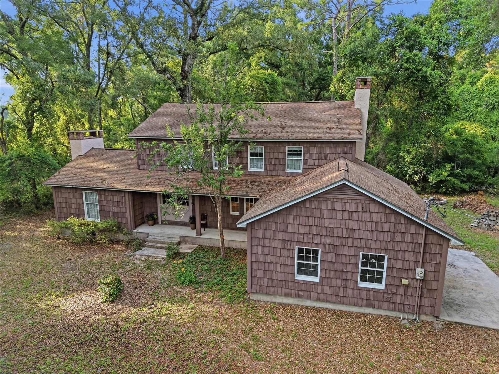 Fall in love with the warmth, craftsmanship, and unmistakable character of this one-of-a-kind owner-built estate nestled on 5 beautiful acres. Surrounded by mature trees and large stretches of neighboring farmland, the property captures both an Old Florida, laid back feel with a level of care and detail that’s hard to find today… this is the kind of home where “they don’t make them like this anymore” truly rings true. This Charming & Rustic Custom Built 2-Story Home offers Oak Hardwood Floors and Baseboards throughout- 3 bedrooms, 3 full bathrooms, 3 fireplaces, a 2-car attached garage, basement, a central vacuum system, large deck and an impressive detached garage/workshop ideal for hobbyists, collectors, craftsmen, or anyone needing substantial workspace and storage. The home is wrapped in cedar wood shakes and accented by Andersen double-hung windows and doors let in natural light while overlooking the native and lush surroundings. Feel welcomed as you step through a double-door entry into a natural slate tiled foyer, rich living room, and striking staircase that is a tribute to the craftsmanship carried throughout the home. The living room is the heart of the home- featuring tongue-and-groove wood ceilings, knotty pine wood walls all anchored by a classic wood burning brick fireplace that evokes a cozy lodge-inspired feel. The first floor features a full bathroom with antique inspired tile, a formal dining area, spacious kitchen with eat-in dining nook, and a separate living room with its own wood-burning fireplace. The country kitchen pairs artisan-style wood cabinetry with glass front displays, organic textures and everyday practicality. Head upstairs to a wood-enveloped loft overlooking the living space below that is home to two guest bedrooms, abundant storage, a full bathroom, and the Primary Suite. The Primary features its own wood-burning fireplace with stone surround, cedar-draped custom walk-in closet, walk-in shower, and bidet. One of the property’s most unique features is the basement — a rare find. This expansive lower level offers endless possibilities…finish it off as a game room, man cave, additional bedrooms, bunk space, guest quarters, multi-generational living, workshop space, or even potential rental accommodations. Conveniently located near Manatee Springs State Park, Chiefland Golf & Country Club, the Suwannee River, and Florida’s beloved Nature Coast recreation while still within reach of Gainesville conveniences. For those seeking a connection to nature, room to roam, and a legacy property where generations can gather, grow, and create lasting memories, this is a rare opportunity to own something truly unforgettable and truly special!