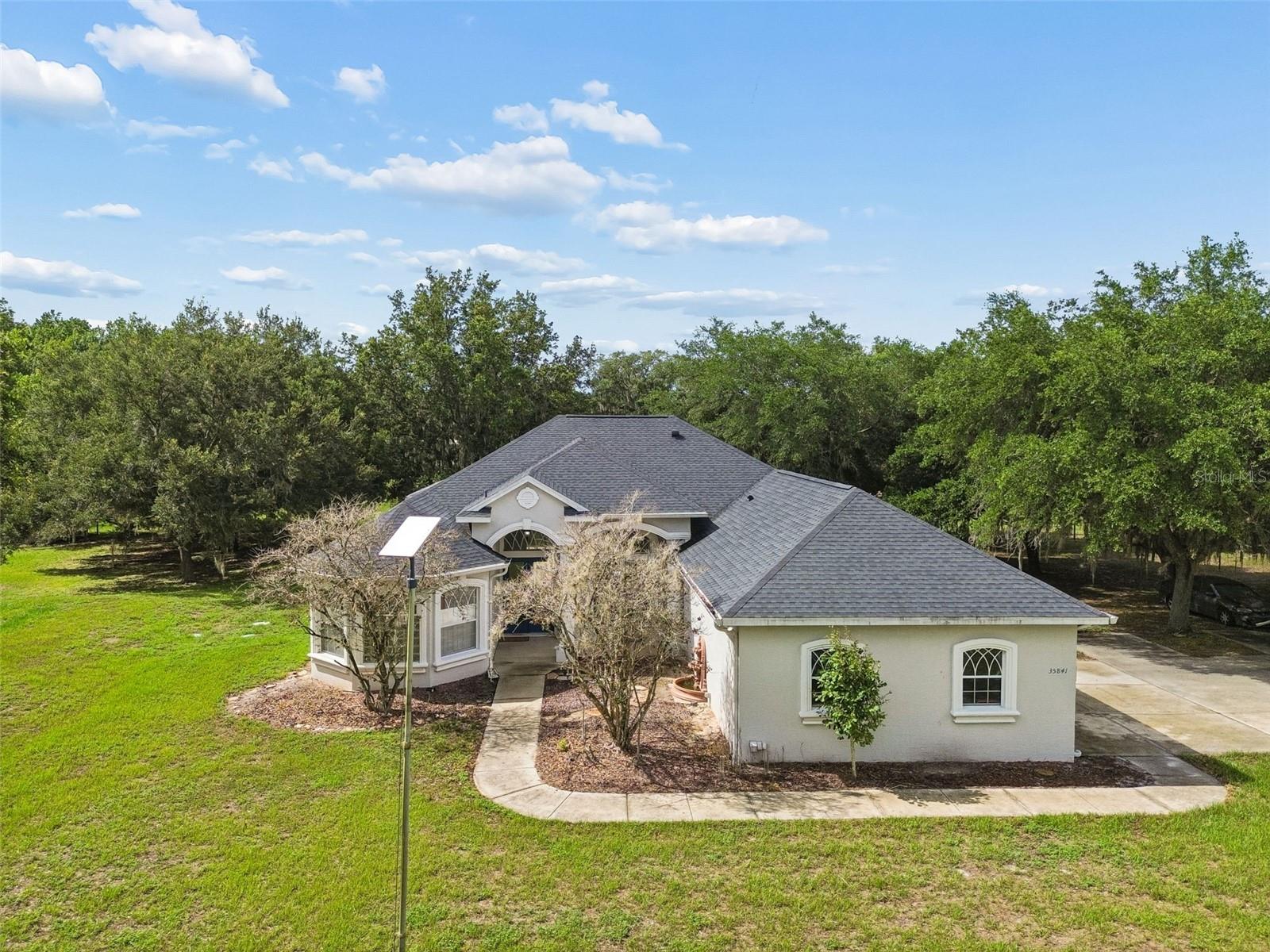 Virtually Staged. Country Living at Its Finest on 5 Acres! Welcome to this rare equestrian-friendly estate in the desirable Arrowwood Place community of Zephyrhills, where peaceful country living meets the convenience of nearby shopping, dining, and modern amenities. Nestled on a sprawling 5-acre homesite, this beautifully maintained 4-bedroom, 3-bathroom pool home with a 3-car garage offers the perfect blend of space, comfort, and privacy. Step through the grand foyer into a light-filled formal living and dining room featuring soaring ceilings, abundant natural light, luxury vinyl plank flooring, and crown molding throughout. The expansive split floor plan offers both functionality and privacy for family and guests. The oversized owner's suite is privately situated at the front of the home and serves as a true retreat, complete with elegant tray ceilings, two walk-in closets, and a spa-inspired ensuite featuring dual vanities, a relaxing Jacuzzi tub, and a separate shower. At the heart of the home, the spacious kitchen opens seamlessly to the inviting family room, creating the perfect gathering space for everyday living and entertaining. The family room showcases soaring ceilings, custom built-in cabinetry, and large windows that flood the space with natural light. Two generously sized bedrooms and a full bath are located just off the kitchen, while a fourth bedroom and full bath at the rear of the home provide an ideal private space for guests or multi-generational living. Step outside to your own private oasis featuring a screened lanai and sparkling pool, where you can relax, entertain, and enjoy peaceful views of your expansive property. Recent updates provide peace of mind and include a new roof (2022), new HVAC system (2024), fresh interior and exterior paint (2022), updated appliances, new water softener, and pool pump. Whether you're looking for room to spread out, space for horses, or simply a peaceful retreat surrounded by nature, this exceptional property delivers it all. Conveniently located near parks, nature trails, recreational facilities, and everyday conveniences, you'll enjoy the best of both worlds—tranquil country living with easy access to everything you need. Don't miss this incredible opportunity—schedule your private showing today! **ASSUMABLE VA MORTGAGE AT 4.625%**