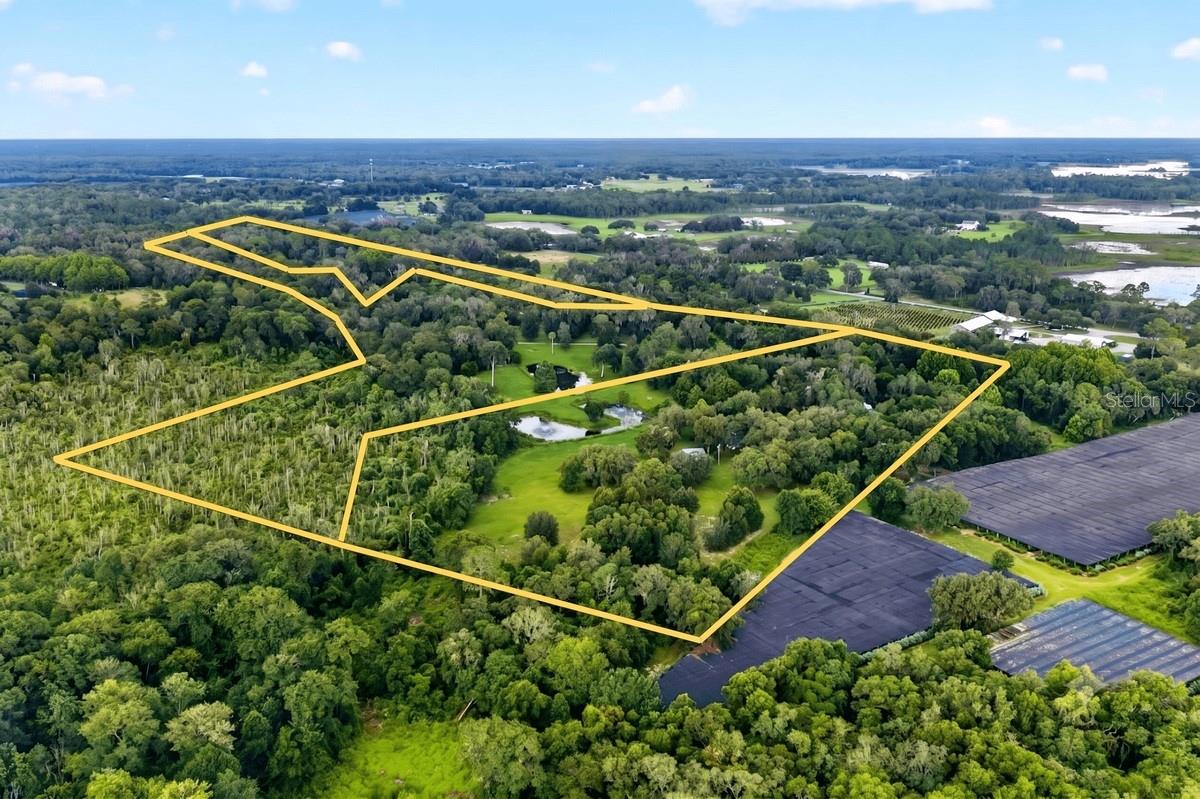 Tucked away on a quiet stretch of Lake Hires Road in DeLeon Springs, this two-story residence offers over 2,300 square feet of living space surrounded by more than 42 acres of Old Florida beauty, with a mix of wooded areas, cleared central pasture, and multiple ponds that create a truly private, scenic setting. A long drive leads past an elongated pond near the roadway and continues through the property toward the home, where an inviting covered front porch welcomes you, and an elevated wrap-around wood deck at the rear frames sweeping views of the pastures, scattered oaks, and the ponds closer to the homesite. The residence is thoughtfully designed for comfortable country living and multi-functional use. An attached oversized two-car pull-through carport offers easy in-and-out parking for vehicles, trailers, or equipment and connects directly to an unfinished 168-sq ft storage room, ideal for tools, feed, or workshop space. Inside, the first floor features a kitchen and a half bath combined with laundry, and a large wood-paneled living room anchored by a substantial brick two-sided fireplace. Off the kitchen, a finished, 160-sqft enclosed porch with wrap-around windows extends the living area and offers a comfortable all-season spot to enjoy the surrounding land, ponds, and wildlife views without stepping outside. The second floor offers a cozy loft with 2 bedrooms and 2 full baths. The primary bedroom is generously sized and includes two walk-in closets, along with an en-suite bath. A door from the primary suite opens directly onto the roof deck above the enclosed first-floor porch, creating a private outdoor retreat. Outside, a storage barn and a newly built 1,200-sqft storage shed offer substantial room for equipment, vehicles, or hobby use, all positioned to take advantage of the central cleared acreage that is highly usable, approximately 33.22 acres of the 42.32-acre tract. For equestrian or livestock use, the property is particularly compelling. A 2024-built, 1,360 sqft equestrian pole barn features a dirt-floor breezeway and 4 horse stalls, with an unfinished tack room that already has an elevated wood subfloor ready to be finished to your specifications. Complementing the equestrian infrastructure, a 2024 RV carport stands 14 ft high with durable metal construction in like-new condition. The land itself is a standout feature, combining privacy, usability, and natural character. The majority of the site is wooded, creating a buffer from neighboring properties and the road, while the central portions are cleared into pasture for riding, grazing, or future additional structures. Multiple ponds, including the elongated pond along the driveway and the ovular and u-shaped ponds near the home enhance the tranquil, retreat-like feel of the property. This rare combination of a home with extensive storage and like-new equestrian and RV facilities on over 42 acres makes this DeLeon Springs estate an exceptional opportunity for buyers seeking a private rural lifestyle, equestrian retreat, or multi-use homestead within Volusia County's growing countryside.