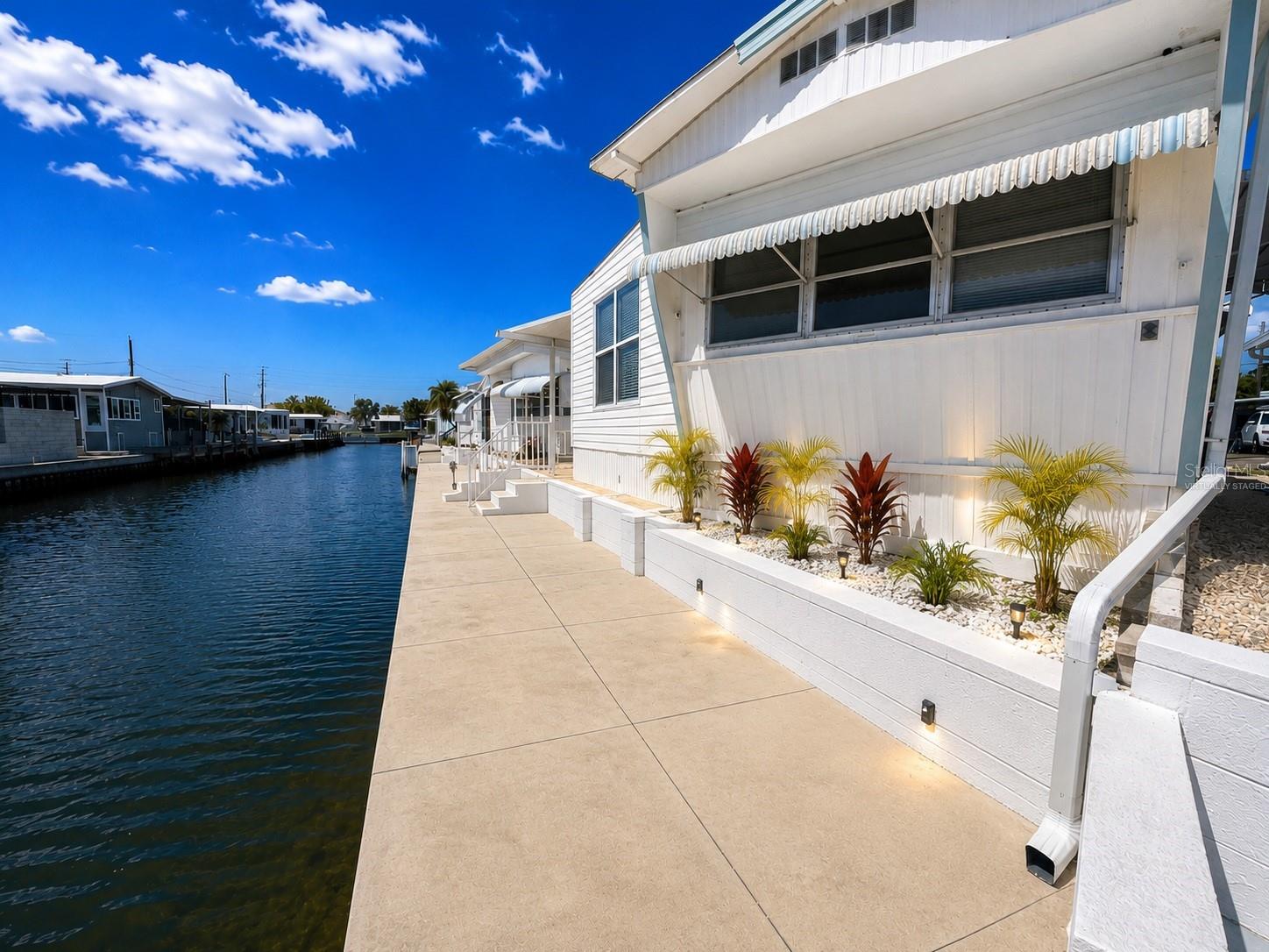 Virtually Staged. Wake up to the peaceful beauty of waterfront living in this spacious 2-bedroom, 2-bath home offering 1,561 square feet under roof. Perfectly positioned on a canal with glimpses of Sarasota Bay, this home offers the opportunity to enjoy Florida waterfront living every day.

The waterfront is the heart of this property. The private concrete seawall creates the perfect place to set out a couple of chairs and unwind while watching boats pass by, enjoying spectacular sunsets, casting a fishing line from your own property, launching a kayak, paddleboard, jet ski, or boat, or simply embracing the waterfront lifestyle.

Inside, the living space is expanded by a bright addition with vinyl windows, creating the perfect place to relax while enjoying the canal and Sarasota Bay views. The home also features a spacious primary bedroom with a private ensuite bath, providing a comfortable retreat for owners and guests alike.

Recent improvements include a new air conditioning system and all-new ductwork, providing added peace of mind. A covered carport offers convenient parking and additional outdoor living space.

Located in Trailer Estates, a Special Park and Recreation District governed under Chapter 418, Florida Statutes, residents own their land with no lot rent, CDD, or HOA fees. The annual park tax covers cable, high-speed internet, trash pickup, fire and rescue services, and access to outstanding amenities including a marina with rentable boat slips, private beach, pool, hot tub, fitness center, shuffleboard, bocce ball, pickleball, woodshop, and nearly 60 active clubs and social events. Experience one of Sarasota Bay's most vibrant and welcoming 55+ communities.

Propety sells furnished. Patio set and potted plants not inlcuded. Some shrubs are virtual. Buyer responsible for verifying measurements and details.