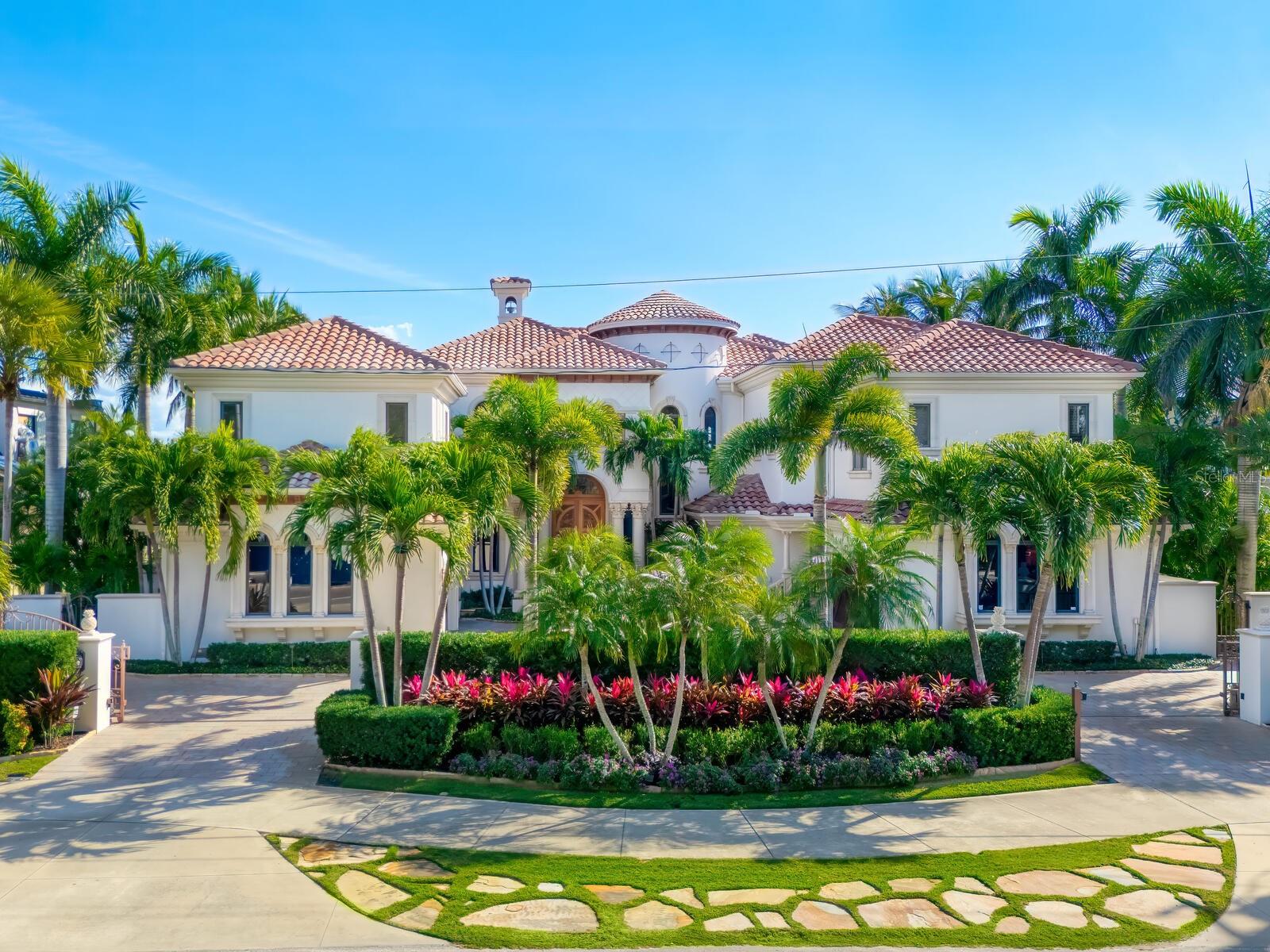 Live your luxury at Casa Lido, a spectacular waterfront estate in the enclave of Lido Shores, offering sweeping, unobstructed views across Sarasota Bay to downtown Sarasota and iconic Ringling Bridge, while having private beach access. This is a rare opportunity to own a residence of extraordinary scale, presence and craftsmanship, where every detail has been custom-designed and executed at the highest level. A private, gated drive leads to a dramatic custom arched wooden double door entry opening to a two-story grand foyer, setting the tone for the home’s impressive proportions and architectural sophistication. Soaring ceilings, refined millwork, curated chandeliers and walls of glass frame the open bay views, while electric screens allow you to enjoy uninterrupted vistas throughout the day without sacrificing comfort or privacy. Spanning an exceptional amount of square footage, the residence offers five bedrooms, five full baths, four half baths and a thoughtfully designed layout that balances grandeur with livability. Two dedicated office spaces include a stunning wood-paneled office with a spiral staircase leading to a second-story library, complete with custom bookcases and a charming tucked-away nook, ideal as a child’s hideaway or creative retreat. The first-floor primary suite is a sanctuary, featuring oversized dual walk-in closets and a spa-inspired bath designed for effortless daily living. Wake each morning to tranquil water views and the gentle rhythm of the bay. An additional private office adjoining the suite offers an inspiring workspace with panoramic scenery. Designed for entertaining at every scale, the chef’s kitchen is anchored by premium appliances, an expansive island, a butler’s pantry, dual dishwashers and seamless flow into the family room. Pocketing sliders open to the outdoor living areas, blurring the line between indoors and out. Wellness and leisure are elevated throughout the home, including a private gym with sauna, a temperature-controlled wine room and storage, and a fully equipped entertainment room with theater seating, wet and dry bars, and game space. Upstairs, spacious guest suites enjoy refined finishes and access to wraparound balconies with a gas fireplace. ideal for sunset views over the water. Guests will appreciate the separate guesthouse, featuring a private entrance, living area, kitchenette, dedicated laundry, en-suite bath and serene water views, ideal for extended stays or multigenerational living. Outdoors, the estate continues to impress with upper and lower resort-style pools, a fire pit, outdoor kitchen, and multiple spaces for dining and relaxation. Boating enthusiasts will enjoy direct bay access from the private dock, complete with lifts and accommodations for watercraft and paddleboards. Every space in Casa Lido is oversized, intentional and undeniably grand, a home that must be experienced in person to fully appreciate its scale, finishes and commanding presence. Just minutes from St. Armands Circle, world-class beaches and downtown Sarasota, this is waterfront living without compromise.