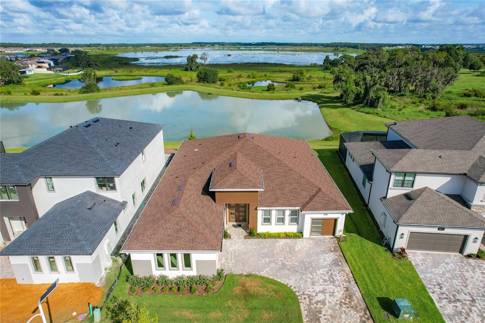 Contemporary masterpiece with wide expansive lakefront views and beautiful sunsets year round. Located in the first of its kind tropical Epperson Ranch Lagoon community. One of the best elevated premium lots with unobstructed views from the Master bedroom, main room and dining room and kitchen, overlooking the beautiful king lake! This incredible one-story layout boasts the perfect blend of four spacious bedrooms, plus a separate office space, three striking baths, a formal dining space adjacent to the kitchen, as well as a large great room that opens to the backyard with four-panel sliding glass doors. This stately home offers highly durable, hypo-allergenic, long-lasting LVP floors throughout bedrooms. The exquisite chef’s kitchen, with upgraded cabinets to the ceiling, is highlighted by a massive island with quartz countertops, a corner pantry and elite stainless steel appliances, including a built-in oven and a gas cooktop with a custom hood vent. The luxurious owner’s suite features its own sitting area overlooking your stunning water views, boasting an incredible bath with a large glass walk-in shower, elegant free-standing, plumbing for deep soaking tub and dual sink vanity, all of which leads into the master closet. Additional features include a large, covered rear paver screened patio, Top of the line Coyote outdoor kitchen with Concrete countertop with two grills (propane and charcoal) and sink, front paver driveway, mudroom with built-in lockers, upgraded windows, 10-foot ceilings, 8-foot interior doors and stylish panel garage doors. This home also contains a three-car split garage set up. Gutter, Vivint security system, water softner are all installed and included in the sale. Located on a premium lot in the award-winning, gated Epperson Ranch community with expansive king lake views out the back of the property. Epperson Ranch features the nation’s first crystal lagoon of 7.5 acres of clear blue water, including sandy beaches, a swim-up bar, as well as UltraFi, a community-wide internet and cable experience, solar streetlights, golf cart paths, miles of fitness trails, green spaces and dog parks. This growing area also has the sought-after Innovation Preparatory Academy and The Kirkland Ranch Academy of Innovation schools while close to the shopping and dining of the Tampa Outlets and Shops at Wiregrass.