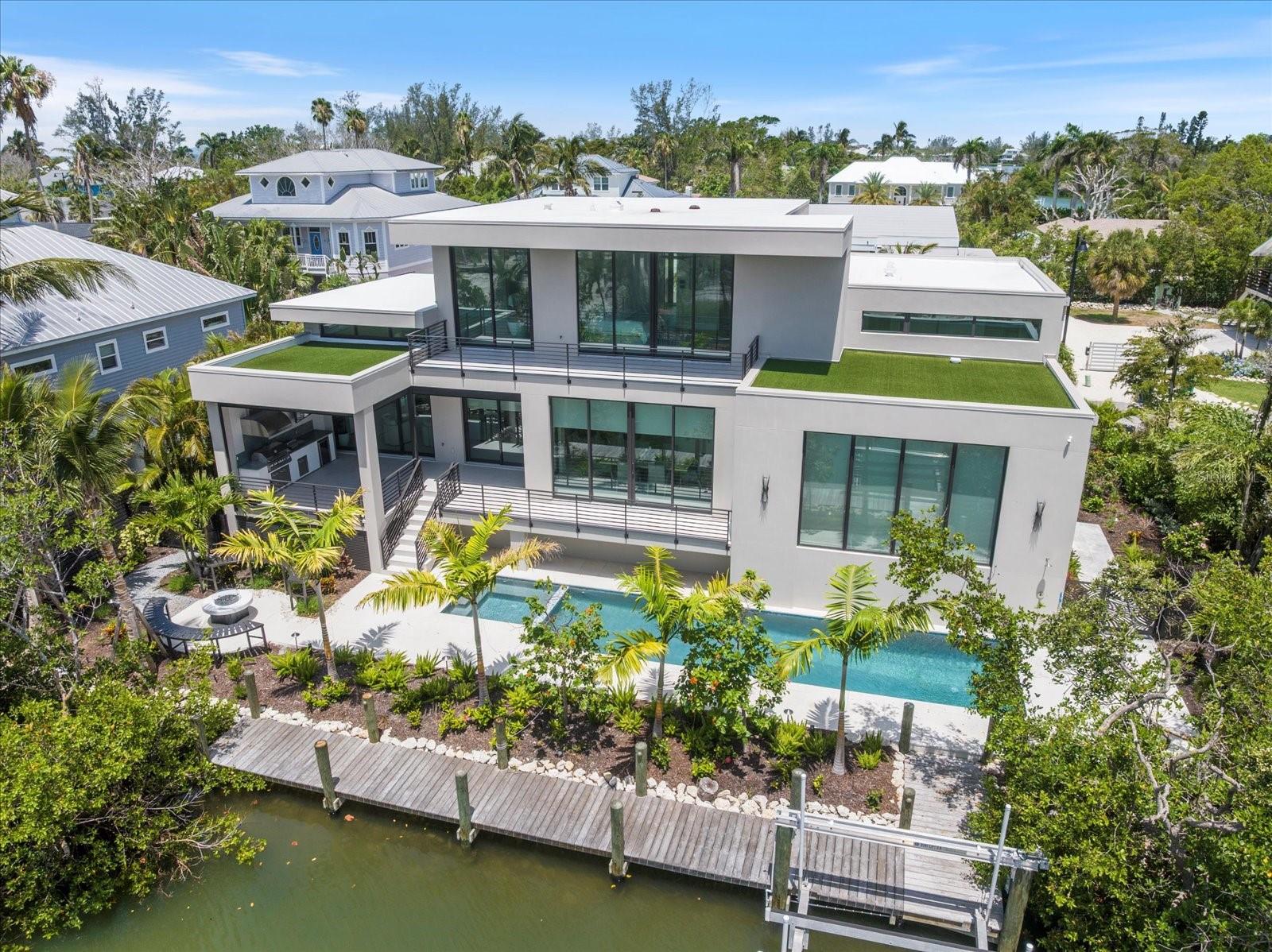 Step into a new era of coastal modern living with this breathtaking, newly constructed waterfront retreat, perfectly positioned on the exclusive north end of Longboat Key. Designed with intention and offered fully turnkey-furnished, this residence is a refined sanctuary where architectural elegance meets cutting-edge technology and relaxed sophistication. The grand entry leads into a dramatic great room, showcasing driftwood-accented ceilings and expansive floor-to-ceiling windows that flood the space with natural light. From here, the home flows effortlessly into the open dining area and chef’s kitchen, where rich wood-tone custom cabinetry, premium appliances, and clean modern lines create an atmosphere of understated luxury. Just off the dining space, you’ll find an expansive entertainer’s room with its own full bath—ideal for hosting dinner parties, events, or enjoying a night in with guests. Upstairs, the home’s private quarters await. Bedrooms two and three are located on the second level, while the third floor is reserved entirely for the primary suite, accessible by private elevator. This executive-level retreat features multiple walk-in closets, serene private balconies overlooking the water, and a spa-inspired primary bathroom designed with curated finishes and timeless style. Throughout the home, attention to detail is evident in every finish and feature—including a full Lutron lighting system, motorized shades, integrated surround sound, and a Brinks security system with CCTV monitoring. Outside, the coastal lifestyle truly comes to life. Enjoy a resort-style pool, fire pit lounge, and a brand-new private dock just a few homes away from open water—offering easy access to the Gulf and endless boating adventures. This property was crafted to bring people together, whether relaxing with family or entertaining in style.