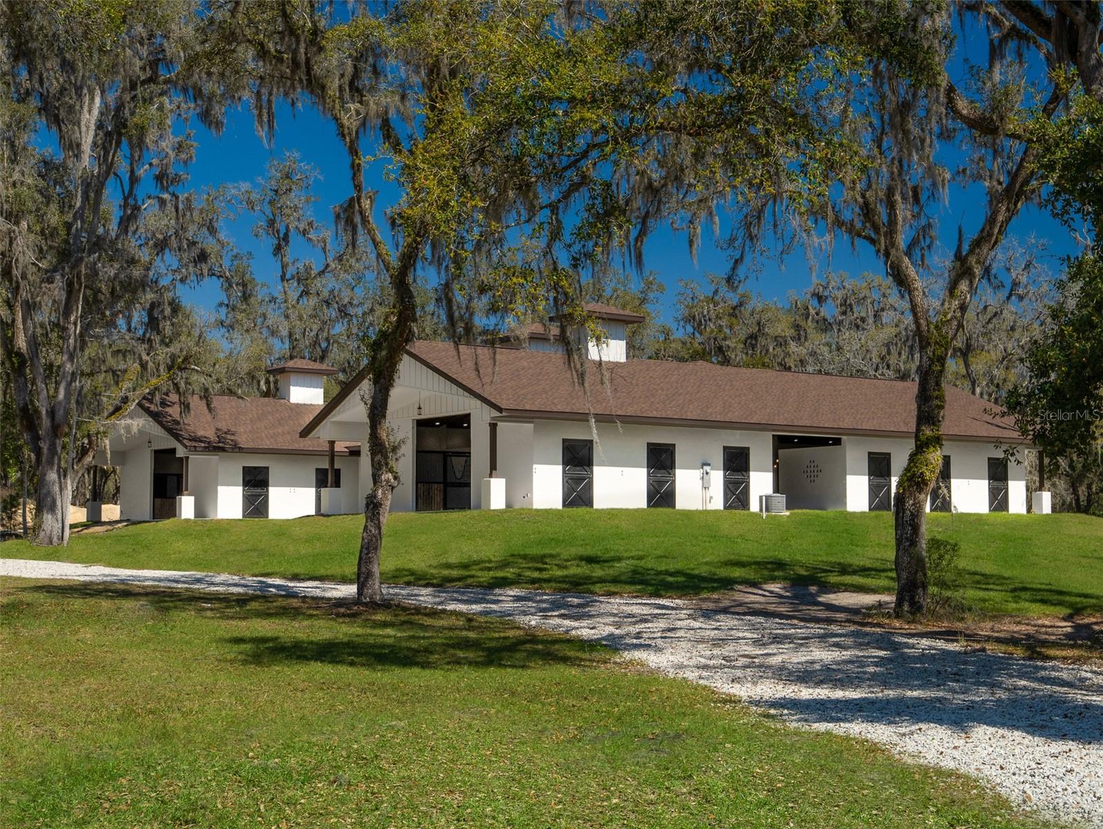 This 26.77-acre property, featuring stunning live oaks and magnolias, is a prime opportunity for equestrian enthusiasts seeking both privacy and convenience! Located just 5 minutes from HITS and 15 minutes from the World Equestrian Center, it boasts a high-end, 20-stall H-style barn with 12,050 sq. ft. of finished space. The barn includes spacious aisles, rubber pavers throughout, fans, sliding front stall doors, and rear Dutch doors, along with two air-conditioned tack rooms and a feed room. Additional amenities include 8 grooming/wash stalls, a 150'x250' Wordley Martin riding ring with irrigation from a dedicated well, and a cement curb along the perimeter. The barn also features a kitchenette with granite countertops, a dishwasher, refrigerator, and microwave, as well as an adjoining bathroom. A large laundry room with dual hookups and ample cabinet space further enhances convenience. Plans for a custom 5,886 sq. ft. home by Rispoli Architects are also included. The property is fully fenced, with options for paddocks and outbuildings, offering the perfect balance of seclusion and easy access to top equestrian facilities. NW 115th St is a private, paved dead-end road, lined with newer horse farms on parcels of no less than 10 acres each, and Spectrum has recently installed cable for both internet and cable services, adding to the property's appeal.
