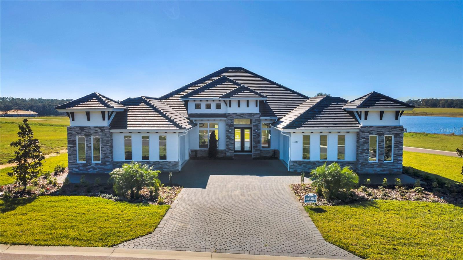 A rare blend of privacy, elegance, and effortless modern living, without the wait. Welcome to The Monica, a showcase of architectural grace and thoughtful craftsmanship. Set on more than half an acre in the exclusive gated enclave of West Hills Estates, this single-story residence spans nearly 3,500 square feet and embodies the art of refined Florida living: spacious, sunlit, and serenely private. Beyond its stately elevation and four-car garage, every detail has been curated for those who appreciate both beauty and purpose. Inside, the grand foyer opens to formal and flexible spaces, an elegant dining room for memorable gatherings and a study that invites quiet reflection or inspired work-from-home moments. The heart of the home unfolds in an expansive open layout where the living area, kitchen, and breakfast nook flow effortlessly together. Double sliding glass doors blur the line between indoors and out, filling the home with natural light and tranquil views. The chef’s kitchen is a masterpiece of function and style, featuring soft-close cabinetry, premium stainless steel appliances, a walk-in pantry, and generous counter space that makes entertaining a joy. The primary suite is a private sanctuary with dual walk-in closets and a spa-inspired bath complete with dual vanities, a soaking tub, and an oversized walk-in shower. Three additional bedrooms are thoughtfully positioned for comfort and privacy, each with its own or nearby bath, ideal for family or guests. Nestled amid the rolling hills and pastoral beauty of Dade City, West Hills Estates offers the peaceful charm of Old Florida living while keeping you close to the conveniences of Wesley Chapel, Tampa, and major thoroughfares. Here, the sounds of nature replace city noise, and every sunset feels like a private escape. Discover a life of space, serenity, and sophistication - your new custom home awaits in West Hills Estates.