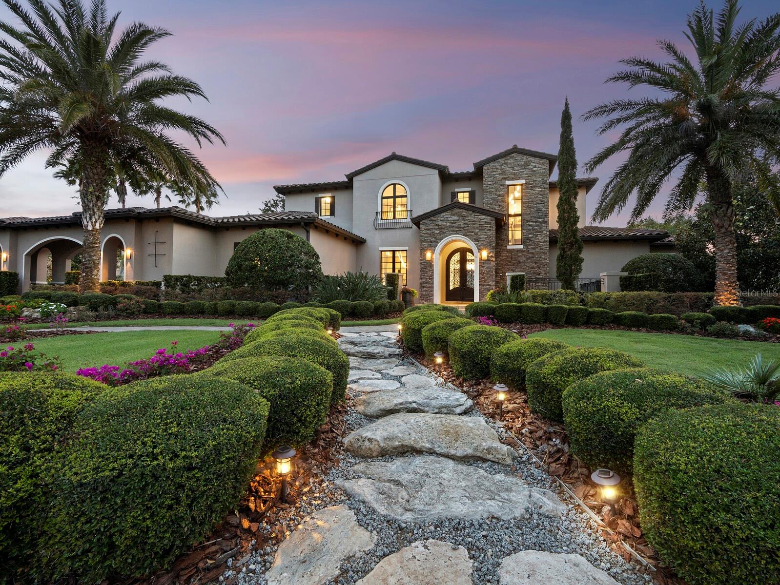 Welcome to a truly distinctive residence, masterfully envisioned by acclaimed architect Francis Rodriguez and expertly built by Nutter Construction. Located in the exclusive, gated enclave of The Lake Club in Lakewood Ranch, this remarkable home offers a secure and serene lifestyle, ideal for those seeking refuge from hurricane threats. Spanning nearly 5,000 square feet of air-conditioned space, the home features 4 spacious bedrooms, 3.5 luxurious bathrooms, and 4 climate-controlled garage bays (one with a lift for two vehicles), all set on a pristine half-acre lot at the end of a quiet cul-de-sac. Privacy and quality craftsmanship define every inch of this exceptional estate. From the moment you arrive, the home’s elegance is unmistakable. A stone-accented porte-cochère and stately cast iron double doors set a sophisticated tone. Inside, imported limestone flooring from Alicante, Spain, and soaring 12-foot ceilings with wood-beamed accents create a warm yet refined atmosphere. Every element—from impact-rated windows, doors, and sliders to the premium Viking appliances in the chef’s kitchen—has been thoughtfully selected to offer the highest level of luxury and resilience. The primary suite, situated on the main floor, offers a serene retreat with a spa-like bath featuring a soaking tub, walk-in shower, and expansive closets. Step through to your private patio—a peaceful spot to enjoy a coffee, meditate, or watch the sun dip below the horizon. Upstairs, a second terrace reveals stunning views of the manicured landscaping and tranquil lake beyond. Outdoors, the west-facing patio—with electric screens to keep open for unobstructed views and closed when needed—boasts an elegant pool, spa, and waterfall. Entertain with ease thanks to a fully outfitted outdoor kitchen, perfect for casual get-togethers or elegant evenings under the stars. Designed with flow and light in mind, the floor plan delivers seamless transitions between spaces, making everyday living effortless and enjoyable. As a resident of The Lake Club, you’ll have access to an unmatched array of amenities, including the Grande Clubhouse, dual swimming pools, game and billiards rooms, fitness and wellness facilities, tennis and pickleball courts, and a gourmet dining room with an on-site chef. With 24-hour guarded security, you’re free to explore the scenic walking trails, lush parks, and sparkling lakes in complete peace of mind. For those seeking a refined lifestyle in a fortress-quality home away from Florida’s coastal risks, this property is an extraordinary sanctuary of style, strength, and seclusion. Make this exceptional residence your safe haven.