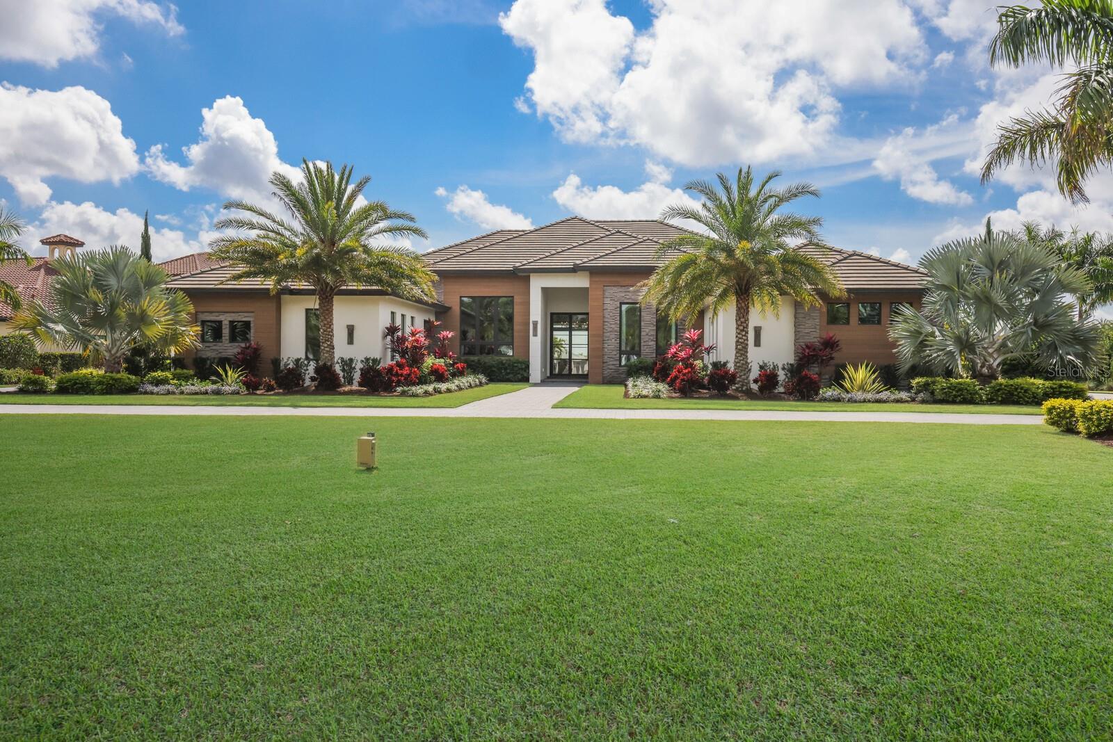 Designed with a nod to the modern movement of architectural styles and positioned on a scenic 1.71 acres in the exclusive and sought-after gated community of The Concession, this residence showcases clean lines, exceptionally planned indoor-outdoor spaces, and the latest in smart home technology. Voted “Best Overall Home” by Parade of Homes in 2021, the former Newcastle model was built by John Cannon encompassing 4,814 square feet of generously proportioned one-story living including private casita, and an expansive outdoor retreat encompassing 2,806 sqft screened lanai with extensive open and under cover spaces grounded with deep gray slate pavers, soaring accent ceilings, full summer kitchen, lounging chaise deck, putting green, fire pit, PebbleTec heated saltwater pool/spa with sun shelf, panoramic clearview screen, and a separate nature viewing deck to enjoy the lake views beyond. 10' accordion-styled impact glass walls with black iron horizontal lines seamlessly connect the resort-styled outdoor living space to a grand great room with sumptuous hardwood flooring, gas fireplace and stunning beam-accentuated ceilings. Dinner guests are treated to an open feel surrounded by disappearing cornerless glass doors and an all-glass temperature-controlled wine room with backlit agate accent wall.  Meanwhile chefs will delight in the oversized kitchen with show-stopper sized windows, two separate marble islands, Albrecht wood cabinetry, a hidden pantry with built-in cabinetry, and all high-performance appliances. An impressive club room directly off lanai beckons for entertaining complete with built-in beverage center, luxuriant ceiling design and direct access to an open courtyard. Relax and unwind in the owner’s quarters positioned on a private wing, offering a spectacular ceiling treatment, large scale windows overlooking the lake, direct lanai access, two oversized walk-in customized closets, and a luxuriously appointed bath with two separate vanity station wings anchored by an oversized all-glass dual entry shower at its center, a jetted tub surrounded by walls of glass looking into a private courtyard with outdoor shower, and even two separate water closets. The private casita off the lanai is optimal for guests with its own morning bar, walk-in closet, private full bath, volume beamed ceiling and stunning views. On a separate wing of the home there are two additional guest suites generous in size, both with walk-in closets and connected to private full baths.  The residence also offers an impressive office behind double-entry doors with elevated step up area, built-in shelving and accent sconce lighting.  Other notable highlights of this 7,704 total square foot residence includes a brilliantly located laundry room with cabinetry, sink, and desk area, Navien tankless water heater, built-in mudroom area, a dual split side load 4-garage, one with an air-conditioned wall unit, and Control4 home automation and networking system unifying lighting, audio, video, climate control, and security. This bespoke offering defines modern refinement beckoning a lifestyle fulfilled in this renowned community infamous as the home to the World Golf Championship PGA golf tournament in February 2021, to the World Champions Cup in December 2023, and to its striking oak hammocks, pines and large lakes, all near dining, shopping, polo, events in the vibrant Lakewood Ranch and UTC area, yet still nearby to the enriching culture and beaches of Sarasota