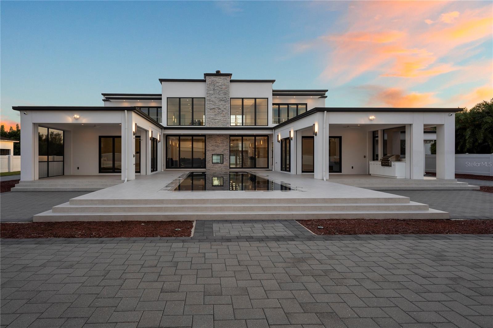 Experience the epitome of modern luxury living, where the fusion of location, style, innovation, and automotive excellence culminates in a masterpiece of architectural prowess. Nestled within the popular Dr. Phillips area, renowned for its upscale living and vibrant community, this custom home by Phil Kean Design Group redefines the essence of refined living. From its sleek exterior showcasing clean lines and premium materials to its meticulously crafted interiors, every detail reflects a harmonious blend of luxury and functionality. Floor-to-ceiling windows invite natural light, seamlessly blurring the boundaries between indoor and outdoor spaces, while minimalist aesthetics create an ambiance of timeless elegance. This fully automated home will do things for you seamlessly integrating technology to anticipate and fulfill your needs, offering unparalleled convenience and comfort. At the heart of this architectural marvel lies the pride of automotive enthusiasts—a 2,365 sq.ft. climate-controlled auto residence with space for 10-12 cars designed to showcase automotive excellence, and transform the conventional garage into a display area to showcase the automotive masterpieces where each vehicle is not just stored, but celebrated as a work of art. Upon entering, the grand foyer welcomes you, setting the tone for the entire home with its minimalist elegance. The open-concept layout seamlessly integrates living spaces, creating an inviting atmosphere for relaxation and entertainment. A two-story stone fireplace serves as a captivating focal point with its see-through feature offering an elegant ambiance from multiple vantage points. The kitchen embodies modern elegance with its clean lines, lift-up Servo Drive cabinetry, luxurious natural quartz countertops, and backsplash, highlighted by a striking island waterfall design and ultra-luxury brand appliances. Its seamless integration of sleek aesthetics and practical functionality creates an inviting space perfect for both culinary endeavors and entertaining guests with style. The master suite, a sanctuary of serenity, features a neutral color palette, soft textures, and a spa-like ensuite bathroom complete with a freestanding tub, walk-in rain shower, and oversized wardrobe room with designated his and her spaces. Ascend to the second level and discover an open loft area designed for elevated entertainment, seamlessly blending contemporary aesthetics with functionality. A custom home theatre, equipped with state-of-the-art technology and an 8-seating arrangement, offers an immersive cinematic experience. Stepping outside, you're greeted by an extension of the home's stylish aesthetic—an outdoor haven boasting a 44 ft. by 15 ft. zero-edge pool with sleek lines and a 6-person spa. With a large sun shelf, it's perfect for soaking up the sun or luxuriating in warm waters, offering an ideal retreat for relaxation and rejuvenation. No details were left behind, from the entrance to the backyard entertaining space every aspect of this home is thoughtfully curated to elevate your lifestyle and provide an immersive living experience like no other. Indulge in the ultimate expression of luxury living, where the perfect harmony of location, style, innovation, and automotive pride awaits. Welcome to a world where every detail is a testament to excellence, and every moment is an opportunity to savor the finer things in life.