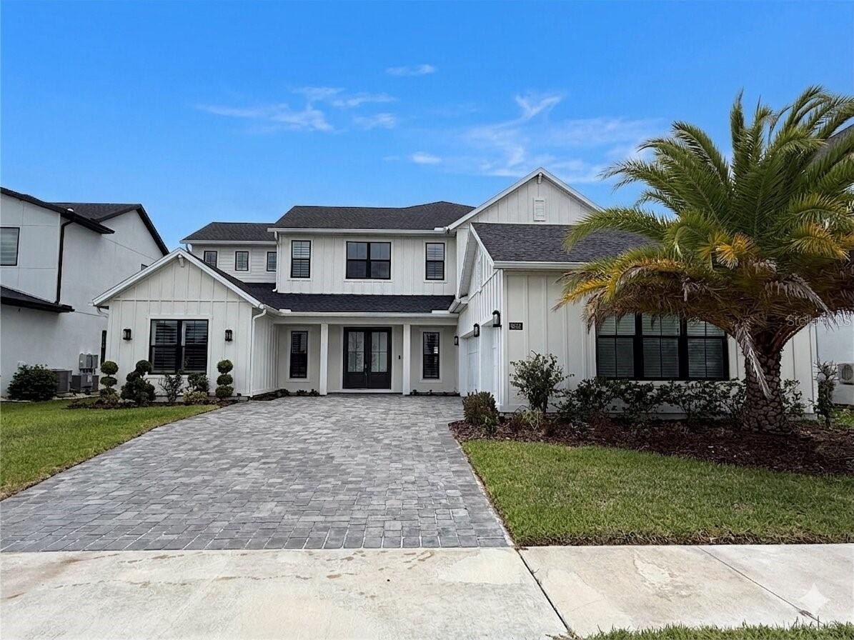 Thoughtfully designed with exceptional attention to detail and overlooking tranquil water views, this extensively upgraded residence in the gated community of Laurel Pointe blends warm contemporary style with functional everyday living. A welcoming front porch and impressive double-door entry open to a dramatic foyer with soaring ceilings, designer finishes, and striking architectural details that continue throughout the home. The spacious great room showcases decorative ceiling treatments, exposed wood beam accents, a fireplace, and custom built-ins with floating wood shelving, creating an inviting focal point for both entertaining and daily living. The kitchen combines beauty and functionality with an oversized quartz island, artisan stone backsplash, premium KitchenAid appliances, solid wood soft-close cabinetry, a large walk-in pantry, and a separate prep pantry. Nearby, the dining area captures views of the pool, water, and outdoor living spaces while allowing for a seamless indoor-outdoor flow. Located near the foyer, a dedicated office/flex space framed by contemporary sliding wood doors with glass accents adds both functionality and architectural character. The first-floor primary suite offers a peaceful retreat with wood beam accents, a custom feature wall, dual walk-in closets, and a spacious bath featuring a soaking tub, oversized walk-in shower, dual sink vanity, and private water closet. A separate downstairs guest suite provides privacy and flexibility for visitors or multi-generational living. Upstairs, the oversized loft with custom entertainment built-ins is surrounded by generously sized secondary bedrooms, including an additional suite with its own private bath, designer accent wall, and window seating area. Plantation shutters, a custom mudroom drop zone, built-in audio in the kitchen, family room, and lanai, upgraded garage flooring with overhead storage, water softener system, and security pre-wire further enhance the home. Designed for year-round enjoyment, the outdoor living area offers an impressive setting for relaxing or entertaining. The saltwater pool features a PebbleTec finish, quartz stone decking, a shallow sun shelf, and a spa finished with dramatic mosaic tile accents. The lanai is highlighted by a cedar plank ceiling, retractable motorized screens and shades, a full cabana bath, and a fully equipped outdoor kitchen featuring a premium Paradise Grill, oversized stainless vent hood, and generous prep space. A covered pergola creates an additional outdoor living space, offering the perfect setting for dining, entertaining, or unwinding while enjoying the pool and water views.