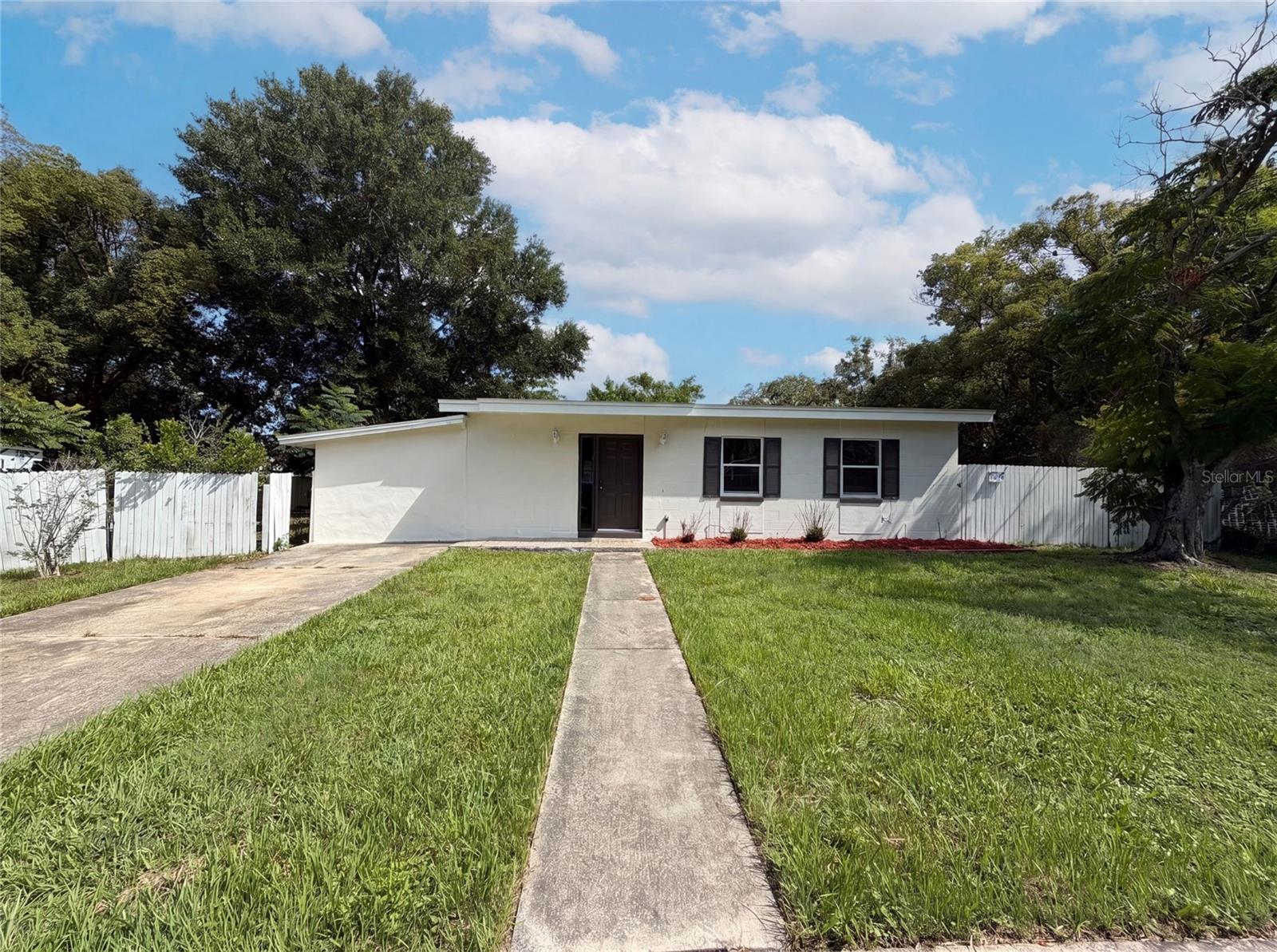 Virtually Staged. 1502 Daroca Dr is a 1-story Deltona single- home built in 1968, set on a roughly 10,900-square-foot lot with three bedrooms and two bathrooms across 1,016 square feet. The kitchen combines granite countertops with dark cabinetry, a tile backsplash, and stainless steel appliances including an electric range, microwave, dishwasher, and refrigerator, opening to the main living space for connected daily use. An open living and dining area sits beneath a vaulted ceiling with a ceiling fan, running on wood-look flooring with a wall-mounted air conditioning unit. One bathroom pairs a vanity with a walk-in shower, while a second full bathroom a vanity and a tile-surround tub-and-shower combination. Wood-look-floored bedrooms with ceiling fans, a fully fenced backyard with a storage shed, and a covered carport complete this single-level residence with practical amenities throughout every room.. Included 100-Day Home Warranty with buyer activation