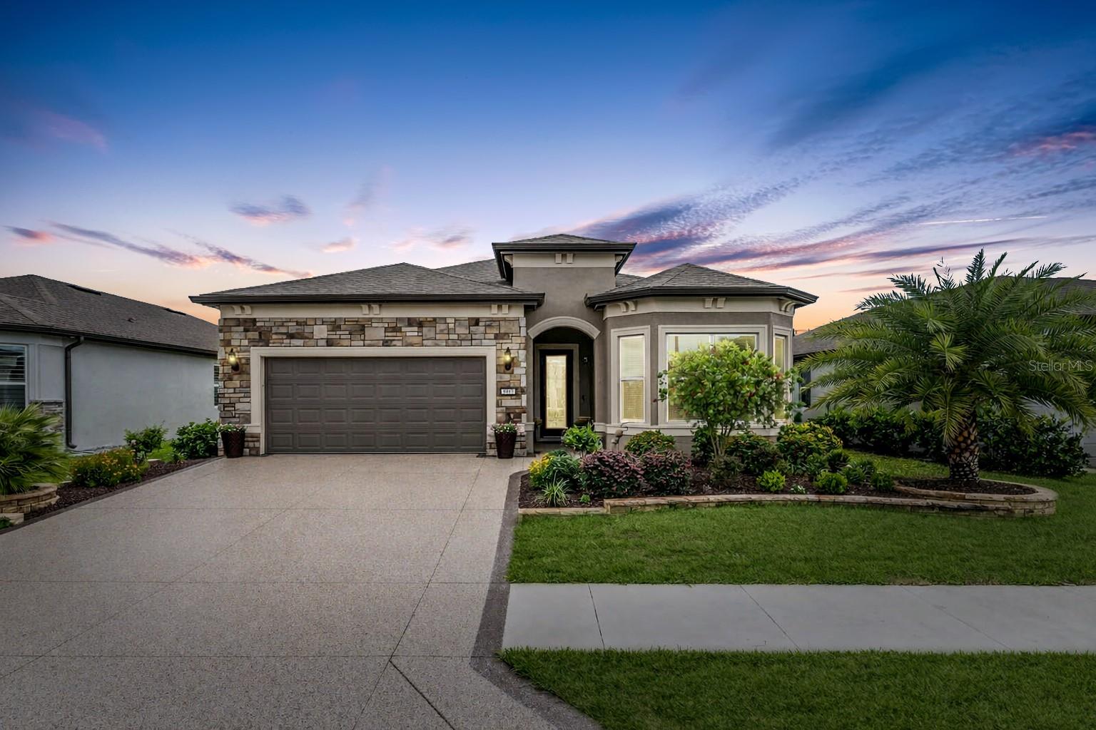 Situated in the gated 55-plus Stone Creek Golf Course Community, known for its luxurious resort-style amenities, this beautifully appointed 2-bedroom, 2.5 bath Prestige model home blends modern sophistication with smart functionality for an elevated living experience. The exterior features a widened driveway, stacked stone accents, professional landscaping, and Trimlight accent lighting that adds a warm, modern glow across the front elevation. A decorative glass front door and retractable screen create a welcoming entry opening into this thoughtfully designed home offering upscale finishes, a flexible bonus room with a storage closet, a glass-enclosed four-season sunroom with heat and air, and a stunning stacked stone-accented foyer. The contemporary layout is perfectly enhanced by lofty ceilings with crown molding, 8’ interior doors, recessed LED lighting, surround sound, and upgraded luxury vinyl plank flooring, creating a seamless flow through the gathering room, café, and kitchen. The gathering room showcases an elegant tray ceiling and opens directly into the bright sunroom, a relaxing spot to enjoy soft northeast morning light. Just outside, a paver-lined patio expands your everyday living with a comfortable setting for outdoor dining, lounging, and effortless entertaining. The chef’s kitchen stands out with a stacked stone accented island ideal for meal prep and casual dining, and crisp Shaker-style cabinetry with upper and under cabinet lighting, soft-close hardware, and convenient pullouts. Gleaming granite countertops, a statement glass tile backsplash, a walk-in pantry with an added electrical outlet, and stainless steel appliances complete this impressive space. The spacious owner’s suite includes a large walk-in closet with pass-through access to the laundry room, and a spa-inspired bath with a granite-topped double vanity, upgraded Roman shower, private water closet, linen closet, and transom window. The secondary bedroom offers a walk-in closet, bay window, and its own full bath. Additional highlights include a guest powder room, a spacious laundry room with cabinets and a sink, a practical mudroom, added ceiling fans, additional closet shelving, a whole-home water softener, and a 4’ extended two-car garage with custom RaceDeck flooring and ample space for a golf cart. Step beyond this thoughtfully designed home and into a vibrant, amenity-rich community where every day feels like a retreat. With a 24/7 staffed gated entrance providing both security and peace of mind, you’ll enjoy comfort, connection, and convenience throughout the neighborhood. Residents have access to heated pools, a state-of-the-art fitness center, a spa, and soothing hot tubs and saunas. Opportunities to stay active are endless with pickleball, bocce, tennis, and a softball field, while a dedicated lifestyle team plans entertainment, activities, and special events that make it easy to meet new friends. Just outside the gates, a beautifully maintained golf course, pro shop, and on-site restaurant offer the perfect setting for socializing and unwinding. Make your move today and experience resort-style living at its finest.