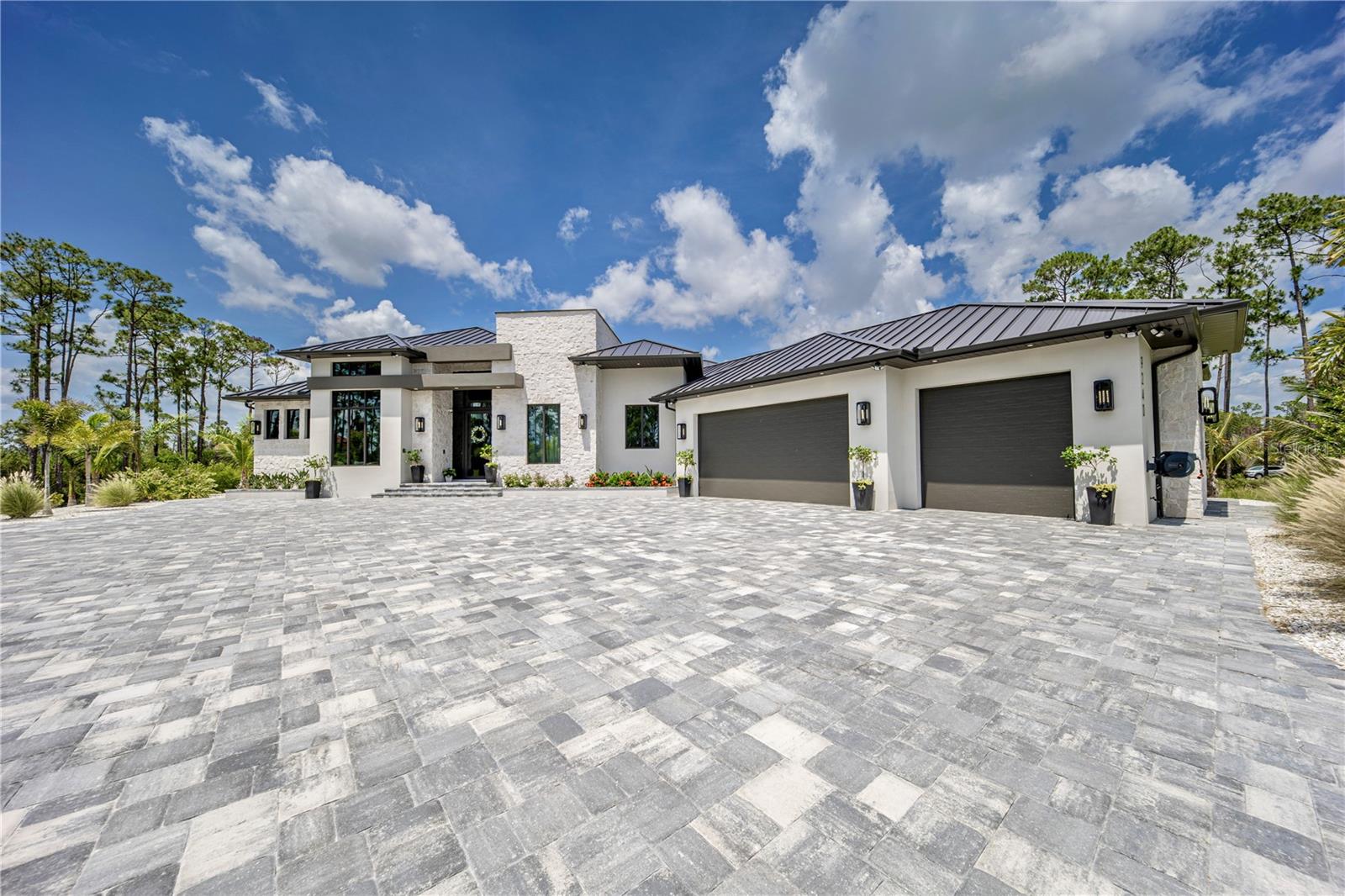 Discover an extraordinary level of luxury in this brand-new 2025 custom-built estate, perfectly positioned on a sprawling over 3-acre lakefront parcel within the prestigious, gated Lake Geraldine community. Offering rare privacy and serenity along the Myakka River, this architectural gem delivers resort-style living with breathtaking natural surroundings, majestic palms, and meticulously designed landscaping featuring fruit trees and a private vegetable garden. Spanning 5,402 square feet of exquisitely finished living space (8,050 total square feet), this 4 bedroom, 5 bathroom residence showcases dramatic 12' to 17' ceilings, creating an open, light-filled atmosphere of grandeur. Every surface reflects uncompromising quality: luxury engineered wood flooring, elegant marble throughout, striking cement-textured Mica walls, and bespoke designer finishes. The exterior stone facade and standing-seam metal roof complete the timeless, sophisticated curb appeal visible in the accompanying photographs.The heart of the home is the true chef’s kitchen, equipped with top-of-the-line Dacor appliances, a luxury gas range, built-in coffee machine with direct plumbed water line, quartzite countertops, and custom white oak solid-wood cabinetry. The expansive pantry can function as a second kitchen, making entertaining effortless. Adjacent spaces include a spacious game room with a mini bar, a dedicated gym, and a large open living area—all enhanced by a whole-home Sonos sound system and cutting-edge Lutron lighting with app control and WiFi mesh networking. The luxurious primary suite offers a private retreat with solid-wood custom closets and a spa-inspired ensuite featuring fully tiled walls, frameless glass showers, and a solid bathtub. Additional highlights include a built-in loft-style bedroom, a sophisticated office with custom cabinetry and seating hidden behind a striking arched iron door, a full-sized custom mudroom, and two laundry areas (including one in the master closet). All bathrooms are fully tiled with glass showers and solid bathtubs. Outdoor living reaches new heights with a large entertainment summer kitchen, paver driveway and sidewalks encircling the home, and an outdoor pool shower. The property is fully prepped for future enhancements: poured footer and gas lines for a future pool, pre-wired and pre-plumbed sauna room, and pre-wired and gas prepped for a future generator. A fully enclosed concrete tornado/safe room (including a concrete ceiling), high impact low-E windows and sliding doors, and the home’s elevated position (2 feet above FEMA minimum) provide exceptional peace of mind. Additional luxury appointments include a whole home reverse osmosis system, 1,000-gallon underground propane tank, upgraded septic system, insulated oversized 3-car garage, central vacuum, two separate tankless gas water heaters, 400-amp electrical service, security and camera system, and window treatments throughout. A full irrigation system covers the entire 3 acres, including the garden area. Low HOA fees include high-speed Hotwire internet, making this turnkey masterpiece as convenient as it is opulent. This is more than a home—it is a private sanctuary where modern technology, timeless design, and Florida’s natural beauty converge in perfect harmony.