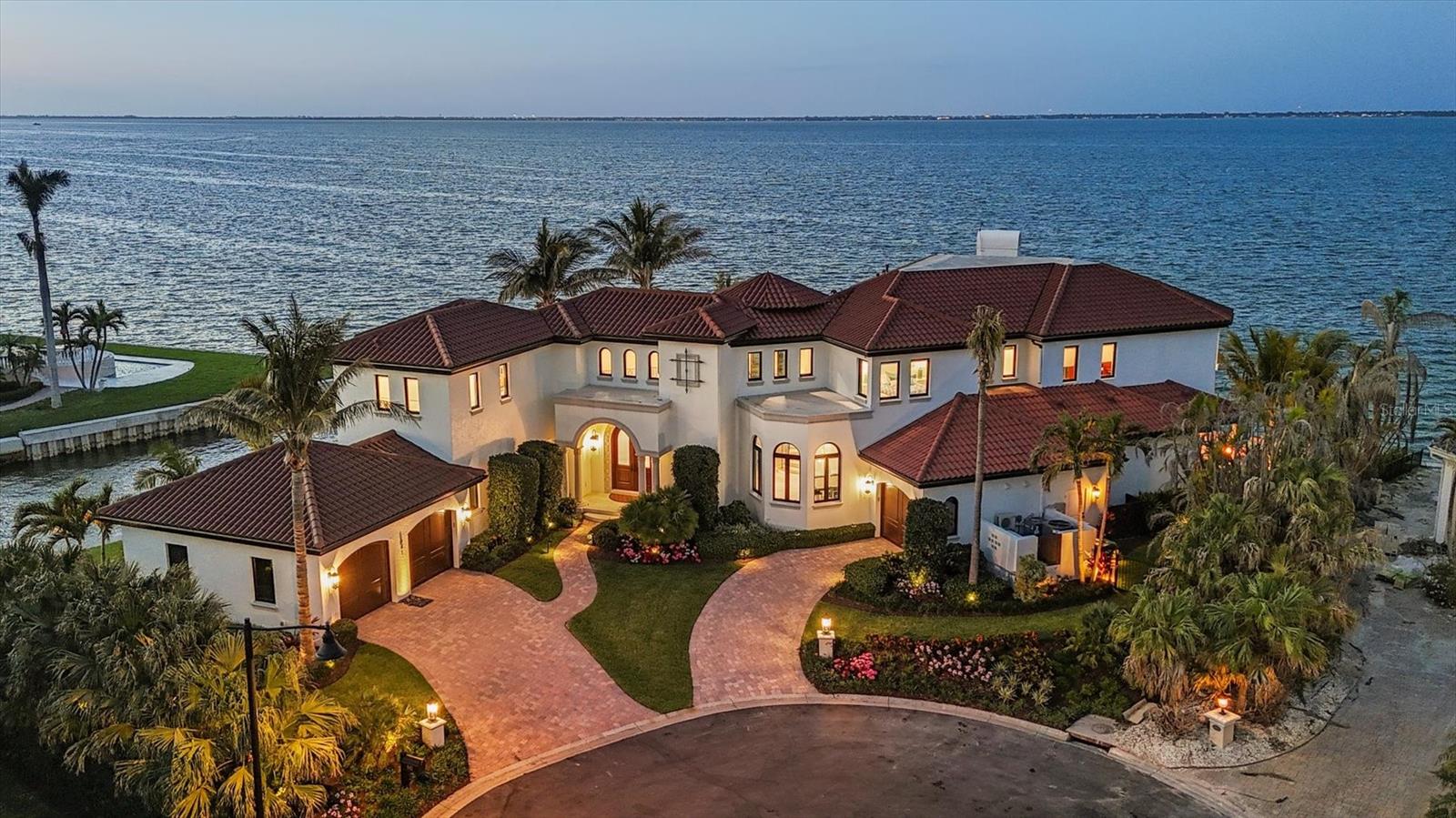 A luxurious coastal retreat at the water’s edge on Longboat Key, 641 Ranger Lane captures the essence of relaxed waterfront luxury. Set on a rare .42-acre corner lot with over 270 feet of prime waterfrontage, this coastal estate offers four bedrooms, 5.5 baths and 7,033 square feet of refined living space. With sweeping views from nearly every room, this home lives as beautifully as it entertains. A dramatic foyer and staircase introduce the home and the craftsmanship throughout. Travertine floors and dark crown molding flow through the main living areas, and a two-stop elevator adds effortless access to all levels. The open-concept great room appeals with a sleek linear fireplace and walls of sliding glass doors that frame the water, blurring the boundary between indoors and out. The beautifully designed kitchen was created with function and flow in mind. Two oversized islands feature seating, dual wine coolers, ice makers and generous storage. The professional-grade Sub-Zero refrigerator, Wolf cooking suite, custom pantry with a built-in coffee station complete with pot filler and coffee pod drawer, and hidden outlets throughout speak to thoughtful luxury. Start your day with coffee in the window-lined breakfast area and end it hosting guests in the elegant dining room with designer wallpaper, a statement chandelier and room to entertain. Step outside to experience island living through a series of outdoor vignettes. A covered area with a wood ceiling and built-in wet bar sets the stage for alfresco dining with coastal breezes. The infinity-edge pool appears to spill seamlessly into the water beyond. Nearby, a hammock sways between two coconut palms, while a fully equipped outdoor kitchen leads to a sunken fire pit lounge, near the seawall for unobstructed views of the bay. With a concrete seawall and ample room for a new custom dock and lift (waiting for installation date), the property is primed for water enthusiasts. The first floor also offers a bonus space— a bunk room—with soaring ceilings, coastal design and sliders to the pool deck. A guest suite features a walk-in closet, designer wallpaper and an en-suite bath. The adjacent laundry room includes quartz countertops, Whirlpool appliances, and generous storage. Upstairs, the primary wing is a sanctuary with double tray ceilings, a linear fireplace, and two private balconies with incredible views. The spa-inspired bath is clad in marble and features a soaking tub, a smart temperature-controlled shower with waterfall fixtures, a makeup vanity and a Toto commode. Dual walk-in closets are thoughtfully designed for form and function. A private office with a wood-paneled ceiling, tile flooring, and balcony access provides a peaceful workspace or retreat with serene water views. Hallways lined with windows of vistas lead to private guest suites with spa-like baths, balconies and water views. A second laundry room and full bath add everyday convenience. Experience the ultimate island lifestyle where coastal sophistication meets everyday serenity. In Longboat Key’s Country Club Shores community with deeded beach access and proximity to golf, tennis and boating, this home offers easy access to The Longboat Key Club, The St. Regis, St. Armands Circle and downtown Sarasota. Recently named one of Forbes Travel Guide’s Top 12 Destinations for 2025, Longboat Key is where waterfront living comes to life.