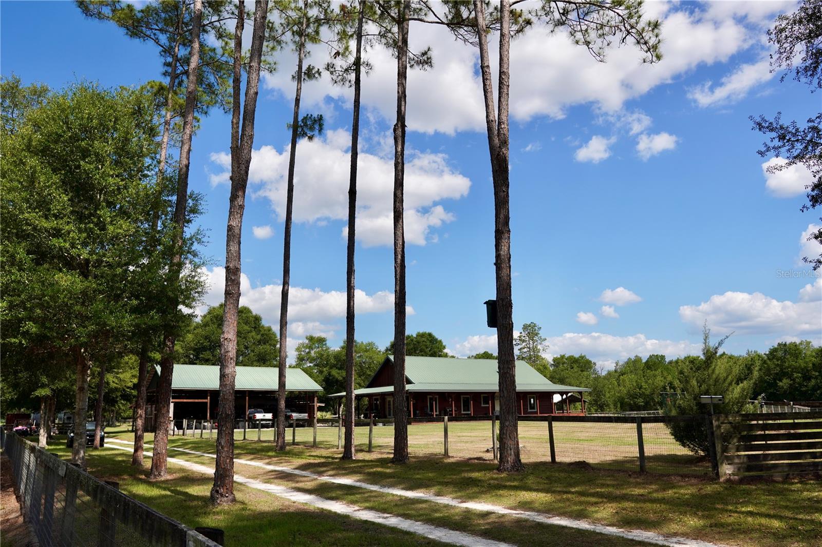 This exceptional gated equestrian estate truly has it all — perfectly blending country charm, privacy, and a prime central location positioned between WEC and Gainesville. Easy drive down Hwy 27 to HITS and WEC. Set well back from the road and surrounded by lush open pastures shaded by majestic oaks. Thoughtfully designed home and property to capture sweeping views of the entire farm, the home offers a seamless connection to the surrounding landscape. Relax on the expansive wraparound porch and enjoy peaceful mornings and stunning sunsets while watching horses graze across the lush, green pastures. Beautiful 3-bedroom, 2.5-bath custom log home showcasing timeless craftsmanship and rustic elegance. The inviting wraparound porch welcomes you into a spacious interior featuring soaring ceilings, stunning live-edge wood trim, and a blend of rich wood and tile flooring throughout. The well designed chef’s kitchen offers granite countertops, stainless steel appliances, and a gas range, making it ideal for both everyday living and entertaining. A large 4-bay 12’ high and 2 are tandem depth carport provides ample space for trucks, vehicles, equipment, and recreational toys. Another thoughtful feature is the separate fenced and gated yard, providing a safe and secure space for family pets to play and roam while remaining apart from the farm’s larger animals and operations.
Outstanding equine amenities include a matted 12-stall center aisle barn with foaling stall option complete with full bath, laundry, and climate-controlled tack room, plus a matted 4-stall shed row barn with an expansive storage room. Training facilities are second to none, featuring an irrigated all-weather GGT arena approximately 150’ x 250’, an additional irrigated sand arena approximately 150’ x 200’, and a 60’ round pen. Ride off the property on the  trails located at back of property.
The farm is exceptionally well-equipped with 8 paddocks (4 with 5’ fencing), 5 spacious pastures with no-climb fencing and top board, 2 large run-in sheds, and an oversized run-in that could easily convert to 6 additional stalls if desired. Additional amenities include 4 wash stalls with hot and cold water, dual RV hookups (30 amp and 50 amp) with septic, 2 wells, a manual hand pump and 2 septic systems.
As an added bonus, the barn is outfitted with $50,000 in solar panels, offering valuable energy efficiency and long-term savings for the entire property. 40’ steel container rodent proof for hay and grain storage.
Rarely does a farm offering this level of infrastructure, functionality, and versatility come to market at such an affordable price. Williston is thriving small town that blends rural charm with everyday convenience. Residents enjoy easy access to feed and hay suppliers, tractor supply, Sparr building & farm supply, local coffee shops, restaurants. It’s the perfect place to enjoy an equestrian and agricultural lifestyle without sacrificing modern amenities.