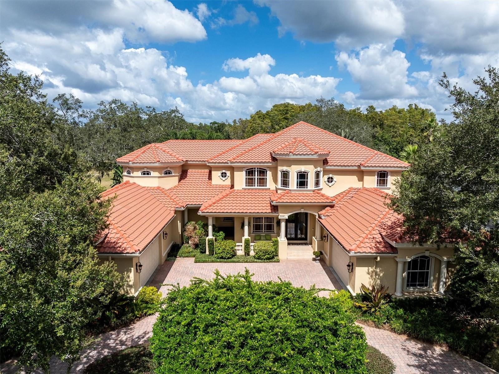Welcome to this exquisite custom-built estate home perfectly situated in the prestigious guard-gated community of Wentworth. Nestled on a quiet cul-de-sac. This two-story Mediterranean masterpiece offers the perfect blend of luxury, comfort, and thoughtful design. Boasting nearly 5,800 sq. ft. of exceptional living space, this home has been meticulously maintained and upgraded with the finest finishes and details throughout. The spacious gourmet kitchen is a chef’s dream, featuring custom cabinetry, granite countertops, a large island, butler’s pantry, breakfast nook, pot filler faucet, and top-of-the-line appliances. The first floor also includes a grand living area with surround sound, formal and casual dining spaces, a billiard room, a dedicated exercise room with equipment that conveys, and a beautifully appointed home theater featuring a 122” screen—equipment and furniture convey. Upstairs, the luxurious master suite offers a private retreat with a sitting area, two custom-built walk-in closets, and a private balcony. The spa-like master bath showcases elegant finishes, creating a serene and relaxing atmosphere. Designed for both entertaining and everyday living, this home features two laundry rooms (one on each floor, with the downstairs updated in 2023), tankless water heater and one traditional water heater, central vacuum system, travertine and wood flooring throughout. The 4-car garage with golf cart garage includes epoxy floors, offering both beauty and function. Step outside to your private resort-style oasis with an extended covered veranda, custom lagoon-style pool, and spa with PebbleTec Ocean Blue finish, three waterfalls, and marble-accented Lightstreams tile (pool renovated 2022–2023, $230k). The outdoor kitchen makes this an entertainer’s paradise, all within a fenced backyard surrounded by tropical landscaping. Additional updates and features include three new A/C units with 10-year warranty (2023), new front door (2024), outdoor lighting (2023), whole-house generator, updated home theater system (2023), ADT security system with cameras covering the entire property, a reverse osmosis system (2024), and a 100-bottle wine cooler. Conveniently located in the East Lake corridor near top-rated schools, beaches, and shopping, this stunning estate truly has it all—luxury, function, and timeless appeal in one of Pinellas County’s most sought-after communities. Must see to apppreciate!