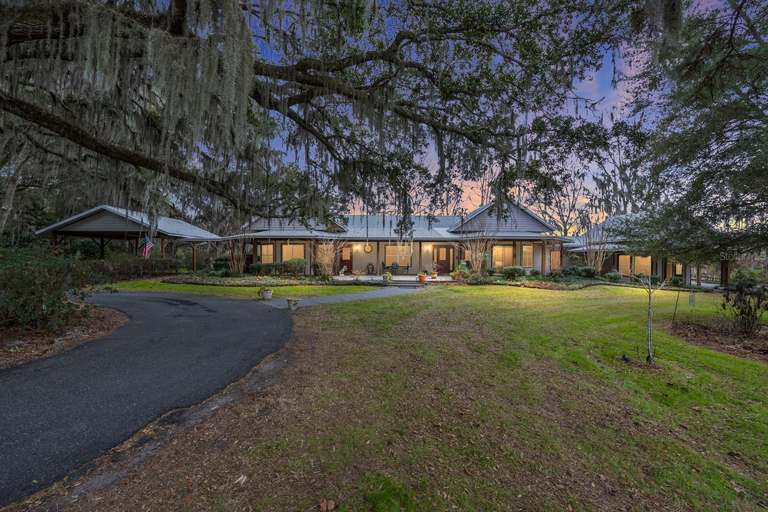 At the end of a long, paved drive — crossing gently over a fish-filled pond — you arrive somewhere that feels set apart from the world.
Welcome to Forever Spring Farm. For more than 20 years, this 50-acre sanctuary has been the gathering place. Custom built with intention and heart, the home was designed not just to live in, but to live fully. Sunlight pours through expansive windows, framing rolling pastures, ancient live oaks, gardens in bloom, and the quiet rhythm of grazing horses. A grand formal dining room has hosted holidays and laughter-filled dinners. A wood-burning fireplace anchors cool evenings. The Florida room at the back and the wide front deck have witnessed countless sunsets, conversations, and celebrations. This is a home where memories were layered season after season. The main residence offers 3 bedrooms and 2 baths, along with a thoughtfully attached mother-in-law suite — perfect for multi-generational living, long-term guests, or private retreats. For the equestrian, the property is as functional as it is beautiful. A 7-stall center-aisle barn includes an air-conditioned tack room, feed room, and bathroom — designed for comfort and practicality year-round. Lush pastures stretch under open skies, while the surrounding woods create a natural backdrop where deer, turkey, and native wildlife wander freely. Tucked privately on the property is the lovingly nicknamed “Happy House,” an income-producing short-term rental that has welcomed guests seeking the same peace the owners found here.  Every inch of this land tells a story — from the mature live oaks standing strong through decades, to the gardens tenderly cultivated, to the quiet pond reflecting morning light. Forever Spring Farm isn’t simply 50 acres with a home and barn.

It’s a place to build a life. To gather. To grow. To ride.  To plant roots. To watch children and grandchildren run under the trees. To create the kind of memories that feel timeless. Some properties are purchased. Others are carried forward.