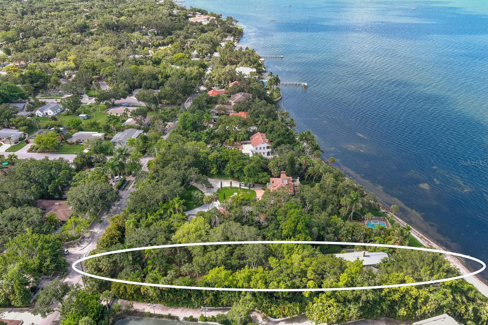 Exotic and extremely private bay front property on the market for the first time in 40 years. In fact, this is only the third time it’s been available in 100 years. Travel back in time to find ancient oaks and large palms, Banyans, and cedars. It’s an idyllic paradise reminding us of why people have come to these shores for millennia. Even the beachfront appears unadulterated as do several others along Sarasota’s north shore. Although this is direct waterfront, most of the land is not in the flood zone creating many possibilities for new structures on or near grade. What is most unique is the 444-foot lot depth. This is almost 4 times that of other bayfront parcels being redeveloped in the area. This extreme distance provides complete privacy from Bay Shore Road and with each adjacent property a multi-acre estate, the feeling of spaciousness and seclusion is complete. Leave the world behind on the long, winding shell drive through tree canopy and lush vegetation. At “the end of the road” is the original homesite on a small bluff directly on and overlooking Sarasota Bay. Your views are of Longboat and Lido Key and out New Pass to the Gulf of Mexico. Looking south you see our bustling little city of Sarasota and the John Ringling Bridge. Enjoy sea breezes in the afternoon and sunsets all year round. The original home on property evokes a bygone era but land values, building codes and FEMA regulations point toward new construction. A parcel like this is an architects dream providing the size necessary to create what anyone might want, elevation allowing cascading terraces down to the waterfront and multiple, potential “footprints” for accessory dwellings, accessory structures and more. Bay Shore Road has become an eclectic location for the grandest homes in Sarasota. This has led to sales over 10 million dollars and have exceeded 15 million. But you could not put a price on the most spectacular neighbor, Ca’ d Zan. John Ringling’s gilded Venetian palace anchors the neighborhood to the north and downtown Sarasota is just 2 miles south. Other nearby cultural & educational institutions include the Ringling Museum of Art, the Asolo Theater of Performing Arts, the Sarasota Ballet, the Ringling College of Art & Design and our newest amenity, The Bay Park Conservancy redeveloping 53 acres of City waterfront into a world class public park.