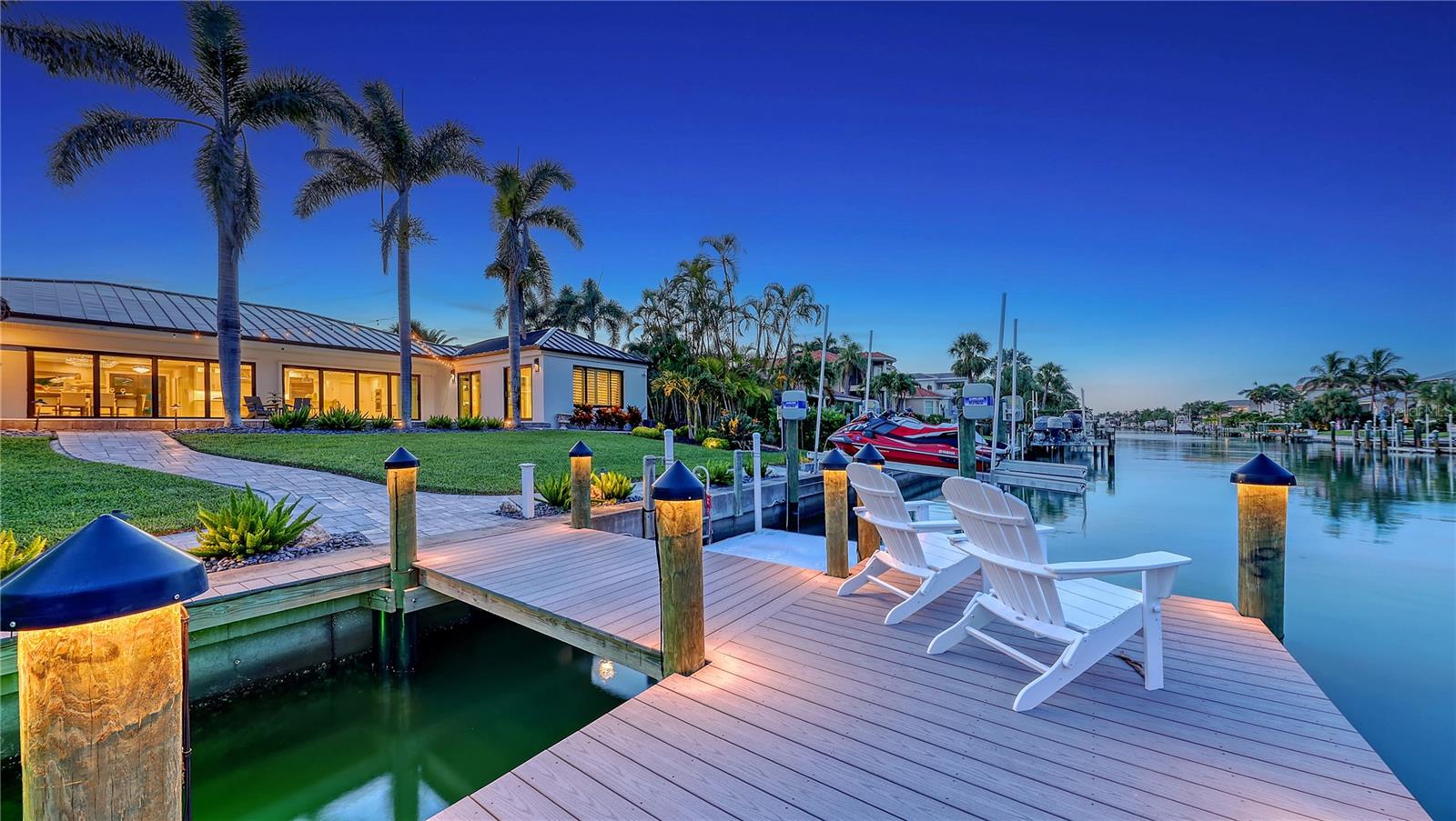 This striking waterfront Bird Key residence delivers a seamless blend of refined updates, thoughtful design, and effortless coastal living. Nestled along a wide canal just moments from Sarasota Bay, this four-bedroom home—with additional office—offers nearly 3,400 square feet of open living space, designed to showcase its serene water views and inviting indoor-outdoor lifestyle.  Noteworthy enhancements include new roof in 2023, hurricane-impact windows and sliders, custom lighting, updated bathrooms, and a paver driveway framed by lush tropical landscaping. Step inside to a light-filled layout where wide-plank tile flooring flows throughout. At the heart of the home, the redesigned kitchen sets a stylish tone with crisp white cabinetry, quartz countertops, a massive island with bar seating, and premium stainless-steel appliances. A secondary counter area doubles as a coffee/wine bar or serving station—perfect for entertaining. The adjacent living and dining room is anchored by a custom paneled accent wall with fireplace and floating shelves, while oversized pocketing glass doors create a continuous connection to the expansive pool terrace and the water beyond. The split-bedroom plan enhances privacy, with the waterfront primary suite tucked away for maximum tranquility. Beautiful water views are complemented by a spa-like bathroom featuring dual vanities, glass-enclosed shower, and generous custom closets. Across the home, three additional guest bedrooms offer versatility. One is currently used as an office with a built-in Murphy bed; another includes its own en-suite bath and patio access—ideal for guests or multigenerational living. Outdoor entertaining takes center stage on the reimagined lanai, where a resurfaced heated swimming pool and expansive newer deck invite relaxation. Dine while relishing bay breezes, enjoy drinks at the custom tiki bar with built-in grill, or unwind at the water’s edge. The 100-feet of seawall (2005), newer dock (2023), dual 7,000-pound jet ski lifts, and 10,000-pound boat lift complete this boater’s paradise. Located on one of Sarasota’s most sought-after barrier islands, Bird Key offers private club amenities (with additional membership to the Bird Key Yacht Club), security, and an unmatched central location. Just minutes from downtown Sarasota’s cultural attractions, St. Armands Circle’s boutique shopping and dining, and the white sands of Lido and Longboat Key beaches, this home is an extraordinary opportunity to live the Gulf Coast lifestyle with every comfort in place.