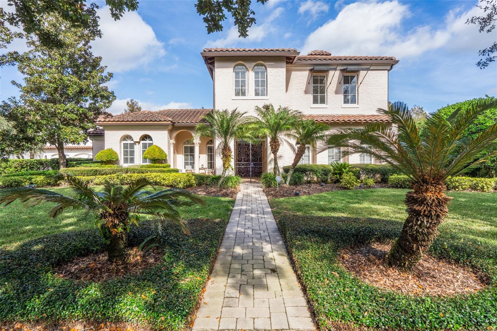 Discover timeless Mediterranean elegance in this rare 6-bedroom, 5-bath estate home, tucked within a quiet cove of Celebration’s prestigious Acadia section in North Village. From the moment you arrive, the home’s stately presence and serene water views set the tone for luxury living. A dramatic entry through wrought-iron gates and twin solid-wood doors welcomes you into the residence, immediately introducing the home’s refined character and architectural grandeur. Inside the main residence, every downstairs space is designed to impress. An elegant great room with soaring ceilings enjoys shimmering views of the tranquil pool, creating a dramatic focal point from the main living areas, the gourmet kitchen, and the luxurious primary suite. The kitchen is richly appointed with upgraded cabinetry, beautiful surfaces, a wine cooler, a butler’s pantry, and premium finishes suited to a home of this caliber. Chiseled travertine flooring and crown molding elevate the home’s warm Mediterranean character. The primary suite offers pool views, an expansive custom walk-in closet, a gas fireplace, and a spa-inspired bath featuring a Jacuzzi tub and walk-in shower. A guest bedroom sits conveniently on the main level. At the rear of the home, the dining room and secondary living room capture peaceful lake views, providing yet another beautiful backdrop for everyday living and entertaining. Upstairs, three additional bedrooms radiate from a loft-style entertaining area complete with a wet bar and built-in desk perfect for movie nights, play space, or a private retreat. Stepping outside, an ultra-private, sun-filled courtyard oasis awaits. A sparkling pool and spa are framed by lush landscaping, a fully equipped summer kitchen with gas grill, refrigerator, and sink, and generous space for outdoor dining and relaxation. Just off the courtyard, a charming one-story guest house offers complete privacy for visitors and easily functions as a pool cabana. A three-car garage provides abundant storage while a wide brick-paver driveway accommodates parking for up to seven vehicles. Full iron fencing and gates surround the property for exceptional privacy and presence. Celebration itself offers an unmatched lifestyle shaped by beauty, recreation, and convenience. Residents enjoy multiple community pools, over 26 miles of scenic walking and biking trails, tennis and basketball courts, playgrounds, and a dedicated dog park. The vibrant downtown area features charming shops, unique dining, lakeside strolls, and year-round festivals and entertainment. With effortless access to I-4, 417, 429, and World Drive, you’re just 10 minutes from Walt Disney World and approximately 25 minutes from Orlando International Airport—perfectly positioned for both everyday living and quick getaways.