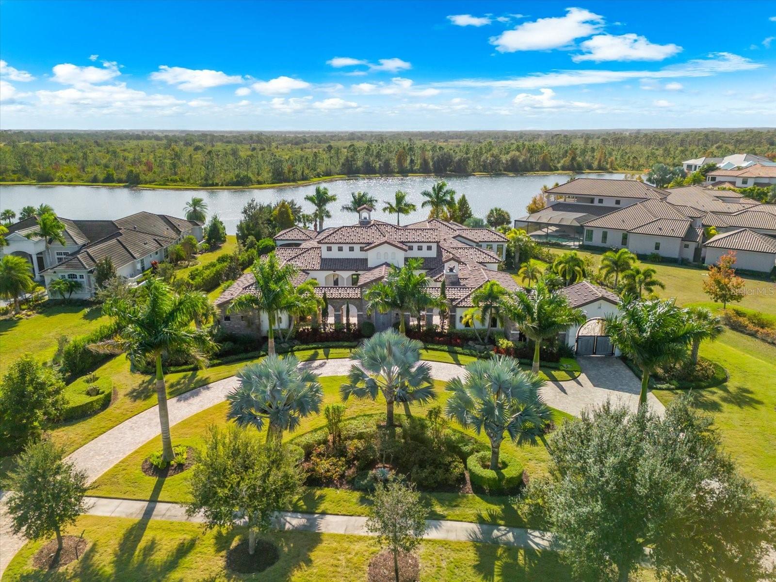 A home like no other, this one-of-a-kind John Cannon estate embodies the art of luxury living in The Concession, one of Lakewood Ranch’s most exclusive gated communities. Set on 1.3 acres of peaceful preserve and water views, this residence blends architectural integrity with thoughtful design, creating an experience that feels both refined and welcoming from the moment you arrive. A grand circular drive leads to double entry doors and a private courtyard with its own fireplace, setting the tone for what awaits inside. Once through the doors, every detail reveals craftsmanship and character; beautiful wood flooring, travertine, and wood accent beams spanning the family room, kitchen, living room, and bonus room. The living room’s statement stone fireplace serves as a dramatic focal point, balancing scale and sophistication.  While the formal dining room, adorned with a mica-flecked ceiling, is an experience of its own ideal for intimate evenings or memorable gatherings.  At the heart of the home, the gourmet kitchen is a chef’s dream, offering Sub-Zero and Wolf appliances, an oversized entertaining island, extensive counter and cabinet space, and a walk-in pantry designed for function and style. Nearby, a climate-controlled wine storage room serves as a striking architectural statement, showcasing your collection with sophistication. The primary suite is a true sanctuary, featuring two custom walk-in closets and a spa-inspired bath designed for serenity—with dual vanities, a freestanding soaking tub, a walk-in shower, and a tranquil waterfall feature that enhances the sense of relaxation. Two additional ensuite bedrooms provide comfort and privacy, while the spacious fourth bedroom is part of an attached casita complete with kitchenette, private entrance, and lanai access, creating the perfect private quarters for guests, extended family, or live-in arrangements. Designed for effortless indoor-outdoor living, the home includes smart home automation, Sonos audio, a richly appointed office, home gym, and a versatile game or bonus room with bar and indoor/outdoor grill area. Expansive sliders open to an outdoor living area defined by cypress-paneled ceilings and graceful architectural columns, creating the feeling of a true extension of the interior spaces, a seamless blend of design and lifestyle that makes this a home like no other. Outdoors, the experience becomes truly unforgettable. The gazebo offers a place to unwind in the evenings before the fireplace, as the glow of firelight reflects across the custom-designed pool with fire features, sun shelves, and a large spa. Framed by serene preserve and lake views, this thoughtfully designed retreat balances beauty, privacy, and sophistication in perfect harmony. The Concession is an elevated luxury neighborhood that is quiet, private, and surrounded by natural beauty, yet just moments from the best of Lakewood Ranch and Sarasota. Residents enjoy proximity to premier shopping, dining, and community events, as well as easy access to Florida’s Gulf Coast beaches, top-rated airports, UTC, and downtown Sarasota. A showcase of elegance, craftsmanship, and livable luxury, this residence redefines what it means to live beautifully in The Concession.
