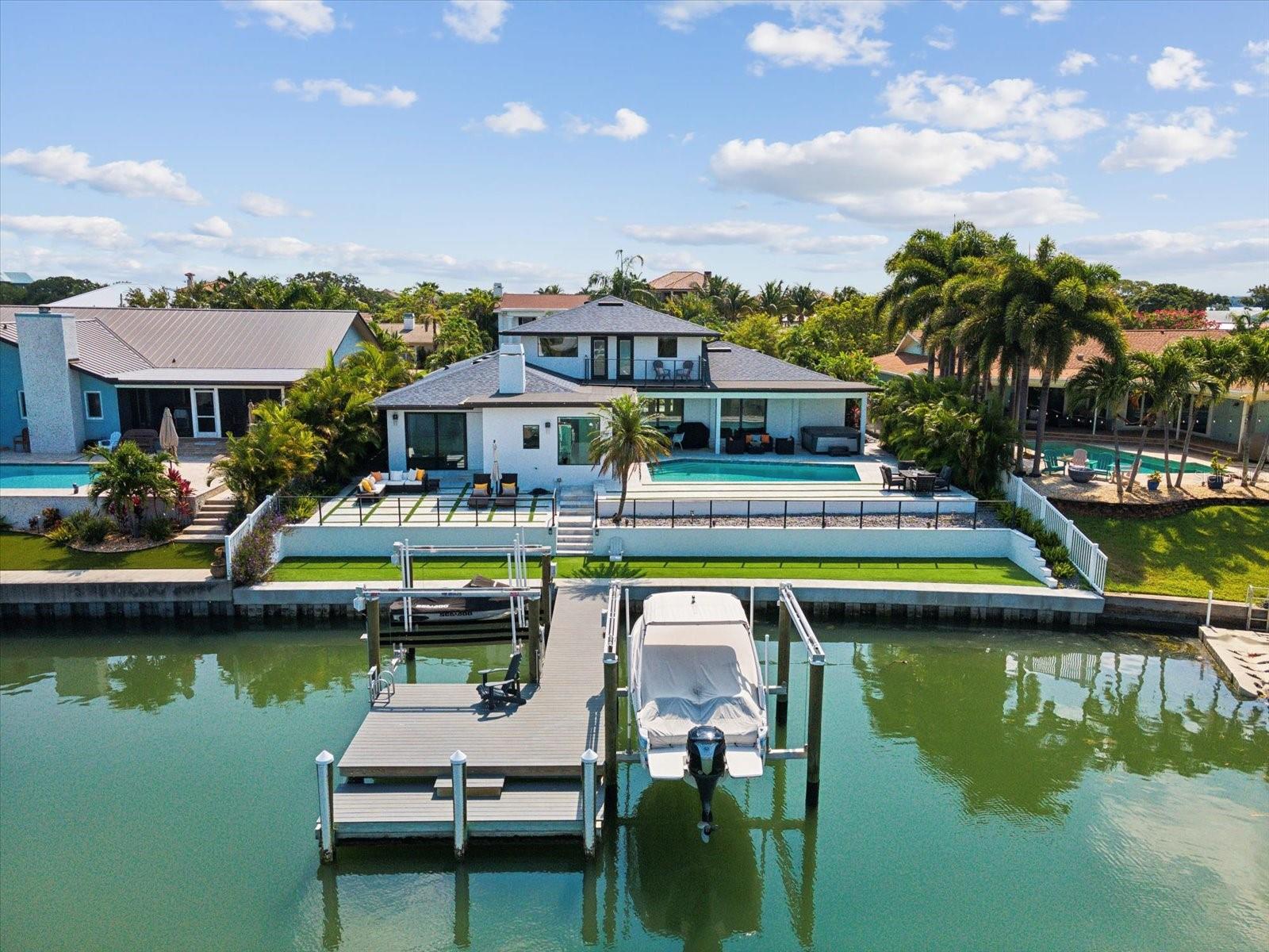Turnkey waterfront elegance at its finest! This 4 bedroom 4.5 bathroom Island Estates home is being sold completely furnished! It sits perched up on an elevated 1/4 acre lot and has recently received an extensive remodel highlighted by a new seawall, new roof, and all new impact glass for peace of mind. A brand new whole home smart system was just installed to include custom electric blinds on all windows and doors, easy control access to security system, lighting, surround sound, HVAC and more. As you approach the home you're greeted with aesthetically pleasing pavers and artificial grass. Upon entry you have an open floorplan filled with natural light and complemented by a gorgeous 180 degree water view. On the main level you have two separate living areas both with ventless fireplaces. They're separated by a dining area and wet bar with ample seating great for large gatherings.The chef's kitchen has been outfitted with designer light fixtures, double oven, twin dishwashers, television, pot filler, vent hood, an abundance of storage and seating for four at the waterfall finished island.  Also located on the main level is the dreamy owner's retreat complete with a 200 sq ft custom built closet, en suite with soaking tub, walk-in shower with twin rain shower heads, wands and large bench for relaxing, dual vanities with LED lighting creating a tranquil ambiance. This retreat provides for the ideal way to wake up and with the touch of a button, raise the blinds and take in the sweeping water views while overlooking the sparkling pool. Upstairs are three guest bedrooms with two additional bathrooms and access to a balcony which offers breathtaking sunset views. A heated AND cooled saltwater pool features custom lighting and is great for entertaining. After a day of boating, rinse off in the outdoor shower before heading inside. Other upgrades include a new composite dock with boat and two jet ski lifts, new electric, water treatment system, epoxy garage floor, upgraded wifi, plumbing upgrades and more. Highly coveted Island Estates is a self-sustained golf cart friendly community that has high-end restaurants, grocery stores, gas station and easy access to the #1 beach in America.