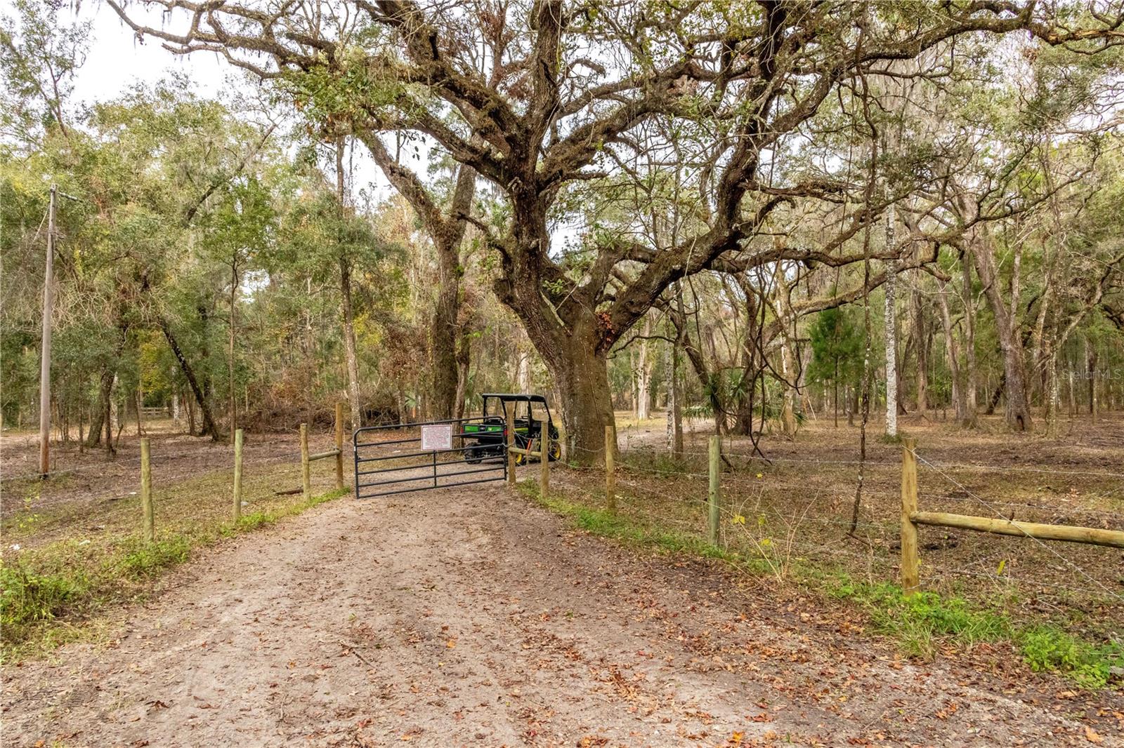 Private 17.3-acre country property with mature oak and pine trees, fully fenced and cross-fenced acreage, and direct access to the Good Neighbor Trail, offering a rare combination of peaceful rural living and convenient access to town. The property includes a massive insulated 42x42 barn with AC and brick floors, and plenty of room for equipment, vehicles, animals, and outdoor recreation. Two separate wells service both the future homesite and barn area for added convenience. The outdoor features make this property truly stand out. Recently under-brushed acreage showcases the natural beauty of the land, with towering oaks and pines creating a scenic and private setting. The fully insulated barn with attached carport provides exceptional space for storage, hobbies, workshops, or recreational vehicles, while the fenced and cross-fenced layout supports a variety of agricultural or outdoor lifestyle uses. Located directly on the paved Good Neighbor Trail, you can bike into town or enjoy miles of scenic riding through Florida's natural landscape while still being just minutes from shopping, dining, and everyday amenities. With expansive acreage, impressive outbuildings, trail access, and the flexibility to create your ideal country retreat, this property offers an outstanding opportunity for buyers seeking space, privacy, and lifestyle versatility.