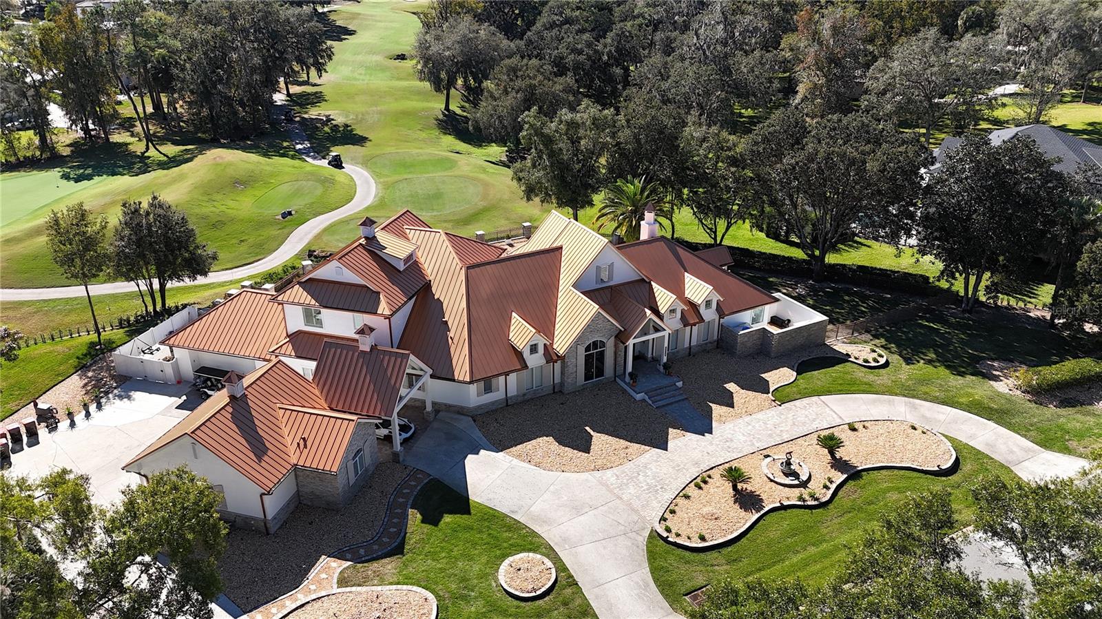Welcome to a breathtaking estate in the Country Club of Ocala, where timeless architecture, modern elegance, and resort-style living come together in perfect harmony. Nestled along the rolling fairways of a unique, manicured golf-course community, this striking residence commands attention with its copper-toned metal rooflines, stone accents, and grand presence- an estate as beautiful as it is unforgettable.
Inside, the home unfolds with soaring ceilings, abundant natural light, and sweeping golf views framed by dramatic floor-to-ceiling windows. The formal living room creates a showstopping first impression with its coffered ceilings, stately fireplace, and wide-open vistas that blur the line between indoors and out.
The gourmet kitchen is designed for both beauty and function, featuring rich custom cabinetry, a massive entertaining island, double ovens, and warm gathering spaces that flow effortlessly into the family and dining areas. Every detail speaks to quality craftsmanship and comfort.
This exceptional home offers 4 bedrooms and 5.5 baths, plus an office and a media room, ensuring ample space for both relaxation and productivity. A breezeway conveniently connects to the man cave, which includes a full bath and can easily be transformed into a mother-in-law suite, adding versatility to the layout.
Step outdoors to your private retreat—an expansive resort-style pool area surrounded by stone pavers, elegant fencing, and multiple lounging spaces. From sun-drenched patios to an inviting fire pit terrace, the setting offers unmatched views of the manicured greens and mature oaks that define the landscape. Outdoor living is elevated even further with a covered patio, upper-level terrace, and a full outdoor kitchen, ideal for hosting unforgettable gatherings.
Set within one of the area’s most desirable golf communities, this estate captures the essence of refined living—grand, welcoming, and effortlessly impressive. From sunrise over the fairways to evenings by the pool, this home offers a lifestyle of privacy, elegance, and year-round enjoyment.