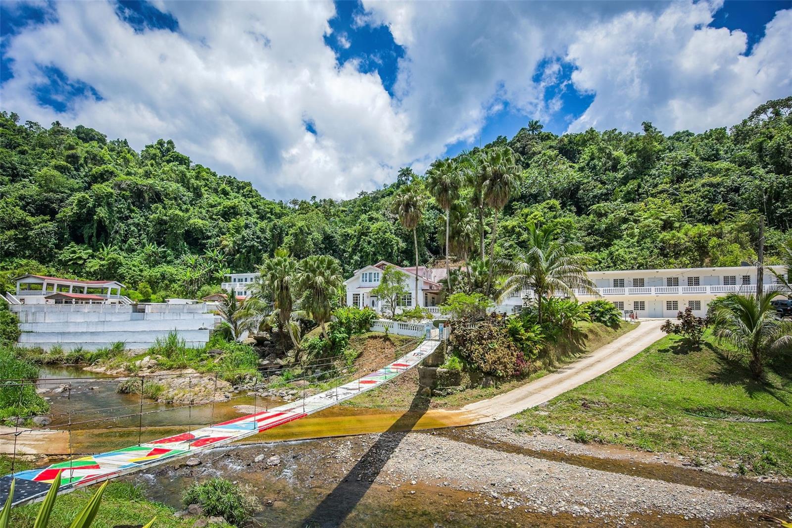 Discover an exceptional opportunity to own a one-of-a-kind mountain estate in the heart of Puerto Rico’s lush central highlands. Nestled within 23 acres of rolling terrain, this expansive property offers unmatched privacy, panoramic mountain views, and an atmosphere of pure tranquility, making it the ideal setting for a boutique wellness retreat, nature-inspired hospitality project, healing sanctuary, or an exclusive private estate.
 
Strategically located just 40 minutes from Ponce, one hour from Arecibo, and 90 minutes from San Juan, the estate provides the perfect balance of seclusion and accessibility. Guests and visitors will enjoy a peaceful escape without sacrificing proximity to major cities, airports, and coastal destinations.

Whether you envision a sanctuary for healing and reconnection, a private luxury compound, or an income-producing tourism venture, this property is uniquely positioned to support a visionary project that honors the natural surroundings and meets the growing demand for experiential travel.

The estate comprises five buildings, three of which are dedicated residential structures. At the heart of the property is a stunning two-story main house, beautifully crafted in wood and featuring multiple bedrooms, bathrooms, and a private kitchen. Two additional guest residences complement the main home, bringing the total to 19 fully furnished bedrooms thoughtfully distributed across the property. Collectively, the residential buildings are approximately 12,440 square feet of interior living space, providing ample accommodations ideal for retreats, family gatherings, or group getaways.

At the heart of the outdoor amenities lies a striking 35 ft. x 55 ft. swimming pool, with a capacity of roughly 100,000 gallons, perfectly positioned to capture breathtaking mountain views and the nearby river. Enhancing the poolside experience is a dedicated kitchen building designed for seamless outdoor dining and entertaining. Above, an open-concept balcony serves as a picturesque venue for events, offering elevated panoramic vistas of the surrounding landscape.

Recreation and wellness amenities include a separate building with a game room and a fully equipped gym, featuring 18 workout machines. An efficient commercial-grade kitchen is also on-site, ideal for hosting meals or catering events. In total, the square footage of all buildings—including residential, recreational, and amenity structures—exceeds 20,000 square feet.

The grounds are dotted with charming walking paths and footbridges that cross the river running through the estate. Nearby attractions include Lago Garzas, Bosque Estatal de Guilarte, and Cascada Las Garzas, placing you in close proximity to some of the island’s most scenic natural areas.

Additional property features include a 30KW backup generator, a 5K water cistern, and the inclusion of all furnishings, appliances, and fixtures, making this an expansive and well-equipped estate ready for immediate use.