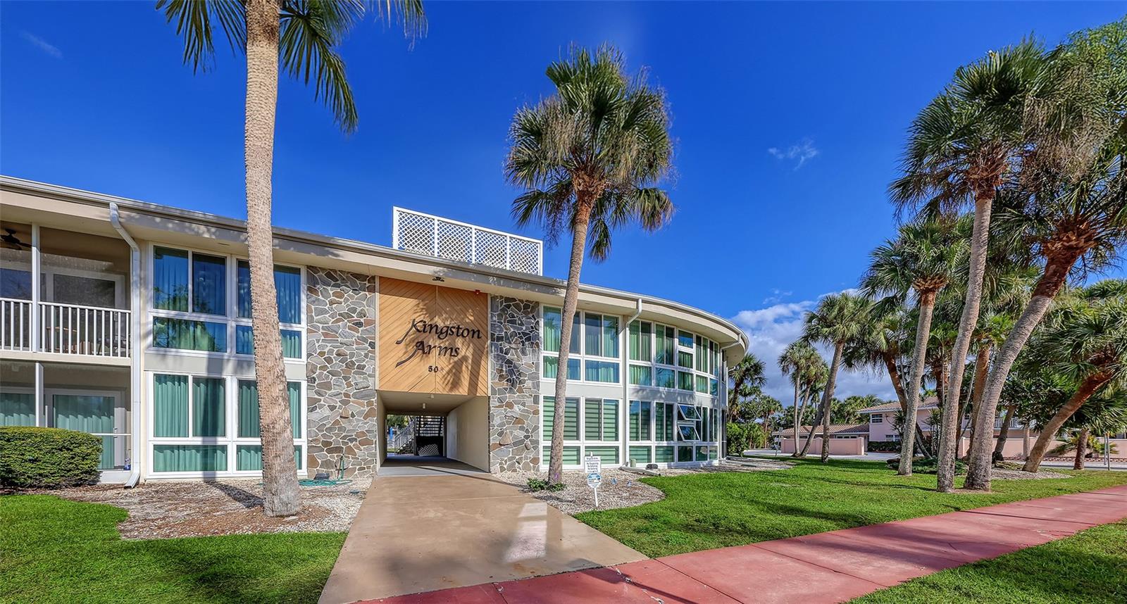 Whether your primary residence, second home, or investment property, this first-floor 2 bed/2 bath condo in Kingston Arms provides a walkable lifestyle second to none. This "hidden gem" is directly behind the shops, dining, and entertainment destinations found on St Armands Circle, and just a short walk to Lido Beach. Kingston Arms rarely has availability due to its amazing location. This fully renovated and turnkey furnished condo offers an open floor plan filled with light from the sliding doors opening to your private screened patio. The kitchen and 2 bathrooms have been beautifully updated with thoughtful finishes, including gorgeous new counters, cabinetry, appliances, and beautiful tiles in both showers. Custom blinds, fresh paint, modern floorboards, and large neutral tiles enhance each room. The primary suite is large enough for a king-size bed and features a walk-in closet, linen closet, and en-suite bathroom with step in shower. The guest bedroom has loads of closet space and an en-suite bath. Additional upgrades include new A/C and wi-fi thermostat, recessed LED lighting, and an interior laundry closet with full size washer/dryer. One covered parking space is included.  A small pet is allowed, as are one-month rentals, up to 12 times a year.