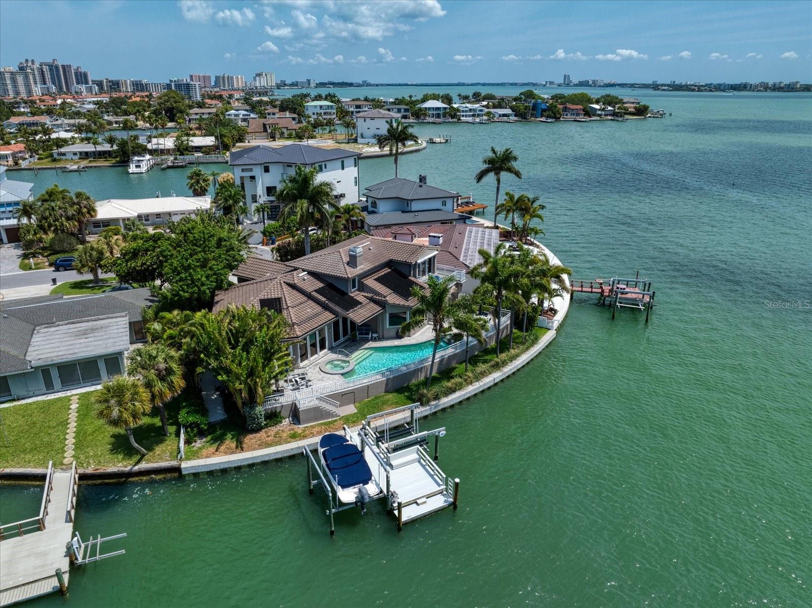 This beautiful waterfront property is ready to be your home in paradise. As you approach from Gulf Blvd to the cul-de-sac at the end of Donato Drive, you'll enjoy the lush tropical landscaping along the way which features elegant new solar-powered street lamps. All utility poles and lines in this part of Bellevue Estates were recently moved underground, making this street one of the most desirable in Belleair Beach. Situated at the end of Donato Drive, the property boasts a 120 foot seawall which was replaced in 2019, along with the new boat dock built in 2019 with composite decking and lifts which accommodate a 10k lb boat plus two jet skis (total 6k lbs.). When you enter the house you will pass through gorgeous art-glass double doors which open to a spacious foyer. And the water views start there. All rooms boast large windows and/or sliders; your enjoyment of the wide-water view is unimpeded. Classic hard wood floors flow throughout the home, connecting all rooms for a spacious feel. The living room is divided from the dining room by a sophisticated gas-burning fireplace and also has a dry bar with cabinets for your barware and serving pieces.  The large kitchen offers a Sub-Zero refrigerator, two dishwashers, a prep sink at the center island, three garbage disposals and a gas stove for the gourmet chef. There is also a substantial wine cellar with separate climate control to protect your wine collection. The primary suite has a lovely tray ceiling, wonderful water views and is located on the first floor for your comfort. Climb the staircase to the second floor, where you will find a family room/den. Both upstairs bedrooms feature en-suite baths, and there is access to a large balcony from one of the bedrooms. This home has two HVAC systems, new in 2022 and 2024, water heater in 2023, new dishwasher in 2022, tile roof was new in 2012, new pool pump 2024. Back on the ground level, you will love entertaining outdoors! The outdoor kitchen has a gas grill with commercial exhaust hood, plus there is a sink, cabinets and an ice-maker, recently installed. The pool and spa are solar heated. Enjoy spending time with your family and friends dining, swimming and boating! Dolphins frequently frolic near the seawall, putting on a show for onlookers. This wonderful home is waiting for you. Make your appointment to view it today.