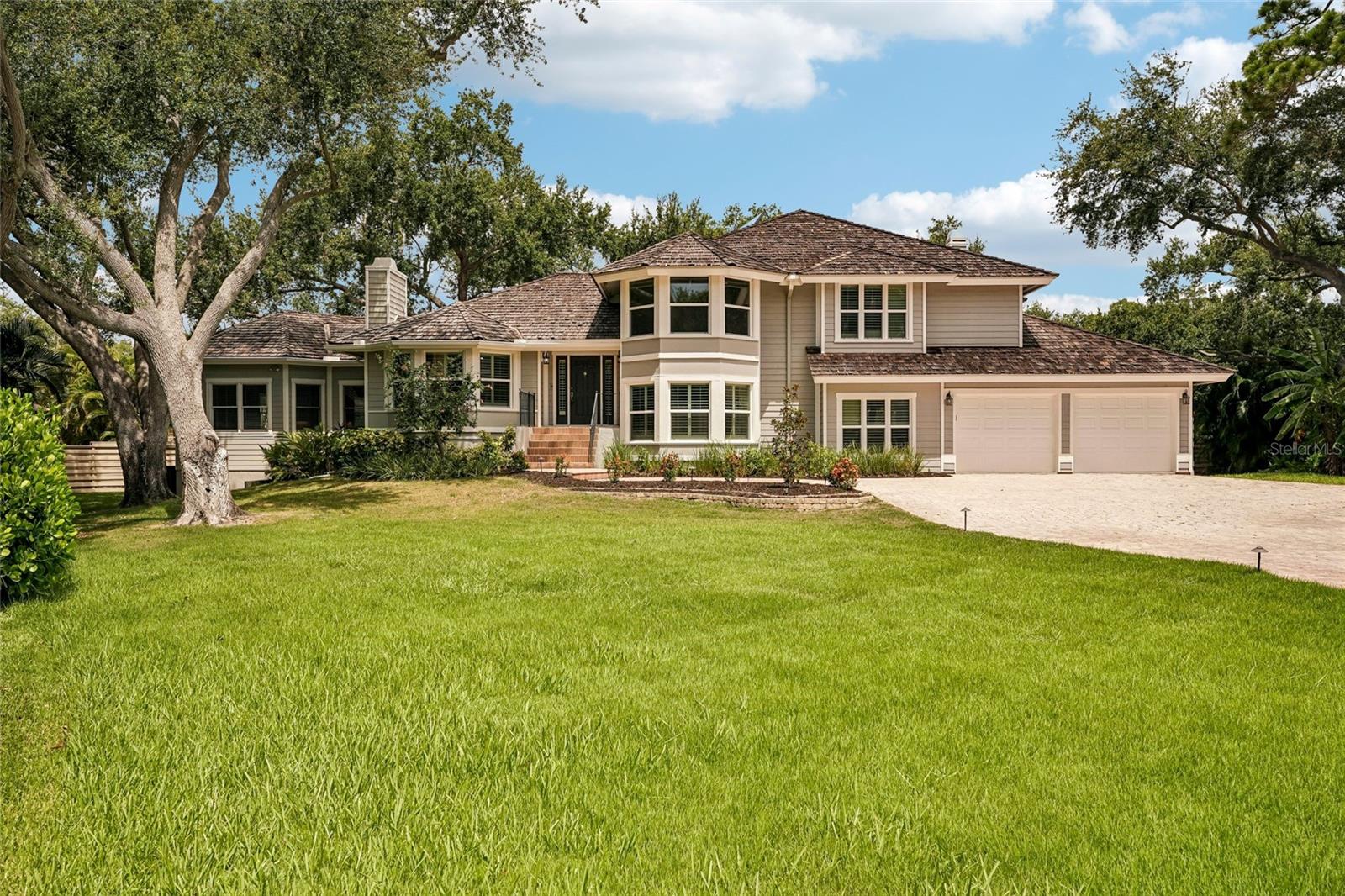 Virtually Staged. Tucked beneath a canopy of sweeping mature oaks in one of Sarasota's most coveted gated communities, this gracious two-story home strikes the perfect balance between timeless elegance and Florida ease. The brick paver driveway, bay window entry, and lush manicured lawn set an inviting first impression that the interior effortlessly sustains. Step inside to soaring vaulted ceilings with exposed beam detail, gleaming hardwood floors, and a stunning crystal chandelier that anchors the grand living room. A classic white marble fireplace, plantation shutters, and an open staircase with white balusters and rich wood railing give the space a warmth and architectural character rarely found at this price point. The kitchen is bright and functional — white cabinetry with glass-front uppers, an island with cooktop, double wall ovens, stainless steel appliances, and a picture window framing the lush greenery outside. A perfect canvas for the cook who wants both form and function. The screened pool and spa with brick paver deck and mature oak surround deliver complete privacy and the quintessential Florida outdoor lifestyle — whether you're entertaining or simply unwinding after a day at the beach. Located in The Landings, Sarasota's premier gated community known for its racquet sports complex, nature trails, and unbeatable proximity to Siesta Key Beach, top-rated dining, and the vibrant arts and culture scene downtown Sarasota is celebrated for.. Included 100-Day Home Warranty with buyer activation