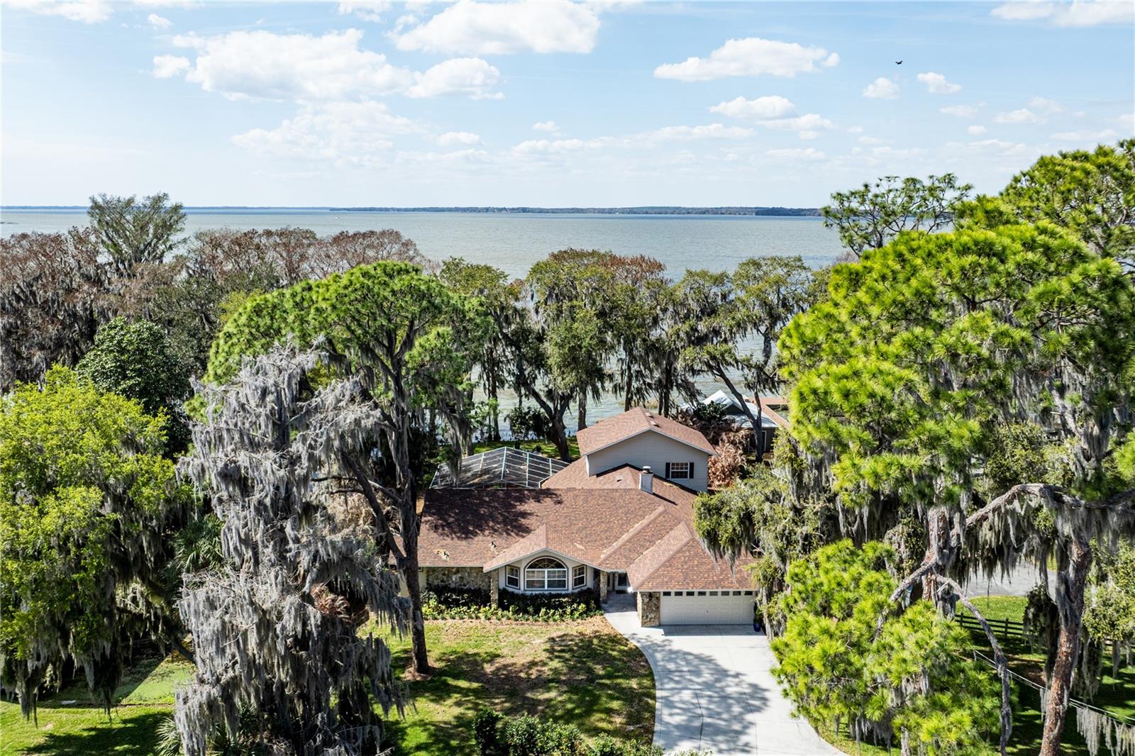 Available Again! Welcome to a rare opportunity to own a private waterfront retreat on the shores of Lake Harris, one of the many lakes that make up the highly sought-after Harris Chain of Lakes. Offering over 3,100+ square feet of living space, this beautifully updated 3-bedroom, 2-bath home is perfectly positioned on a .67-acre lot on a quiet dead-end road, delivering exceptional privacy and breathtaking lake views.

Located in unincorporated Lake County, you’ll enjoy the benefit of lower property taxes while still being just minutes from downtown Tavares, shopping, dining, and medical facilities.

Inside, the home has been extensively updated and thoughtfully designed. The fully renovated kitchen features granite countertops, updated appliances, custom backsplash, abundant cabinetry, and a spacious breakfast bar overlooking the living areas. New hickory hardwood floors run throughout the home, complemented by updated plumbing, luxury ceiling fans, and beautifully renovated bathrooms with new vanities and one-piece luxury toilets. A redesigned fireplace and mantel add warmth and character, while new windows, doors, and a panoramic glass frame that fill the home with natural light and stunning lake views.

The open-concept living area flows seamlessly to the outdoor space, where a large, screened pool enclosure opens to new paver patios, a custom paver firepit, and mature oak trees that create a park-like setting. The decorative stone façade and decorative concrete driveway (2021) provide outstanding curb appeal.

Upstairs, the spacious loft area is ideal for a home office, creative studio, or quiet reading retreat, offering flexibility to suit your lifestyle while overlooking the main living space.

For boating enthusiasts, the property features direct Lake Harris frontage along with a private canal leading to a covered boathouse equipped with a new lift and automatic boat cover. Enjoy year-round navigable access to the entire Harris Chain of Lakes — perfect for boating, fishing, waterfront dining, and sunset cruises right from your backyard.

Major improvements include a new roof (2021) and a three-zone HVAC system (2021), providing peace of mind for years to come.

This is more than a home ~  it’s a private Lake Harris lifestyle defined by space, sunsets, and endless waterfront possibilities. All information recorded in the MLS is intended to be accurate however, it should be independently verified by buyer and their agent.