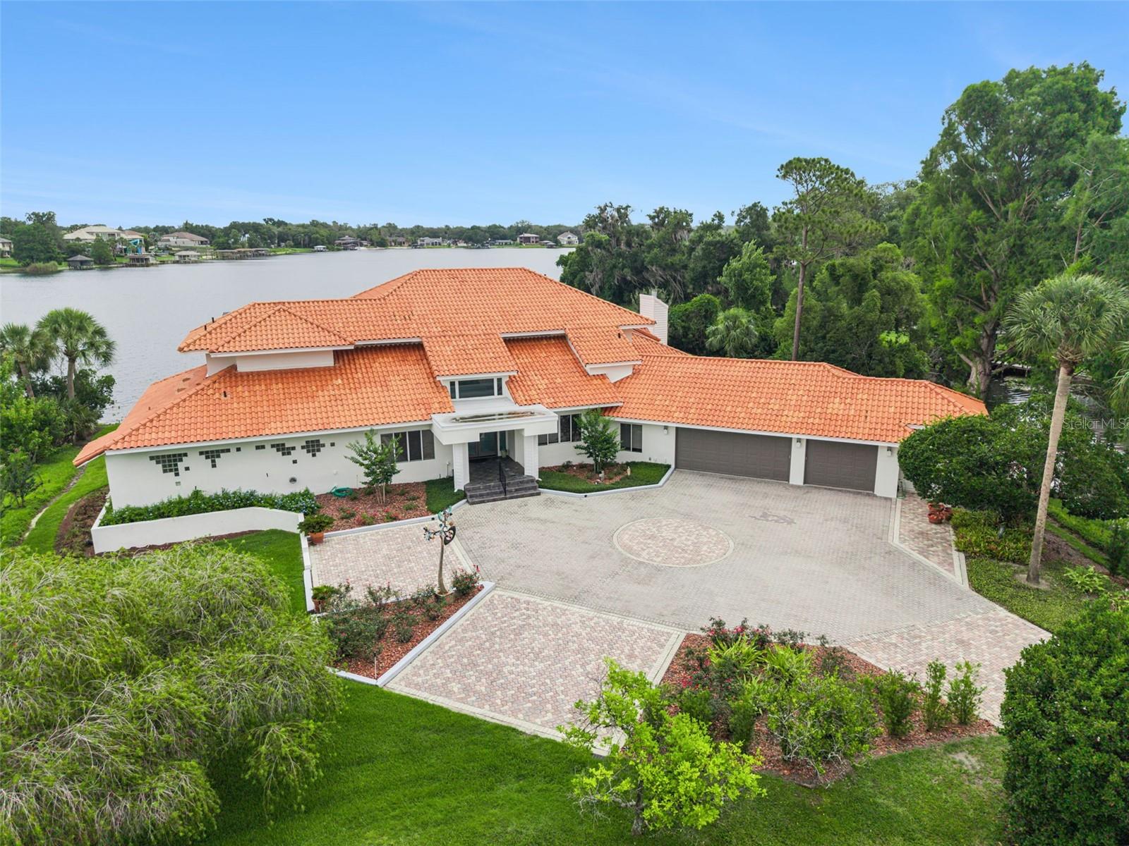 Available for the first time, this exceptional estate is set on a rare peninsula lot surrounded by Lake Brantley on three sides and offers a level of privacy, tranquility, and presence that is truly unmatched. A long, private paver drive winds past the community tennis court and leads to a striking residence featuring a newly painted exterior in a light, timeless tone that enhances its overall appeal. Inside, soaring ceilings and dramatic walls of glass immediately draw your eye to the expansive lake views beyond, with nearly every room oriented to capture the scenery and create a constant connection to the outdoors. The main level is designed for both refined entertaining and everyday living, featuring formal living and dining rooms, an expansive kitchen overlooking the family room, and a sunken gathering space that adds depth and architectural character to the heart of the home. The primary suite is a true retreat, privately positioned on the first floor with serene lake views, a sitting area, an oversized walk-in closet, and a beautifully renovated bath featuring a soaking tub, dual sink vanity, and an expansive walk-in shower. A dedicated office with double door entry and closet offers flexibility as a fifth bedroom. Upstairs, three additional bedrooms include two connected by a Jack and Jill bath, one with its own en-suite, along with a loft-style catwalk and gathering space overlooking the main living area and framing stunning views through the two-story windows. A spacious laundry room and large storage room are located just off the three-car garage, which features a rare pass-through bay with front and rear access ideal for boat storage, plus an additional flex space for a workshop, hobbies, crafts, or storage. The screened pool area is designed for true indoor-outdoor living, complete with a built-in bar, expansive seating areas, and uninterrupted panoramic lake views that create a resort-style experience. The private boathouse with lift and a waterside sitting area, perfect for relaxing or fishing complete the property, offering direct lake access and a lifestyle centered around the water. Ideally located in Longwood, this is a rare opportunity to own a property defined by its extraordinary setting and timeless appeal.