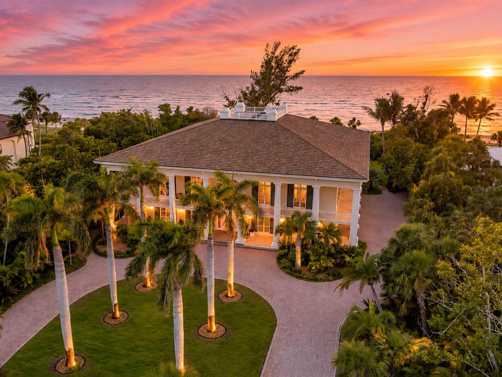 Positioned on a rare 1.97-acre Gulf-to-lagoon estate within the exclusive gates of The Sanderling Club, 8132 Sanderling Road offers one of the most extraordinary waterfront lifestyles on Siesta Key. Framed by lush tropical landscaping and introduced by a sweeping palm-lined drive and stately columned façade, this Christner Bros. built residence combines timeless architecture with exceptional privacy and direct access to both the Gulf of Mexico and Heron Lagoon. The home encompasses approximately 8,209 square feet of living space with 4 bedrooms, 4 full baths, 1 half bath, elevator access, a five-car collector's garage with workshop space, and expansive indoor and outdoor living areas designed for both grand entertaining and everyday comfort. Inside, soaring ceilings, extensive custom millwork, marble flooring, and a sweeping curved staircase create a dramatic sense of scale. The grand living and dining spaces are filled with natural light and open seamlessly to a spectacular 360-degree covered terrace, blending indoor and outdoor living while capturing panoramic views of the Gulf, Heron Lagoon, and the surrounding tropical landscape. The chef’s kitchen is thoughtfully designed for both daily living and entertaining, featuring custom cabinetry, granite countertops, a Wolf gas cooktop, Sub-Zero refrigeration, double wall ovens, generous prep areas, and direct terrace access. A richly appointed office with custom built-ins, an extensive butler’s pantry, media room, and oversized utility spaces further enhance the home's functionality and comfort. The private primary suite serves as a luxurious retreat with terrace access, generous sitting areas, and a spa-inspired bath featuring dual vanities, a walk-in shower, extensive cabinetry, and abundant natural light. Three additional guest suites provide comfortable accommodations for family and guests, each with en-suite baths and tranquil tropical views. The lower level offers tremendous flexibility with expansive bonus space ideal for a fitness center, golf simulator, game room, wellness retreat, workshop, or collector’s showcase. Automotive enthusiasts will appreciate the oversized five-car garage with additional workshop space and room for significant collections or hobbies. Additional features include impact-rated windows and doors, shutters and screens, a security system, and a newer 24-kW Kohler generator. Beyond the residence, the property's Gulf-to-lagoon setting is exceptionally rare. With approximately 150 feet on the beach and 150 feet of Heron Lagoon frontage, the property offers a truly rare combination of beachfront living and protected waterfront recreation. Launch a kayak or paddleboard from the private dock, enjoy breathtaking sunsets over the Gulf, or take advantage of The Sanderling Club's  marina, tennis courts, clubhouse, and unmatched privacy. Just beyond the gates, Siesta Key's world-famous quartz sand beaches, Siesta Village, waterfront dining, boutique shopping, and vibrant Sarasota arts and culture create an unparalleled coastal lifestyle. Consistently recognized among the nation's top beaches by TripAdvisor and U.S. News & World Report, Siesta Key remains one of Florida's most sought-after waterfront destinations. 8132 Sanderling Road is more than a home, it's a legacy Gulf-front estate offering exceptional privacy, architectural distinction, and one of the rarest waterfront settings on Florida's Gulf Coast.