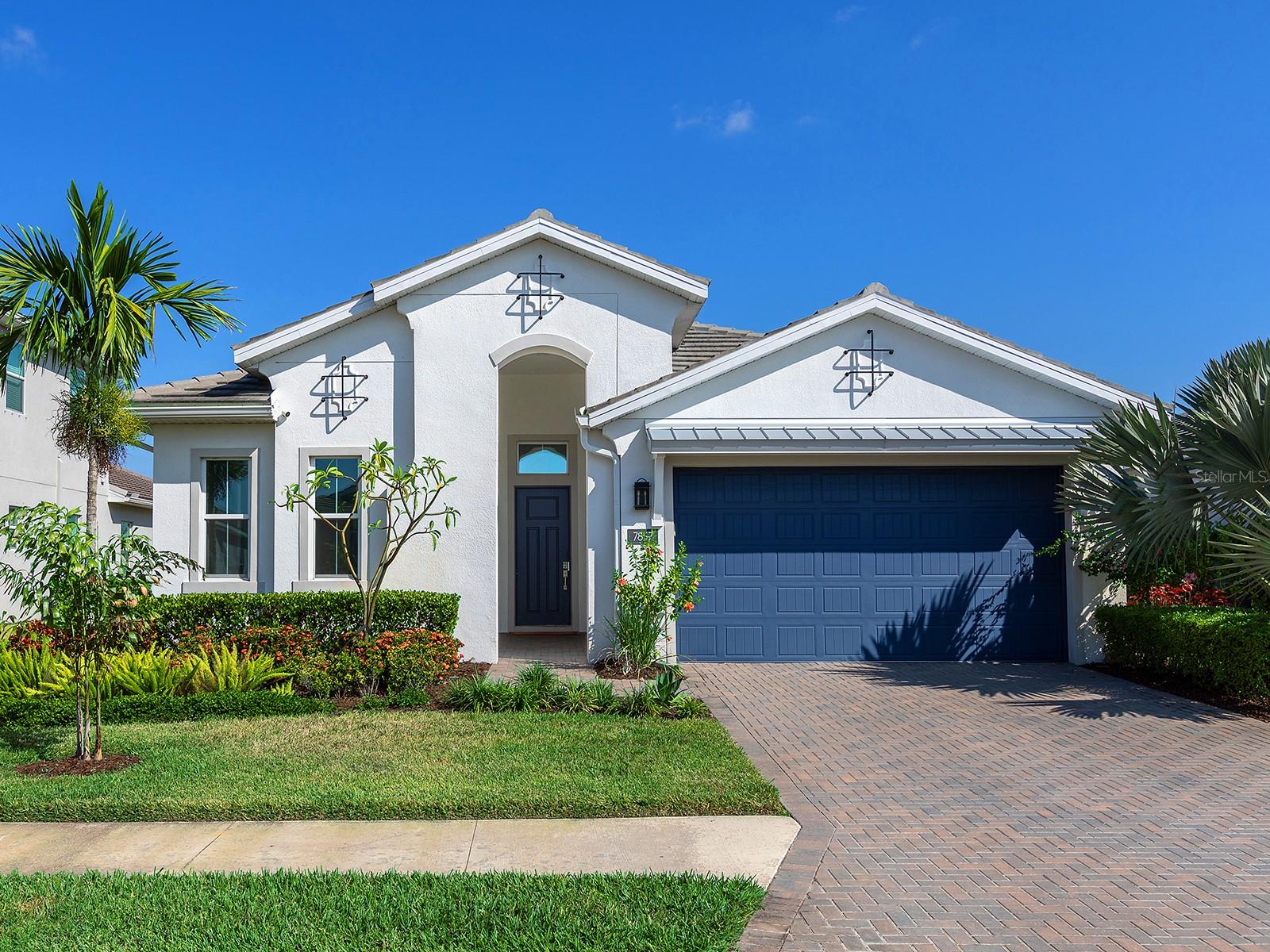 Experience modern coastal living in the Isles, where this light-filled retreat offers refined interiors, effortless flow, and peaceful views of the surrounding lake and preserve. Stepping onto the paver driveway, the home’s crisp white façade immediately sets a modern coastal tone, with clean architectural lines, lush tropical landscaping, and a striking blue front door that hints at the thoughtful design inside. Built in 2021, this 3-bedroom home with an office spans 2,292 square feet of refined living space, offering partial lake views and a seamless indoor–outdoor lifestyle. A covered entry leads into the foyer, where high ceilings and luxury vinyl flooring establish the home’s bright, airy character. The wide hallway draws the eye straight toward the great room. The spacious great room reveals a tray ceiling and recessed lights enhance the sense of scale. Large sliding glass doors line the back wall, pulling in views of the preserve and drawing the outdoors inward. The great room opens directly into the kitchen, creating an easy, connected gathering space. The kitchen centers around a large marble-style island with a farmhouse sink and an industrial spring faucet, complemented by black shaker cabinetry with gold hardware, a white subway tile backsplash, and under-cabinet lighting. Three pendant fixtures provide added warmth, while a KitchenAid wall oven and microwave, Whirlpool cooktop, stainless refrigerator, range hood, and integrated dishwasher complete the polished, functional layout. Adjacent to the kitchen, the dining area is brightened by two large windows and a pendant light, with nearby sliding doors offering seamless access to the lanai. The office provides a quiet retreat with its chandelier lighting and warm natural light. Nearby, the half bath continues the bold blue palette with a pedestal sink, chrome fixtures, and a framed mirror, all clean, simple, and modern.  The primary suite is set in its own wing, an airy, serene retreat with a tray ceiling, ceiling fan, and multiple windows framing the greenery outside. Two walk-in closets with built-in wood shelving add impressive storage, and the en-suite bath delivers a spa-like feel with dual vanities, granite countertops with a dedicated makeup area, a large walk-in shower with frameless glass, and a soaking tub. A private water closet completes the space. Two guest bedrooms on the opposite side of the home offer soft carpeting, wall closets, and abundant natural light, sharing a full bath with a granite-topped vanity, chrome fixtures, tile flooring, and a tub/shower with sliding glass doors and a transom window. Outside, the paver lanai offers an extension of the living space with a ceiling fan and room for seating or dining, all overlooking a preserve and glimpses of the lake beyond. Practical features include a laundry room with cabinetry, granite countertops, sink, upper shelving, and washer/dryer, plus a two-car garage with epoxy flooring. Thoughtfully finished, beautifully maintained, and designed for modern coastal living, this home invites you to walk in, exhale, and feel immediately at ease. The Isles at Lakewood Ranch offers a resort-style pool, clubhouse, fitness center, tennis, pickleball, basketball, a fishing pond and dog park. Minutes from UTC, Waterside Place, downtown Lakewood Ranch, Sarasota, Gulf beaches, Mote Aquarium, Benderson Park, and the Sarasota Polo Fields, this home blends modern elegance and effortless Florida living.