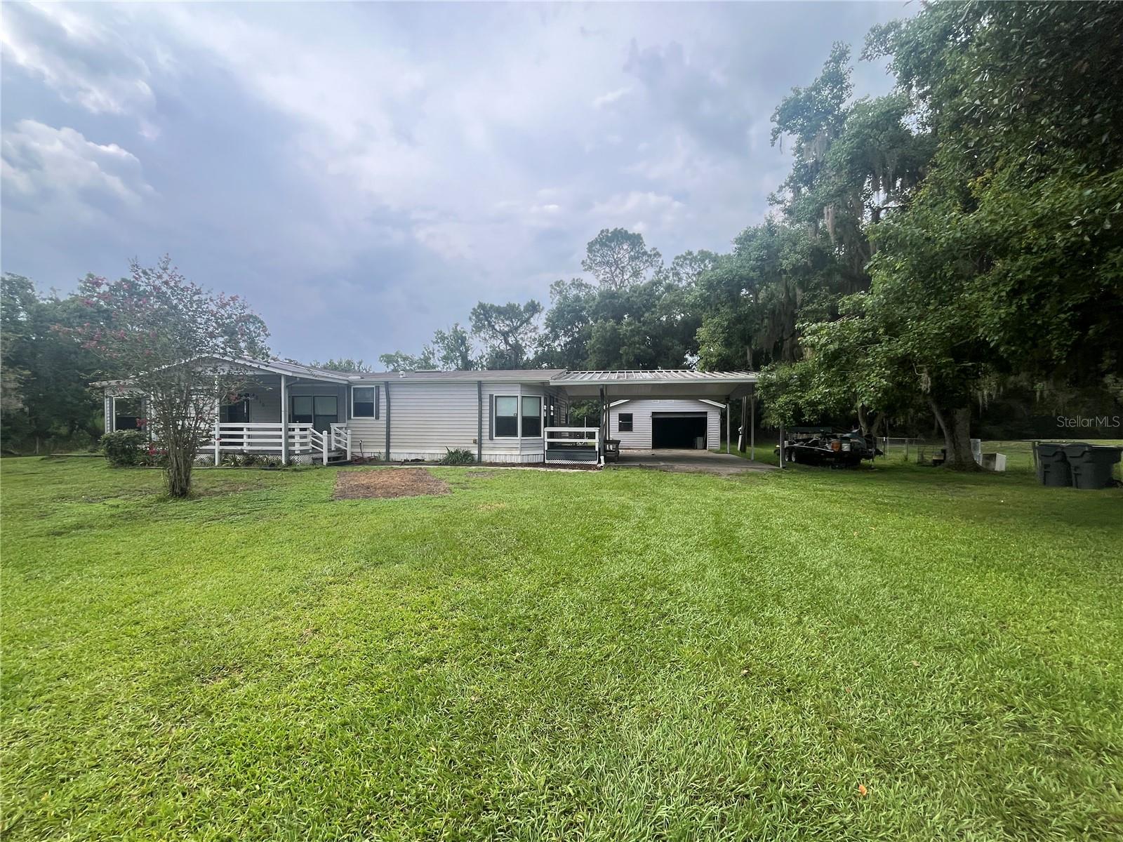 Spacious 1.65-Acre Corner Lot with Endless Potential! Discover the perfect blend of country privacy and practical living on this massive 1.65-acre corner lot. Situated on a quiet, peaceful street, this well-loved and cared-for property offers an incredible foundation for its next owner. Roof installed in 2023. A/C replaced in 2018. Water Heater installed in 2017. Connected to county water and on a septic tank system. Massive carport, 24x26 double carport provides ample covered parking and shade. Detached one-car garage and workshop, perfect for hobbies, tools, or extra storage. Enjoy your morning coffee on either the front or side deck patios. Chain-link fenced in yard, ideal for pets, gardening, or secure play. Inside, you will find a home that has been deeply cared for over the years. Very spacious 1568 sq.ft. living area under roof. The property is being sold As-Is, with some select furniture remaining for your convenience. While it needs new flooring throughout, this is your golden opportunity to choose your own styles, build instant equity, and customize the space exactly to your liking. Don't miss out on this rare acreage opportunity—schedule your viewing today!