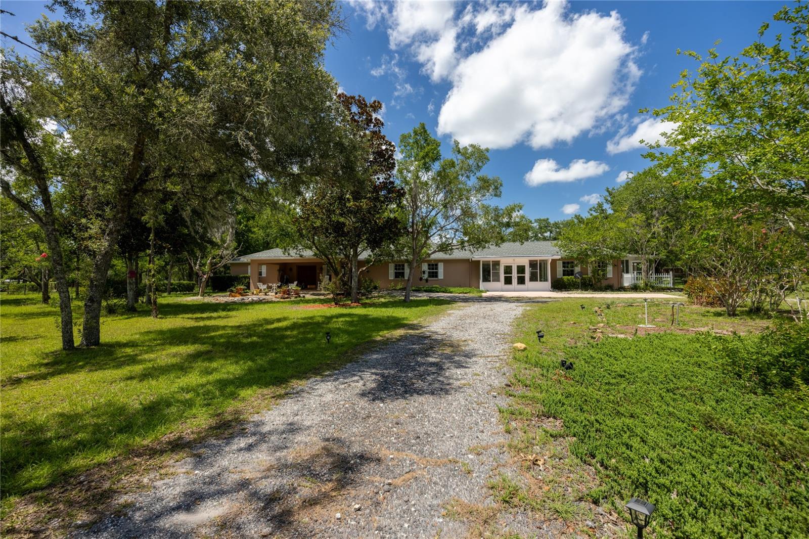 Welcome to Your Dream Horse Farm! Step into this remarkable custom estate, a sprawling 5-bedroom, 4-bath masterpiece with 3,315 square feet of living space. Set on an expansive 10-acre parcel of high and dry pasture land in the charming Steeplechase Farms, this property is a true paradise for horse lovers. With easy access to scenic horse trails and carriage routes that lead directly to Black Prong Equestrian Village and Goethe State Forest, you have the rare opportunity to immerse yourself in the equestrian lifestyle. Ideally positioned between Gainesville and Ocala, you are also just moments away from the exhilarating World Equestrian Center and HITS. Prepare to be amazed by the spacious open split floor plan framed by impressive 10-foot ceilings. As you step into the welcoming foyer, you’ll find a formal dining room and a cozy living room flooded with natural light, both showcasing a stunning stone wall and a charming wood-burning fireplace. The eat-in kitchen is a delight, featuring abundant cabinet space, a breakfast nook, and a bar counter overlooking the great room, allowing you to engage with family and friends while you whip up culinary creations. Indulge in the luxury of two master suites, each offering its own private bath, serving as a serene retreat. The first suite boasts a versatile room, perfect for an office or lounging area, along with two generous walk-in closets, one outfitted with custom shelving. Enjoy the meticulous design of the step-in shower, the luxurious jetted jacuzzi tub, and the elegant dual-sink vanities. The second primary suite includes a full bath and a charming studio with a glass front, perfect for inspiration. The home is tastefully tiled and features a convenient vacuum system. Guests will feel right at home in the living quarters, featuring 1 bedroom, 1 bath, a kitchenette, a cozy dinette, and an attached sunroom. Unwind in the expansive Lanai/Florida Room, where stunning views of vibrant White Stone Rock Gardens await, adorned with lush, colorful landscaping. Experience tranquility as you relax under the stars with three brand new skylights. Revel in the beauty of nature, with birds, butterflies, and fish around you, all while listening to the soothing sounds of the Koi pond's cascading waterfall, surrounded by picturesque canna lilies and flowers. The property boasts an impressive barn with two pole barns, totaling 10 stalls, along with two tack rooms and six run-outs that lead to rolling pastures. Explore the seven paddocks and a beautiful acre nestled between the barns, featuring majestic magnolia and juniper trees, plus a chicken coop. The perimeter is securely fenced, with electric controls in two paddocks, ensuring your animals safety. This property is equipped with a host of additional features, including a brand new generator with a Reliance Pro/Tran electric switch that delivers 7,250 to 9,000 watts throughout the estate, a spacious storage shed, an irrigation sprinkler system, and individual A/C units and water heaters. Recent enhancements include a new roof (2021), a new range and dishwasher (2021), new skylights (2021), and fresh paint (2021). Best of all, there are no HOA fees and no flood zone worries—just pure bliss awaiting you at your ideal horse farm!