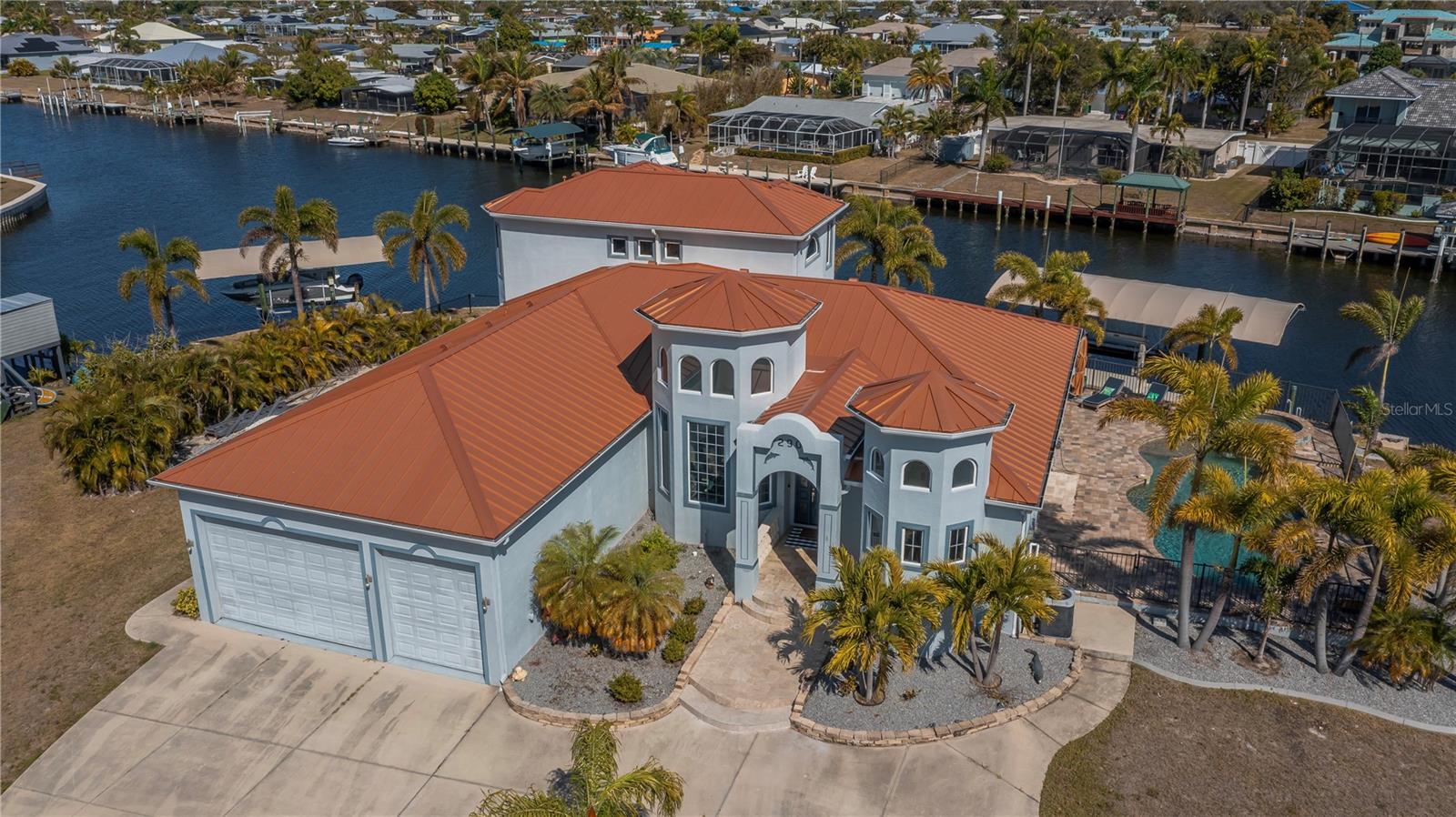 Experience the PINNACLE OF WATERFRONT LUXURY at 290 Tait Terrace, an EXQUISITE EXECUTIVE RESIDENCE set on a ILLUSTRIOUS 260 FT TIP LOT offering panoramic harbor vistas and quick SAILBOAT to the harbor and Gulf. Built with CONCRETE BLOCK TOP TO BOTTOM & ELEVATED at 12FT this custom 2008 4-BEDROOM 4-BATH 3-CAR GARAGE masterpiece accompanies refined open-concept living, graced by soaring 22-foot ceilings, custom crafted arched wooden front door, exceptional chihuly style glass chandeliers, elegant tray ceilings, stunning marble-like tiled floors and cathedral sunburst windows that flood every room with natural light and invite gentle cross breezes throughout. The open-concept office is a sophisticated serene workspace, thoughtfully designed with crown molding & coastal shiplap accents plus expansive desk areas, bathed in natural light from large windows/ soaring ceiling overlooking the grand foyer and circular driveway. This quiet retreat is perfect for focused work/ study while staying connected to the beauty outside.The den offers a cozy, versatile space for relaxation, reading, or a media lounge, providing additional privacy and comfort with sliders to the outside terrace/ pool w dimensional saltwater views. The oversized family room serves as the heart of the home, featuring a seamless flow to the adjoining spaces, highlighted by expansive glass doors that open to the terrace, creating an ideal setting for both intimate family moments and lively entertaining. Dining is an elegant affair here, whether enjoying a casual meal or hosting grand celebrations distinguished by its exquisite lighting and stunning views, while the adjacent gourmet chef’s kitchen features 2 SPECTACULAR BREAKFAST BARS. 
The gourmet chef’s kitchen is a work of art, showcasing granite countertops, premium stainless steel appliances, crafted wood cabinetry w meticulous attention to detail & perfectly positioned walk in pantry/butler closet.Retreat to the lavish master suite, a sanctuary w breathtaking saltwater views, coffered ceiling, plantation shutters, dual walk-in closets, w private pool & patio access. The spa-inspired ensuite indulges with a soaring 22-foot spa shower featuring resort style rain shower heads and bespoke fixtures, a jetted tub, & dual vanities crafted for luxury and comfort. The thoughtful split floor plan offers 2 generously sized guest suites on the main floor, while an impressive 4th bed Primary suite on the second floor boasts sweeping waterfront views & access to a private European-inspired balcony — the perfect vantage point for serene mornings & breathtaking evenings, complete with an elegant ensuite bathroom.
Outdoor living is an entertainer’s dream with a paver lined heated pool with separate spa, multiple terraces for lounging and dining, and two private docks with 2 covered boat lifts (Fishing Boat & Yacht) for effortless gulf access. Savor spectacular sunsets that paint the sky in vivid hues! Additional highlights include 2026 seawall being installed for full 260 ft, 2024 dual-zone A/C system, 2014 STANDING SEAM 100 YR METAL ROOF, NEW SEAWALL INSTALLED 2026, hurricane window, no HOA, public water/ sewer, & underground utilities — every detail designed for luxurious waterfront living. Ideally located near Port Charlotte Beach, historic Punta Gorda, Sunseeker Resort, vibrant dining, festivals, & the airport. Don’t miss your chance to own this extraordinary waterfront estate. Schedule your private tour today and step into your dream.