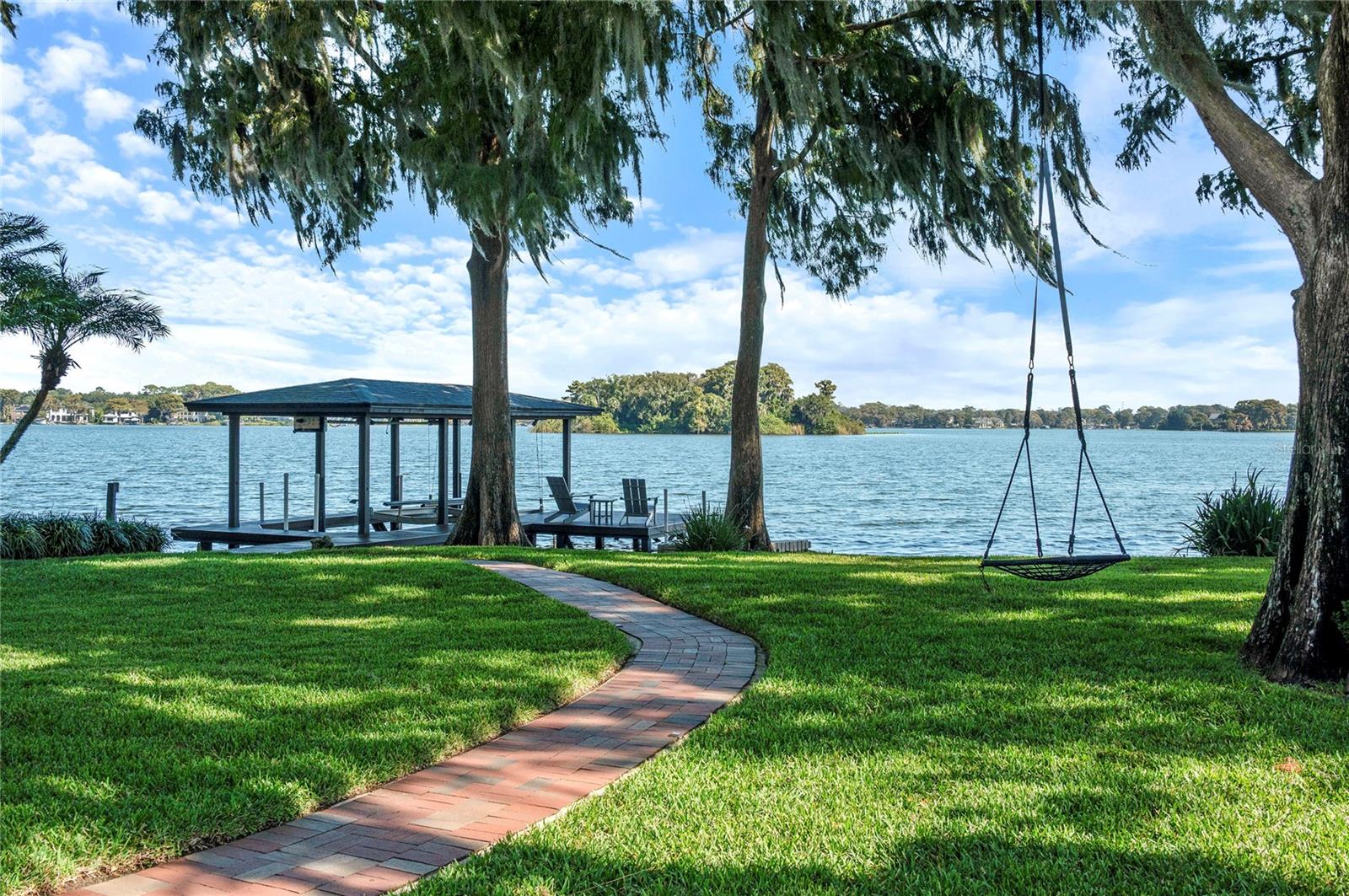 Tucked away on a quiet and beautiful Lake Maitland lot in the highly desirable Green Oaks neighborhood, this stunning French Provincial residence offers magnificent water views from nearly every room. With one of the most private entrances and lots in all of Winter Park, this timeless home blends European charm with modern comfort. The light-filled, open floor plan features a downstairs primary suite and a gorgeous family room with gas fireplace, opening to the pool and lake. The gourmet kitchen, also facing the backyard, is the heart of the home. Featuring granite countertops, light cabinetry and gas cooktop. The open layout includes the eat-in breakfast area and family room. Multiple French doors to the pool and lakefront for everyday indoor-outdoor living and enjoy breathtaking views that make every moment feel like a getaway. Upstairs, two generously sized bedrooms-each with en-suite baths are joined by a cozy conversation area with lake views, a large bonus room and a private office/study that could easily be an additional bedroom. A connecting guesthouse offers a true retreat with two bedrooms, a full bath, living area and kitchen, perfect for hosting friends or family. Sparkling pool, lush landscaping, and private dock on Lake Maitland, enjoy awe-inspiring sunrise views over the Isle of Sicily. Craftsmanship is showcased throughout, from the millwork to the 4-car garage, with extensive updates: roof (2021), multiple A/C systems with UV lights (2020–2025), new flooring throughout downstairs and all bedrooms (2020), updated upstairs windows (2020), rebuilt balcony with Trex decking, new pool equipment (2020) and pool converted to salt (filter 2024), Generac whole-house generator, Trex deck and dock with new cables and 7,500-lb lift (2022), new primary, upstairs guest suites and powder baths (2025), marble porcelain fireplace surround, remote shades in the primary suite, and new lighting fixtures throughout. Surrounded by manicured grounds and minutes from downtown Winter Park, Park Avenue shopping and restaurants, Enzian Theater, library, bike paths, and top-rated schools, (Dommerich, Maitland Middle and Winter Park High School). Just around the corner from Park Maitland and near Lake Highland and Trinity Preparatory Schools. This lakeside masterpiece offers unmatched privacy, luxury, and timeless sophistication-a truly exceptional home. Ski, wakeboard, pontoon or cruise around Dog Island and Isle of Sicily on the chain of lakes. Enjoy the magic of the holiday season- festive boat parade and holiday light displays. 121 ft of lakefront on the Winter Park Chain of Lakes.