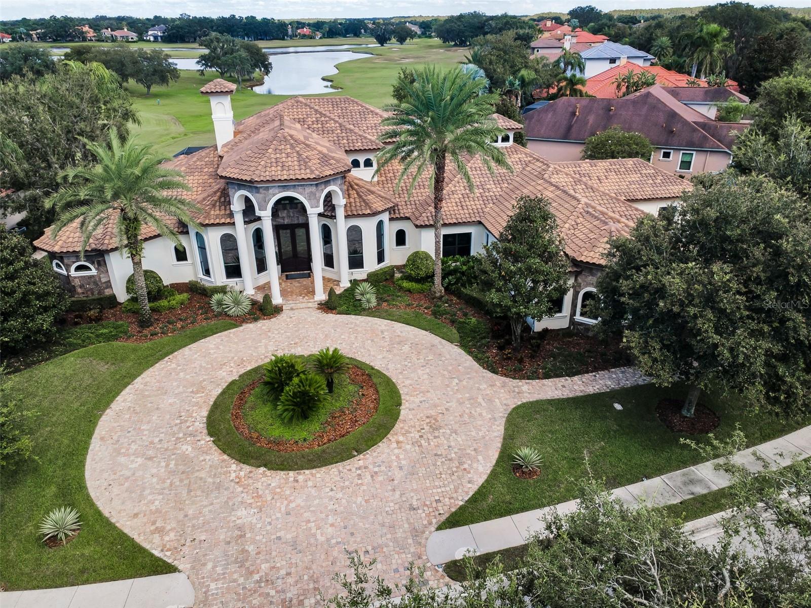 Located in the prestigious gated community of Florencia at the Champion’s Club in Trinity FL, this one-of-a-kind custom estate is set on one of the largest and most desirable lots, offering panoramic views of the lake and the 2nd hole of the renowned Fox Hollow Golf Club. Boasting 5,965 SF of living space and 9,100 total SF, this exquisite residence offers 6 bedrooms and 7 full bathrooms, including a separate 1 bedroom, 1 bath guesthouse. Designed for luxury living and grand entertaining, the home welcomes you with soaring 26-foot ceilings, a dramatic circular staircase, and stunning views of the golf course, water, and resort-style outdoor living area. The expansive layout features a three-way split floor plan, providing exceptional privacy throughout. The oversized primary suite is a private retreat with direct pool access, dual walk-in closets, a double-sided walk-in shower, and a centerpiece soaking tub. The gourmet kitchen is a chef’s dream, featuring high-end appliances, custom cabinetry, designer backsplash, and a large central island that opens seamlessly to the family room and game room, all with unobstructed views of the outdoor oasis. The outdoor living space is truly exceptional, highlighted by a sparkling pool with a large spill-over spa, a fully equipped summer kitchen, cozy fireplace, three distinct lounge areas, and a dining space perfect for entertaining. The detached guest casita is located just off the pool and outdoor kitchen, ideal for visitors or extended family. Additional features include a private office with custom built-ins, bonus/media room, exercise room, and a dedicated study or flex area. A circular paver driveway and lush landscaping complete the impressive curb appeal. This luxury community offers convenient access to top-rated schools, shopping, dining, hospitals, nearby beaches, and the Suncoast Parkway, and just 30 minutes from Tampa International Airport. Residents enjoy exclusive access to Champion’s Club amenities, including a resort-style pool and spa, clubhouse with catering kitchen, tennis and basketball courts, fitness center, and a calendar of resident-only events. This custom-built masterpiece offers an unmatched blend of luxury, privacy, and lifestyle in a secure, amenity-rich setting. Schedule your showing today.