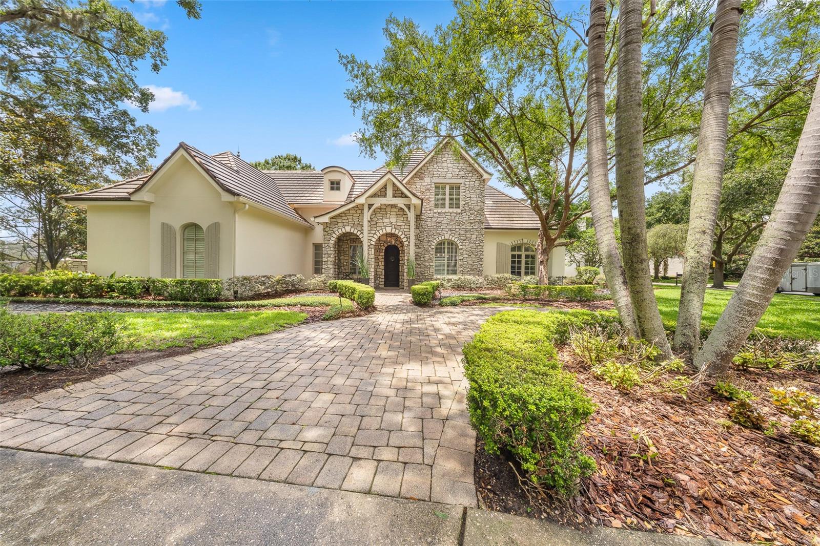 Tucked within the prestigious enclave of Windsong Lakeside in Winter Park, this extraordinary estate is a masterclass in refined living—where thoughtful design, cutting-edge technology, and timeless elegance converge. From the moment you arrive, the circular drive and stately presence set a tone of quiet grandeur. Step inside, and the home unfolds with an effortless sense of scale, defined by soaring vaulted ceilings and an abundance of natural light filtering through custom windows. Every detail has been meticulously curated—from the rich new flooring installed in 2025 to the soft glow of Currey & Co. lighting that adds warmth and sophistication to each space. Designed for both comfort and control, the residence is fully integrated with a wireless home automation system, allowing seamless management of lighting, climate, security, and more. Three A/C units ensure optimal comfort, while a new tankless water heater, water softener, and whole-home surround sound system elevate everyday living. A comprehensive security camera system and ADT Home Control provide peace of mind with modern convenience. Each of the four bedrooms is a private sanctuary, complete with its own en-suite bath, offering an elevated sense of privacy for residents and guests alike. The primary suite is a retreat unto itself, featuring custom built-in storage and electric storm shutters with blackout capability. The spa-inspired primary bath showcases a dual Grohe shower system, thermostatic auto tub filler and integrated TV - creating an environment of indulgence and serenity. At the heart of the home lies a newly renovated (2025) chef’s kitchen—an exquisite blend of form and function. Outfitted with premier appliances including a Wolf six-burner gas range, Sub-Zero refrigerator, Monogram built-in microwave, and dual dishwashers, the space is designed for both intimate meals and grand entertaining. Custom cabinetry with integrated lift features, dual sinks, filtered water dispenser, and elegant stone countertops complete this culinary haven. The living room invites relaxation with its newly renovated gas fireplace (2025), while a dedicated office offers bespoke built-in cabinetry with marble surfaces and glass shelving—ideal for sophisticated work-from-home living. Upstairs, the home transforms into an entertainment destination, complete with a projector theatre setup, wet bar, additional powder bath, and extensive storage. A dedicated A/V closet and the potential for an upstairs laundry add both function and flexibility. Outdoors, a private resort-style oasis awaits. The backyard has been completely reimagined, featuring lush turf, a sun deck platform, and even an in-ground trampoline—blending luxury with playfulness. The saltwater pool and spa, enhanced with upgraded LED lighting and a new heater (2025), were fully refinished and redesigned in 2021 to create a serene and visually stunning escape. A fully equipped summer kitchen—complete with a built-in gas grill, dual burners, refrigerator, and screened enclosure—sets the stage for unforgettable gatherings under the Florida sky. The three-car garage is equally impressive, featuring a Wallbox Level 2 electric vehicle charger (2023), seamlessly blending luxury with modern sustainability. This is more than a home—it is a statement of lifestyle, craftsmanship, and elevated living in one of Central Florida’s most sought-after lakefront communities.