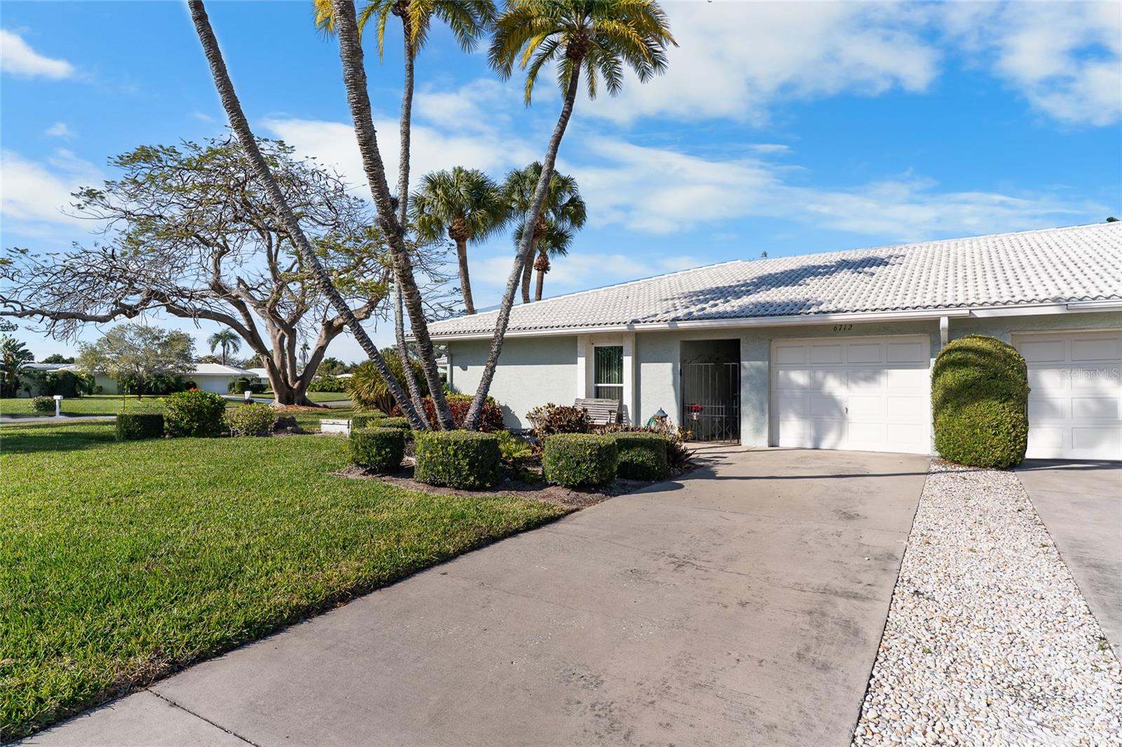 This home has an outstanding location situated on a corner lot with a spacious yard under the grand Royal Poinciana tree all maintained by the association.  Enjoy gorgeous sunset views with the gulf breezes coming from Palma Sola bay a few blocks away. Entering the home, notice the easy flow from the updated kitchen with a breakfast nook to the living area, including a formal dining area and end up in the bright and cheerful sunroom where enjoying morning coffee or a favorite evening beverage is a must. The large primary suite sits far away from the living area for privacy and includes an en-suite bath with updated walk-in shower. There is a sizable second bedroom and bath with a tub. The laundry/mud room has lots of space for storage or simple laundry tasks and the previous owner installed a clever storage area to use as your “basement”. Have the peace of mind that IMPACT WINDOWS are installed and that you are located in FLOOD ZONE X.  Village Green offers comfortable maintenance free living with a swimming pool, located behind the home on the “green”. A few minutes’ drive can get you to Bradenton Beach on Cortez or Anna Maria Island via Manatee Avenue. Blake Medical Center is close by and there is access to shopping galore. Sarasota, Tampa and St. Pete Airports are all a short distance away.