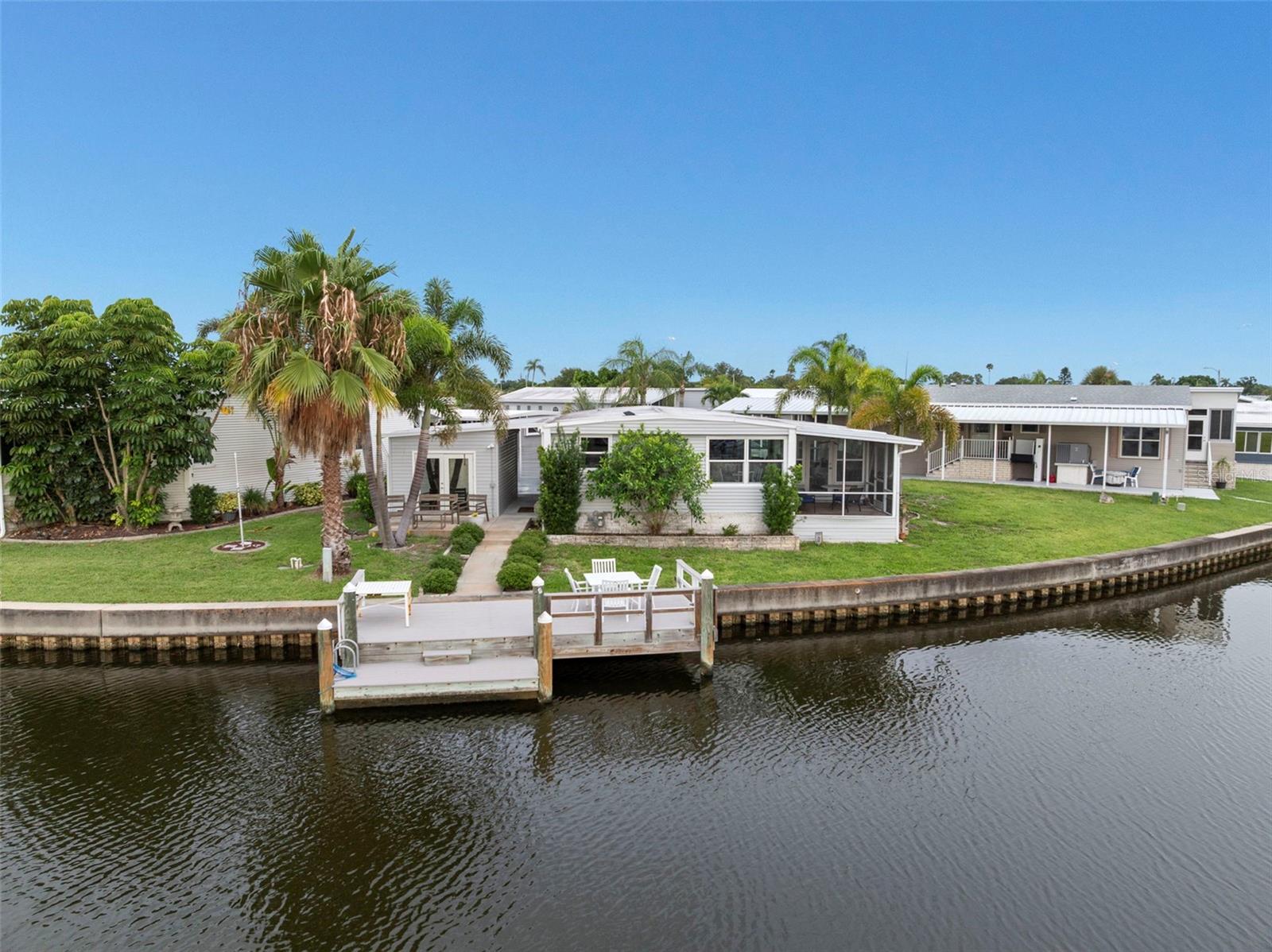 For the discerning buyer who appreciates beautiful views and a move-in ready home for a competitive price! With more than 1,400 sq. ft of living space, this 2 bed/2 bath home has a spacious lot with sweeping views of the water. Composite dock (10 x 12) built in 2017 with room for a lift, large shed with glass doors built in 2018 and two-vehicle carport are included in price. The home was lovingly remodeled over the past 5 years and includes: 1) chef's kitchen with large island, quartz countertops, stainless appliances including gas stove and wine fridge and new cabinets; 2) Open floor plan incorporates living/dining and Florida room creating a great entertainment space; 3) Easy-care laminate flooring throughout with ceramic tile in baths; 4) drywall throughout except in guest bedroom and beadboard motif in primary bedroom; 5) Washer and dryer in utility closet for ease of use; 6) Newer 2016 windows with custom shutters in bedrooms and living room; 7) HVAC system is 2025; 8) Roofover is 2015; Remodeled baths has walk in shower in primary and tub/shower combo in spacious guest bath. Comes tastefully furnished and decorated. Low monthly maintenance fee of $410 includes water, sewer, trash pick up, lawn mowing, 24 hr manned gate, clubhouse, heated pool, fitness center, billiards, two private boat ramps and kayak launch and seawall maintenance--a big benefit when living on the water! Home is located in popular 55+ Americana Cove, a prestigious factory-built housing community located only 10 mins to downtown St. Petersburg, 20 mins to two airports and 3 mins to 4th Street shopping, dining and grocery. Make this home your full-time residence, winter retreat or investment property as renting is allowed with 2-month minimum. 2 pets (dogs or cats) up to 35 pounds each are welcomed! This is a don't miss retirement property!