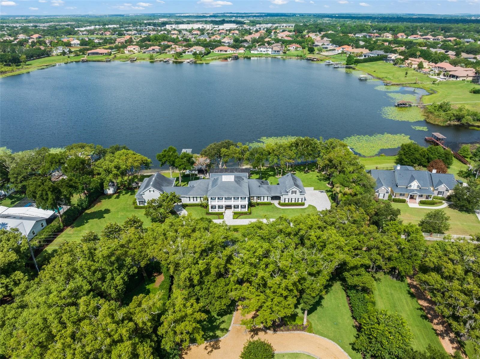 Experience the pinnacle of lakefront luxury breathtaking acres in the heart of Windermere, offering an extraordinary 320 feet of pristine ski lake frontage and an unmatched resort-style lifestyle. This one-of-a-kind waterfront compound features a stunning 6-bedroom, 5-bathroom main residence encompassing 12,323 gross square feet with 7,000 heated square feet, thoughtfully designed to maximize comfort, elegance, and breathtaking water views from nearly every angle. Adding to the property’s exceptional versatility is a private 2-bedroom, 1-bathroom guest house and separate garage apartment, creating incredible multigenerational living potential or the ideal setup for extended guests, private offices, or luxury accommodations. The showstopping covered dock pavilion is truly in a class of its own, featuring an expansive over-water lounge, designer outdoor kitchen, bar seating, dining area, and private boat slip, creating the ultimate lakeside retreat. Every detail of this estate has been curated to deliver a private luxury resort experience unlike anything else on the market. The grounds are equally spectacular with a custom screened pool and heated spa overlooking the lake, a private sandy beach, mature canopy trees, waterfront firepit lounge, multiple entertaining spaces, and beautifully manicured landscaping that creates total serenity and privacy. The property’s incredible resort-style entertaining infrastructure makes it ideal for hosting intimate gatherings or large-scale events with ease. Perfectly positioned just minutes from charming downtown Windermere, and conveniently located near Horizon West and downtown Winter Garden, this extraordinary estate also offers easy access to Orlando’s world-renowned attractions — including approximately 25 minutes to Disney and Central Florida’s premier theme parks, and only 30 minutes to Orlando International Airport (MCO). Whether enjoying peaceful mornings on the water, sunset cruises from your private dock, or entertaining on a grand scale, this extraordinary Windermere estate offers a rare opportunity to own one of Central Florida’s most impressive waterfront compounds. A true WOW property that must be experienced in person to fully appreciate its scale, setting, and lifestyle.