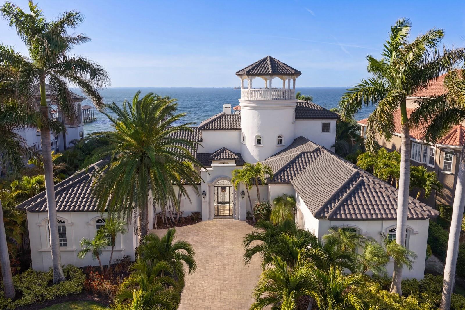 Exquisite Waterfront Estate in the private-gated estate enclave of Mustique Bay, offering refined indoor and outdoor living with multiple waterfront terraces, stunning bay views, and unforgettable western sunsets. Set on an Open Bay 0.7 acre mol waterfront lot with 100 ft of Tampa Bay frontage, enjoy endless days on the water from a dock complete with covered 13,000lb boat lift, double 6,000lb PWC lift as well as an additional uncovered PWC/Kayak lift. A gated entry and palm-lined drive create a gracious arrival to a residence that showcases timeless Mediterranean architecture, travertine flooring, and elegant architectural detailing throughout. A charming courtyard with a koi pond, framed by wrought iron gates, guides you to interiors defined by soaring ceilings and walls of glass that capture expansive water views. Mediterranean columns, a formal dining room, climate-controlled wine cellar, and a sweeping staircase enhance the home’s architectural presence, while a dual-sided fireplace anchors the main living area with warmth and sophistication. The expansive chef’s kitchen is thoughtfully appointed with a Viking professional gas range, stainless steel appliances, a generous island with prep sink and drawer fridge, concealed walk-in pantry, extended breakfast bar, and a wet bar with wine fridge for effortless entertaining. The kitchen flows seamlessly into the breakfast area and family room with retractable doors, all positioned to embrace the waterfront setting. A luxurious primary retreat welcomes you with Bay views and French door access to the pool, dual closets and an exceptional bath that includes a steam shower, dry sauna, and spa tub with courtyard views through a retractable, furniture quality roll-up door. Additional living spaces include an executive den/office with water views and fireplace, along with a first-floor ensuite guest bedroom, laundry room and pool bath. Upstairs, an additional ensuite guest bedroom offers French door access to a private multi-level terrace with water views, along with access to a third level outdoor tower entertaining terrace that features 360-degree views taking in St. Petersburg, South Tampa and Downtown Tampa. Spectacular Florida waterfront living awaits outdoors with a covered lanai, outdoor kitchen, and outdoor fireplace that overlooks a stunning resort-style infinity pool with multi-waterfalls and majestic Bay beyond. Additional appointments include a backup generator, water softener system, smart security and gate system, Anderson doors/windows, surround sound, fortified seawall, and 4 car garage spaces with spare utility space. Immerse yourself in magnificent waterfront living and embrace all that Apollo Beach has in this popular waterfront community. Featuring an abundance of recreation on and off the water, a central location provides easy access to beaches, shopping, dining, parks, Tampa, St. Petersburg and Sarasota.