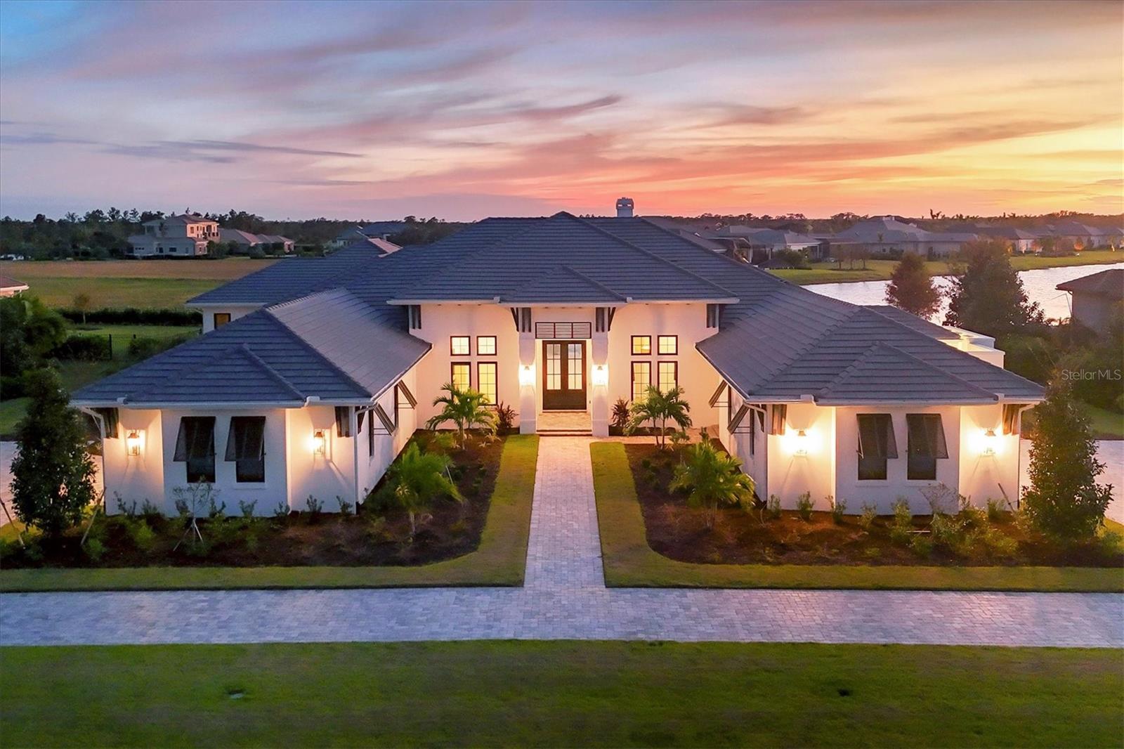 This newly constructed over 5,500-square-foot estate, built by John Cannon Homes and completed in October 2024, is set on an over-an-acre lot with stunning lake and sunset views in the prestigious gated community known as Concession. This home will be fully furnished, with furniture arriving soon to enhance its luxurious feel. The home features a grand entrance with an elongated driveway leading to 12-foot iron double doors that open into a vaulted great room with painted wood beams, a stone-framed gas fireplace and disappearing sliders that enhance the indoor-outdoor flow. The chef's kitchen boasts top-of-the-line appliances, including a Wolf six-burner range, built-in Wolf wall oven and warming drawer, Sub-Zero refrigerator and Fisher & Paykel dishwasher drawers. It includes double islands with quartz countertops, a hidden pantry, and a glass tile backsplash. A climate-controlled wine room with a backlit agate stone centerpiece adds elegance to the adjacent dining area. For entertainment, the club room, which opens onto the lanai, features a built-in beverage center with an ice maker and beverage drawers, leading to an HD golf simulator room. The outdoor retreat includes a screened lanai with beautiful gray porcelain tiles, an outdoor kitchen, gas fireplace with a TV wall, putting green, fire pit, and a heated saltwater pool and spa, all designed to maximize enjoyment of the panoramic lake views. The secluded owner’s suite offers additional lake views, oversized walk-in closets, and a spa-like bath with dual vanities, a glass dual-entry shower and an outdoor shower in a private courtyard. A casita off the lanai provides an ideal guest retreat with a morning bar, walk-in closet and full bath. Two additional guest suites with walk-in closets and en-suite baths are in a separate wing. The home also includes a double-door office with a built-in bookcase, a powder room, an oversized laundry room with built-in cabinetry, a built-in drop zone in the back hall, a storage room, a whole-house generator and a dual split 4.5-car garage with golf cart space. Wood floors throughout, California-style impact windows, custom lighting, and a Sonos, Control 4, and Lutron automated system, including shades, complete this exquisite home. With a total of 8,773 square feet, this residence embodies modern sophistication and refined living. In a serene community known for hosting the PGA World Golf Championships, it offers privacy while being close to Lakewood Ranch, UTC shopping, Sarasota’s beaches and cultural attractions, an ideal blend of luxury and convenience.