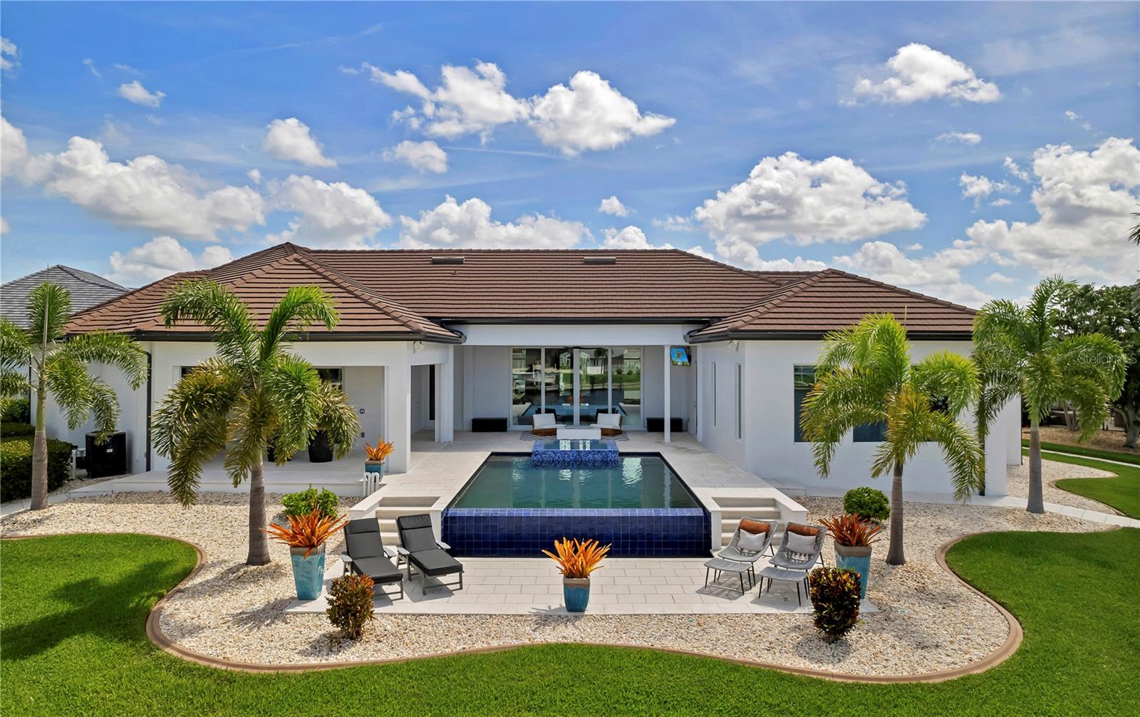 Positioned on a premier 255-foot waterfront key lot in the heart of Punta Gorda Isles, 2795 Bay Court is a rare expression of modern coastal luxury where architectural sophistication, yachting lifestyle, and intelligent design converge. Custom built by renowned builder PGI Homes, this exceptional residence was crafted for the buyer who values both striking design and uncompromising engineering.
From the moment you arrive, the home commands attention with coquina-wrapped columns, a dramatic illuminated fountain, and custom 10-foot iron entry doors that open into soaring interiors framed by expansive water views. Inside, every detail has been elevated: rich hardwood flooring, illuminated tray ceilings, floating cabinetry, marble feature walls, designer lighting and water views from every room.
The main living space was designed for effortless entertaining and everyday indulgence alike. A stunning chef’s kitchen anchors the home with Cambria quartz waterfall counters, premium appliances, custom cabinetry, oversized island seating, gold glass accents, and an adjoining catering kitchen for seamless hosting. The great room centers around a sculptural marble fireplace wall while opening completely to the resort-style lanai beyond.
Outside, the experience becomes unforgettable.
The infinity-edge saltwater pool and spa spill elegantly toward the water, surrounded by shell stone decking, expansive covered lounging areas, tongue-and-groove wood ceilings, oversized architectural fans, and a fully equipped outdoor kitchen featuring a Lynx rotisserie grill, burner, granite counters, and stainless ventilation hood. Every sunset here feels cinematic.

Designed with boaters in mind, the property offers 255 feet of substantial concrete dockage with integrated utilities, commercial-grade shore power, illuminated bollard lighting, fish cleaning station, and a 30,000-pound lift with quad motors and reinforced pilings, all positioned just moments from open water access to Charlotte Harbor.

The primary suite is a private waterfront retreat complete with custom boutique-style closets, chandelier accents, spa-inspired bath finishes, integrated audio, and panoramic water views. A separate VIP guest suite offers its own entrance, HVAC system, wet bar, wine fridge, icemaker, and blackout shades, creating a true private luxury experience for guests or extended stays.
Beyond its beauty, this home was engineered to perform at an elite level. Features include CAT-5 rated impact glass throughout, a 24KW whole-house Generac generator, three separate Carrier systems, buried propane tank, structured smart-home automation, enterprise-grade WiFi, integrated AI security systems, distributed Sonos and Klipsch audio, dedicated AV infrastructure, Starlink capability, and whole-property app-controlled functionality. 
2795 Bay Court is not simply another luxury waterfront home. It is a meticulously executed private coastal estate built for those who expect exceptional craftsmanship, seamless technology, and next level waterfront lifestyle.