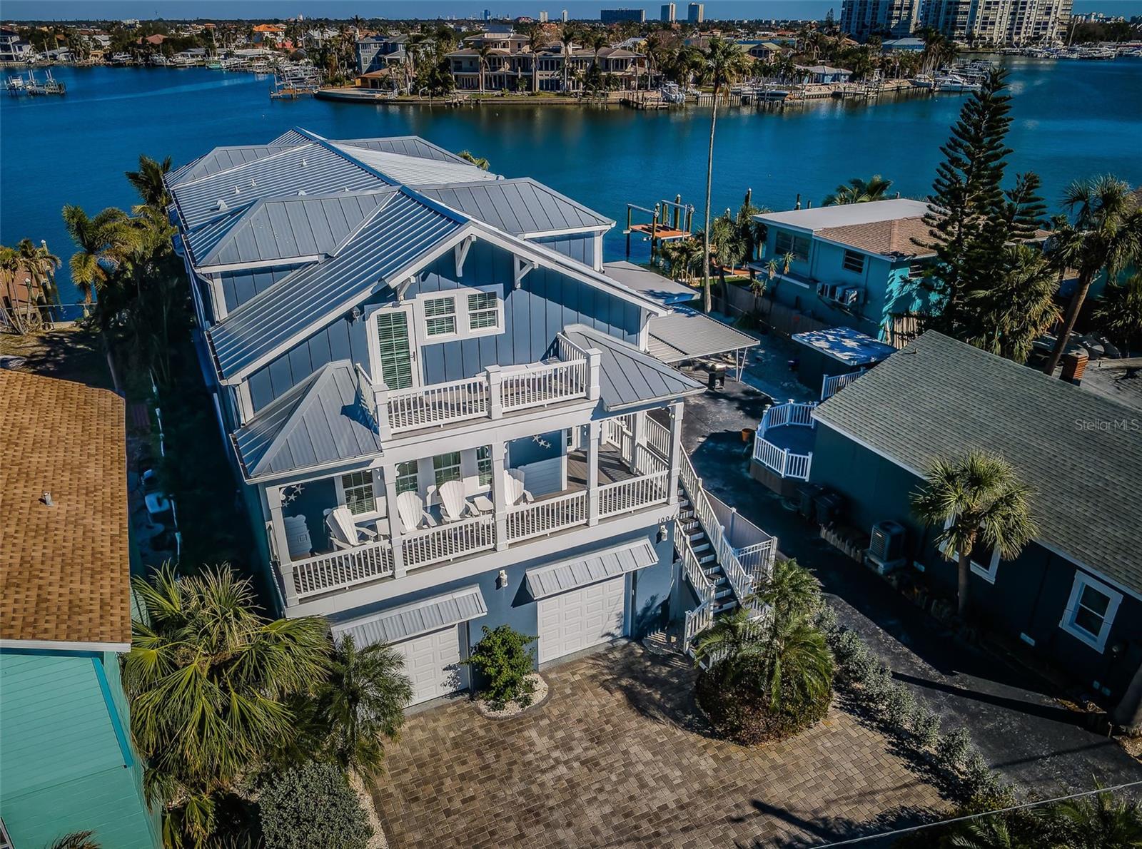 MOVE-IN READY!  LUXURIOUS, CONTEMPORARY WATERFRONT LIVING ACROSS FROM THE BEACH!  Beautifully landscaped with a large brick paver driveway, this extraordinary home enjoys many luxury upgrades/amenities. With focus on its “everyday is a vacation” lifestyle, this gorgeous waterfront residence offers 29-ft wide covered balconies front and back, as well front/back upper-level balconies. The entry foyer transitions to a superb open-concept gourmet chef’s kitchen boasting 2 multi-level breakfast/dining bars, granite surfaces, fine wood cabinetry, high-quality SS appliances, generous storage, matching built-in work center, and casual waterfront dining.  Lovely waterfront living room features an elegant built-in wetbar with Subzero wine chiller and stone tile entertainment wall with electric fireplace. Step out to the covered balcony and take in beautiful views of the pool/waterfront.  Home provides 2 owner’s suites (one on each level) with grand bedrooms, walk-in closet systems, and lavish baths with large dual vanities, and fabulous walk-in glass shower enclosures (one bath has a dedicated cosmetics center and the other, a posh soaking tub). Upper-level suite has extensive storage and a private balcony with Gulf/beach views.  The multi-purpose upper-level living/entertainment room, with a splendid luxury wetbar and full-height wine/beverage center, opens to a waterfront balcony with stunning panoramic vistas of the intracoastal waterway; room could easily become a bedroom suite.  The tall garage level is absolutely pristine, with fine epoxy flooring & storage capabilities. Garage passes to a unique 600sqft covered deck with travertine pavers that flow to/around the swimming pool. Covered deck features electronic storm shutters on 3 sides, turning the space into a private entertainment/dining room – on demand.  The large heated/cooled Pebbletec pool includes a sunshelf for in-pool lounging.  Beyond the pool deck is an impressive composite dock containing a 28,000lb boat lift with custom electric/hydraulic boat cover, 10,000lb dual PWC platform lift, 50 AMP service, step down area for kayaks/paddleboards, and mooring for a large cruiser. This amazing home including a 3-stop elevator and exquisite tilework/finishes. A 60-second walk to the beach, and 10-minute boat ride to the Gulf of Mexico. THE BEST OF BOATING AND THE BEACH and easy walking distance to dining/shopping/entertainment.  An outstanding waterfront value in a great location!